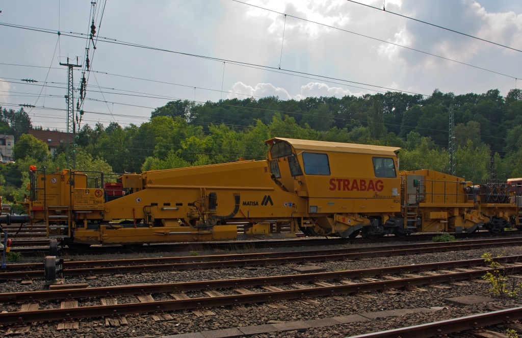 Die MATISA R24 Schotterplaniermaschine der STRABAG Rail GmbH (Schweres Nebenfahrzeug Nr. 99 80 9225 001-3 D-STRA) ist am 30.05.2012 in Betzdorf/Sieg abgestellt.

Die Maschine wurde 2009 von der MATISA Mat�riel Industriel S.A. in Crissier (Schweiz) unter der Fabrik-Nr. 47051 gebaut.

Die R 24 ist eine Hochleistungs-Schotterplaniermaschine auf Drehgestellen, speziell konzipiert f�r den Bau und den Unterhalt der Hochgeschwindigkeitsstrecken. Ihre beiden Kehrbesen garantieren eine ausgezeichnete Kehrleistung bei einer Geschwindigkeit von +/- 6 km/h.
Der erste Kehrbesen f�r die Strecke, best�ckt mit einem L�ngsf�rderband, sammelt den �bersch�ssigen Schotter auf den Schwellen und transportiert ihn mit dem F�rderband  in das15 m� gro�e Silo. So kann �bersch�ssiger Schotter zur�ck gewonnen und in Bereichen mit Schottermangel verteilt werden. Die 4 unabh�ngige Schotterhosen unter dem Silo verteilen den Schotter vor den Pfl�gen, welche diesen im gleichen Arbeitsgang auf dem Gleis verteilen. Der zweite Kehrbesen, f�r Weichen, ausger�stet mit einem Querf�rderband, verteilt den Schotter zur linken und rechten Seite. Mit seiner sehr ger�umigen Kabine, die auch an spezifische Kundenw�nsche angepasst werden kann, bietet die R 24 einen gro�en Komfort.

Die Maschinen sind mit einem hydrostatischen Fahrantrieb ausgestattet, der einfach und bequem zu bedienen ist. Die Fahrgeschwindigkeit kann ohne Rucken durch Schaltvorg�nge gesteuert werden. Das ruckfreie Fahren erh�ht den Komfort und ist ein Gewinn f�r Mensch und Maschine, und das jeden Tag. Ein weiterer Vorteil des hydrostatischen Fahrantriebs ist, dass ein Schlupf der R�der beim Anfahren verhindert wird.

TECHNISCHE DATEN: 
Spurweite: 1.435 mm  (Normalspur)
Achsanzahl: 5 (2 Drehgestellen, eine einzelne Achse)
Achsformel: Bo´ + A1´ + 1
L�nge �ber Puffer: 26.500 mm
Drehzapfen- bzw. Achsabstand: 12.500 mm / 8.000 mm
Achsabstand in den Drehgestellen: 1.800 mm
Treib- und Laufraddurchmesser: 920 mm (neu)
H�he: 4.263 mm
Breite: 3.050 mm
Eigengewicht: 68.420 kg
Anh�ngelast: - t
Zur Mitfahrt zugel. Personen: 5
H�chstgeschwindigkeit (geschleppt): 100 km/h 
H�chstgeschwindigkeit Eigenfahrt: 25 km/h (nur als Rangierfahrt)
Max. Geschwindigkeit beim Planieren: 15 km/h
Max. Geschwindigkeit beim Kehren: 6 km/h     
Zugelassen ab Streckenklasse: C2 
Kleinster befahrbarer Kurvenradius:  R 250 m  (Fahrzeug allein 90 m)
Min. Radius bei Arbeit: R 190 m
Bremse: 2 x KE-GP (K), Max. 57 t
Dieselmotor:  DEUTZ wassergek�hlter V8-Zylinder-Viertakt- Dieselmotor mit Turboaufladung, Ladeluftk�hlung, Vierventiltechnik und wassergek�hlte Abgasrohre vom Typ DEUTZ BF 8 M 2015 CP 
Motorleistung: 440 kW (598 PS) bei 2.100 U/min
Motorhubraum: 15,9 Liter (Bohrung 132 mm / Hub 145 mm)
Motorgewicht: 1.060 kg
Gr��e Schottersilo:15 m�  (Standard 10 m�)
Tankvolumen: 3.000 Liter  (Standard 2 m�)

Bemerkung: Laut Prospekt von Matisa kann die Maschine in Eigenfahrt auch 100 km/h schnell fahren (dann hat sie nur 2 Achsen angetrieben), aber laut Anschriftentafel ist eine Eigenfahrt nur als Rangierfahrt mit 25 km/h zugelassen.
