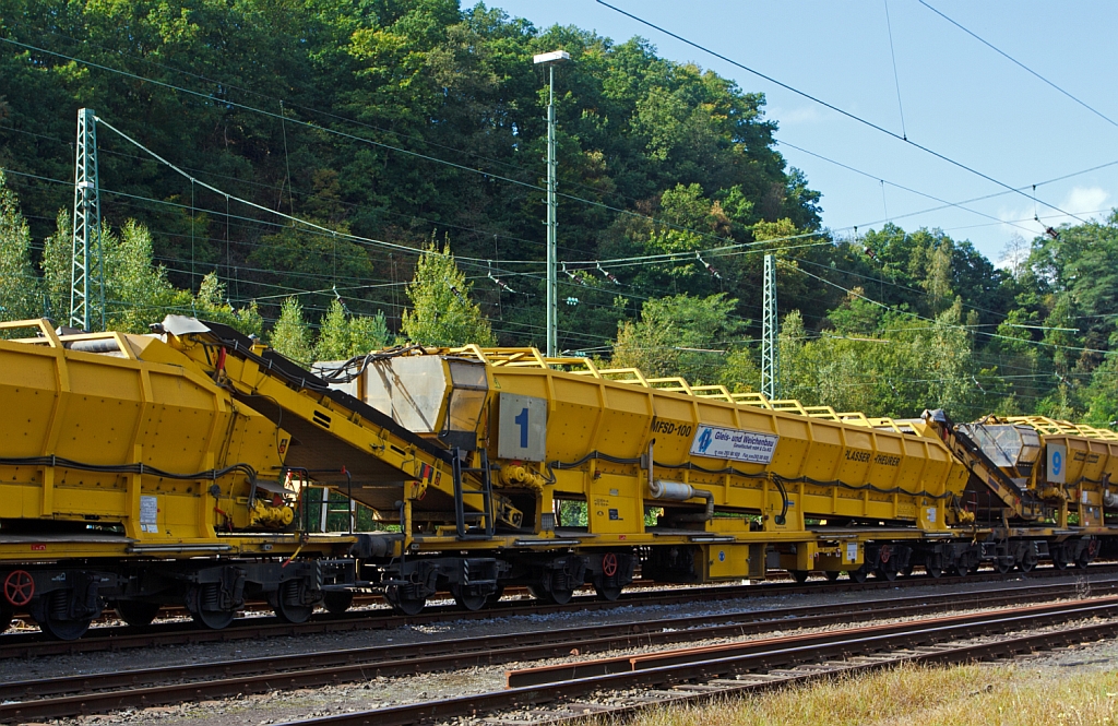 Plasser & Theurer Materialf�rder- und Siloeinheit MFSD 100 der MGW Gleis- und Weichenbau-GmbH (Berlin) Nr. 1 (Schweres Nebenfahrzeug Nr. 97 19 29 55057-4) EBA-Nr. 00 D05 A009,  abgestellt in Betzdorf/Sieg am 22.09.2012.
Die MFS 100 und dienen zum Transport von Schotter, Abraum und Pufferspeicher bei der Bettungsreinigung bzw.Planumsverbesserung. Hauptvorteil ist der kontinuierliche F�rder-, Speicher- und Entladevorgang. Eine Zusammenstellung von beliebig vielen MFS-Wagen zu einem Zug mit jeweils gew�nschter Speicherkapazit�tist m�glich. Der  F�llvorganges beginnt beim  vordersten Wagen (in Arbeitsrichtung), die folgenden Wagen dienen als F�rderstra�e.
Die MFSD 100 sind nur als Durchlader einsetzbar, das �bergabeband nicht schwenkbar,  somit keine Entladung zum Nachbargleis m�glich.
Diese Einheit wurde 2003 unter der Fabriknummer 4064 gebaut.
Technische Daten: L�nge �ber Puffer 22.900 mm > L�nge inkl. F�rderband 26.550 mm > Achszahl 8 (2 Drehgestelle mit je 4 Achsen) > max. Achslast (beladen) 18t > Eigenmasse 54 t > max. zul�ssige Zuladung 90 t > Motorleistung 160 kW f�r Antrieb der F�rderb�nder > max. Geschwindigkeit im Zugverband 100 km/h > max. Fassungsverm�gen 68 m�.