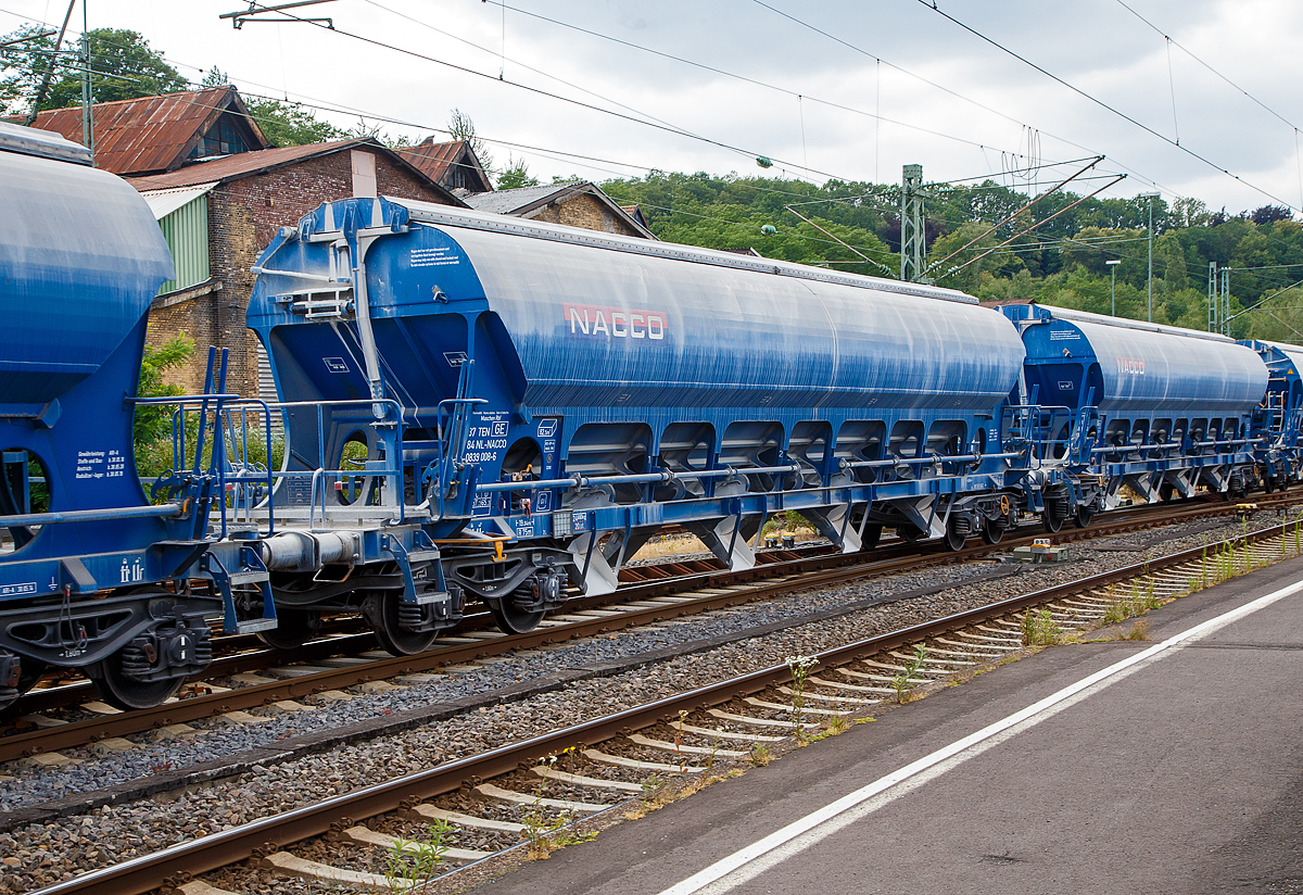 4-achsiger Trichtermittenentladewagen 82,5 m� der Gattung Tadns (Drehgestell-Sch�ttgutwagen mit Schwenkdach) beladen mit Kalk, 37 84 0839 008-6 NL- NACCO, der NACCO GmbH, am 07.07.2019 im Zugverbund bei einer Zugdurchfahrt in Betzdorf (Sieg). Seit August 2018 geh�ren diese Wagen der WASCOSA AG und wurden sp�ter umgezeichnet. 

Der mit einer hohen bilateral kontrollierten Schwerkraftentladung und einem zu �ffnenden Dach ausgestattete Wagen ist f�r den Transport von Kalksteinen und anderen Sch�ttg�tern, die vor Witterungseinfl�ssen gesch�tzt werden m�ssen, konzipiert worden. Das Sch�ttgut wird mit Hilfe der Schwerkraft �ber die Dach�ffnung eingef�llt. Das kontrollierte Entladen wird manuell durchgef�hrt. Die Entleereinrichtung besteht aus 4 Auslauftrichtern die mit je 2 Klappen verschlossen sind und manuell per Hebel, einzeln von den beiden Plattformen an den Wagenenden aus bet�tigt werden. Die Komplette Entladung des Wagens ist durch �ffnung auf nur einer Seite m�glich. Die Entladung des Wagens erfolgt auf F�rderb�ndern oder in unterirdische Bunker.

TECHNISCHE DATEN:
Hersteller: Astra Rail Industries (Rum�nien) geh�rt zu Greenbrier Europe
Spurweite: 1.435 mm
Ladeprofil: G1-TSI
L�nge �ber Puffer : 19.040 mm
Drehzapfenabstand: 14.000 mm
Achsabstand im Drehgestell: 1.800 mm
Eigengewicht: 24.680 kg
H�chstgeschwindigkeit: 100 km/h (beladen) / 120 km/h (leer)
Maximales Ladegewicht: 65,3 t (ab Streckenklasse D)
Kleinster bef. Gleisbogenradius: 75 m
Rauminhalt: 82,5 m�
Lade�ffnung: 15.080 x 1.200 mm
Dach: Spritzwasserfestes Hub-/Schwenkdach mit Handbet�tigung
Drehgestell-Typ: Y25Lsd-KP1
Laufraddurchmesser: 920 mm (neu)
Bremse: KE-GP-A (K) max. 58 t
Bremssohle: C 810
Intern. Verwendungsf�higkeit: TEN GE 
Heimatbahnhof: Maschen Rbf

Ein paar Worte zu ehemals NACCO:
Die VTG AG in Hamburg hatte die CIT Rail Holdings (Europe) SAS, der Eigent�merin der NACCO-Gruppe im M�rz 2018 �bernommen. Die zust�ndigen Kartellbeh�rden hatten der VTG AG den Erwerb unter der Auflage genehmigt, dass rund 30 Prozent des G�terwagenbestands an einen Dritten zu ver�u�ern sind.

Die Schweizer Wagenvermieterin Wascosa AG hat rund 4.400 G�terwagen von NACCO/CIT und somit und 30 Prozent der G�terwagenflotte der NACCO-Gruppe �bernommen. Nebst dem operativen Gesch�ft und den Wagenmietvertr�gen hat Wascosa auch die Mitarbeiter der NACCO GmbH in Hamburg �bernommen. Mit der �bernahme der rund 4.400 G�terwagen ist die Flotte von Wascosa auf �ber 14.000 G�terwagen angewachsen.Damit r�ckt das Unternehmen hinter VTG, Ermewa und GATX an die vierte Stelle der europ�ischen Wagenvermieter.
