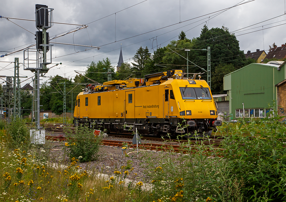 Das Oberleitungsinstandhaltungsfahrzeug 711 201 (99 80 9136 001-1 D-DB) der DB Netz AG, ein Robel 57.44, f�hrt am 15.07.2021 durch Betzdorf (Sieg) in Richtung K�ln.

Der IFO 57.44 wurde 2009 von der ROBEL Bahnbaumaschinen GmbH in Freilassing unter der Fabriknummer 57.44-001 gebaut und an die DB Netz AG geliefert.

Zur neusten Generation an Fahrzeugen f�r die Durchf�hrung von Instandhaltungs- und Entst�rungsarbeiten an Oberleitungsanlagen geh�rt die von der Deutsche Bahn AG bezeichnete Baureihe 711.2, welche von der Firma ROBEL Bahnbaumaschinen GmbH in Freilassing seit 2009 unter der Bezeichnung IFO 57.44 hergestellt wird.

Im Auftrag der DB hatte die Firma Robel mit dem IFO 57.44 ein vierachsiges Fahrzeug f�r Reparaturen und Wartung an Oberleitungsanlagen entwickelt, dass auf allen Strecken der DB einsetzbar ist. 

Der Wagenkasten ist zweckm��ig gestaltet und mit Stahlblech verkleidet. An den Fronten finden sich unter der Verkleidung der Fahrzeugk�pfe, die an moderne Elektrolokomotiven angelehnt sind, stabile Schwei�konstruktionen zur Aufnahme der bei einem Unfall freiwerdenden Kr�fte.

Der Antrieb erfolgt durch zwei Dieselmotoren der Bauart TCD 2015 V08 von Deutz mit jeweils 480 kW, die jeweils mittels eines hydraulischen Getriebes (Voith Turbogetriebe T 212 bre),    auf beide Achsen (mit je einem Voith Radsatzgetriebe SK-525) eines Drehgestells wirken. Lassen es die Streckenverh�ltnisse zu oder kommt es zu St�rungen, kann auch mit nur einer Antriebsanlage gefahren werden. F�r die Arbeitsfahrt (bei den Montage- und Wartungsarbeiten) ist an einem Drehgestell ein hydrostatischer Antrieb installiert, der durch einen der beiden Haupt-Dieselmotoren angetrieben wird. Dieser erlaubt eine Fahrt im Geschwindigkeitsbereich von 0 bis 10 km/h. Die H�chstgeschwindigkeit betr�gt 140 km/h (Technisch m�glich 155 km/h), was vor allem f�r die schnelle Beseitigung von St�rungen n�tig ist. Bei einer Fahrt mit 100  km/h kann das Fahrzeug eine Anh�ngelast von 150 t bef�rdern und ist hierzu mit einer Schraubenkupplung ausger�stet.

Das Fahrzeug besitzt zwei Endf�hrerst�nde mit jeweils zwei Pl�tzen. �ber ein Monitorsystem k�nnen die Fahrzeugl�ngsseiten beobachtet werden. Eine weitere Kamera ist auf die Oberleitung und den Mess-Stromabnehmer gerichtet, wobei die Bilder zur sp�teren Dokumentation aufgezeichnet werden k�nnen. An die F�hrerst�nde schlie�en sich Sozial- und Arbeitsr�ume an. So ist beispielsweise f�r l�ngere Eins�tze eine vollwertige K�chenzeile mit K�hlschrank, Mikrowelle und Kaffeemaschine eingebaut worden. Ebenfalls vorhanden ist eine Nasszelle, deren Abw�sser �ber einen Bioreaktor aufbereitet und erst dann gereinigt in das Gleis abgegeben werden. Mittelpunkt des Fahrzeugs ist der Arbeits- und Werkstattraum, der von au�en �ber die beidseitigen 1.510 mm breiten T�ren erreichbar ist. Auf beiden Seiten befinden sich ausschwenkbare Hebevorrichtungen f�r Lasten bis zu 250 kg. 

Auf dem Dach befinden sich zwei Hubarbeitsb�hnen, je eine vom Typ PA 95 und eine vom Typ PA 360 der Firma Palfinger. Die PA 95 ist vorrangig f�r Arbeiten am Fahrdraht bis zu einer H�he von 9 m �ber Schienenoberkante gedacht, w�hrend mit der PA 360 bis zu einer Arbeitsh�he von 21 m auch das Kettenwerk und Mastspitzen erreicht werden k�nnen. Auch ein Absenken der B�hne neben dem Fahrzeug ist m�glich, um beispielsweise Ger�te und/oder Material aus dem Werkstattwagen direkt in die B�hne umzuladen.

Von diesem modernen Fahrzeug hatte die Deutsche Bahn AG urspr�nglich acht Fahrzeuge dieser Bauart bestellt, die bis zum Sommer 2011 ausgeliefert wurden. Sie kommen im gesamten deutschen Streckennetz zum Einsatz und ersetzen die �ber 30 Jahre alten Turmtriebwagen der DB-Baureihe 704. Ab Februar 2014 wurden nach einem Folgeauftrag vier weitere Fahrzeuge ausgeliefert.

Das Fahrzeug ist in dieser Ausf�hrung speziell f�r die Belange der Deutschen Bahn AG konstruiert worden, kann aber bei Bedarf auch f�r andere interessierte Bahnunternehmen auf deren spezifische Anforderungen angepasst werden.

TECHNISCHE DATEN:
Hersteller: ROBEL Bahnbaumaschinen GmbH, Freilassing
Spurweite: 1.435 mm (Normalspur)
Achsformel:  B'B'
L�nge �ber Puffer:  24.500 mm
Drehzapfenabstand: 17.000 mm
Achsabstand im Drehgestell: 2.500 mm
Eigengewicht:  77 t
H�chstgeschwindigkeit:  140 km/h (Technisch m�glich 155 km/h) / geschleppt 120 km/h
Tankinhalt:  2�750 l
Leistung: 2 x 480 kW (2 x 652 PS)
Kraft�bertragung:  hydrodynamisch (Streckenfahrt) hydrostatisch (Arbeitsfahrt)
Zur Mitfahrt zugel. Personen: 9
Anh�ngelast: 150 t
Zuladung  5 t
Bremse: KB C-KE-PR-H mZ (D)

Motordaten:
2 St�ck Deutz - wassergek�hlter-V8-Dieselmotor mit Turboaufladung, Ladeluftk�hlung und Vierventiltechnik. Motor in V-Ausf�hrung im Winkel von 90�, er hat ein elektronisches, �ber Magnet-Ventile gesteuertes Einspritzsystem.
Motortyp: TCD 2015 V08
Zylinderzahl: 8
Bohrung/Hub: 132 / 145 mm
Hubvolumen: 15,9 l
Verdichtungsverh�ltnis: 17,5:1
Nenndrehzahl: 1800 min-1 
Leistung: 480 kW (652 PS)
Max. Drehmoment: 2.890 Nm
Niedrigste Leerlaufdrehzahl:  600 min-1
Motorgewicht: 1.245 kg

Getriebe f�r Streckenfahrt (2 St�ck):
Voith Turbogetriebe T 212 bre 

Das Turbogetriebe ist ein 3-Gang-Getriebe mit einem Drehmomentwandler, zwei Str�mungskupplungen, einer integrierten hydrodynamischen Bremse und mechanischem Wendeteil. Zus�tzlich ist eine Voith-Federkupplung an das Schwungrad des Dieselmotors angeflanscht.

Bei Traktion erfolgen die Gangwechsel automatisch ohne Zugkraftunterbrechung weich, sto�- und verschlei�frei durch    F�llen und Entleeren der Kreisl�ufe. Die dynamische Bremse erm�glicht verschlei�freies Bremsen, kurzzeitig bis 450 kW Bremsleistung.

Die Kraft�bertragung vom Turbogetriebe erfolgt �ber Gelenkwellen auf Voith Radsatzgetriebe SK-525 (1 St�ck/Achse = 4 St�ck) und somit auf die Achse.
