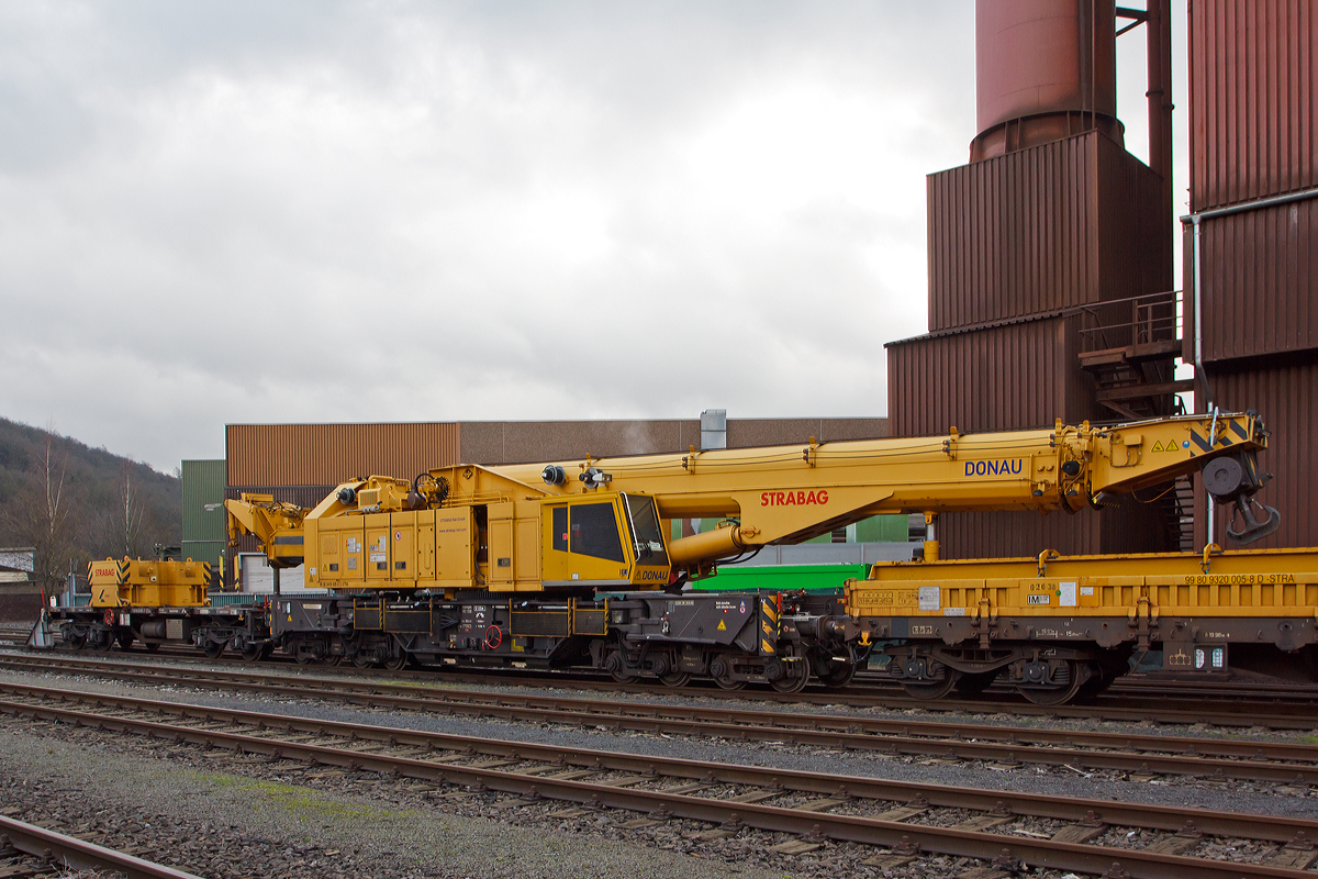 Der 150 t Kirow Gleis- und Weichenbaukran KRC 1200+ (ein Kirow MULTI TASKER KRC 1200+) 99 80 9419 005-0 D-STRA  „DONAU“  (ex 97 82 55 508 17-5) der STRABAG RAIL GmbH ist am 25.12.2014 am KSW Bahnhof Siegen-Eintracht (Betriebsbereich Eisern-Siegener Eisenbahn), in Transportstellung abgestellt. 

Vor dem Kran ist der Schutzwagen 99 80 9320 005-8 D-STRA eingestellt, auf diesem befinden sich auch die zugeh. Traversen und Anschlagmittel. Hinter dem Kran ist der Gegenlastwagen 99 80 9320 001-7 D-STRA eingestellt, auf diesem befinden sich die zugeh. Gegengewichte des Kranes. Auf beide Wagen ist zur Achslastreduzierung der Kran mittel Hydraulikzylinder abgest�tzt, auf den Schutzwagen der Kranausleger und auf den Gegenlastwagen der Gegengewichtausleger.

TECHNISCHE DATEN von dem Kran:
Spurweite: 1.435 mm
Eigengewicht  (in Transportstellung) : 111,0 t 
L�nge �ber Puffer:  15.000 mm  (+13.000 mm Gegenlastwagen)
Motorleistung:  254 kW bei 2.200 U/min
max. Geschwindigkeit im Zugverband: 100 km/h
max. Geschwindigkeit im Eigenantrieb: 20 km/h
Achsanzahl:  8 (in 4 Drehgestelle bzw. 2 Doppeldrehgestelle)
Drehzapfenabstand: 10.000 mm
Drehzapfenabstand im Drehgestell 1 und 2: 2.300 mm
Achsabstand in den Einzeldrehgestellen: 1.100mm
Ergebene Achsabst�nde in m: 1,1 / 1,2 / 1,1/ 6,6 / 1,1 / 1,2 / 1,1
Achsfolge: 1'A'1A'A1'A1'
Radsatzlast Transport Kran: max. 13,8 t
Radsatzlast Gegengewichtswagen:  max. 20,0 t
Meterlast (Streckenlast) in Transportstellung Kran max.: 7,4 t/m
H�he in Transportstellung:  4.300 mm
Breite in Transportstellung:  3.100 mm
max. Ausladung vor Puffer:  21.000 mm
max. Traglast bei max. Ausladung:  40 t
Gr��te m�gliche Traglast: 150 t
max. Hakenh�he:  24.000 mm
hintere Ausladung (Gegenwicht):  7,9 m–13,5 m
Kleinster befahrbarer Radius: 80 m (125 m im Schleppbetrieb)

Besondere Ausstattung:
�berh�henausgleich 180 mm
Schwenkradius � 360�
Abst�tzung teleskopierbar bis 8 m Abst�tzbasis
profilfreies Arbeiten bis � 30�

Der Kran wurde 2009 von Kirow in Leipzig unter der Fabriknummer 152500 gebaut. Er wird als Schweres Nebenfahrzeug Nr.: 99 80 9419 005-0 (ehemals 97 82 55 508 17-5) gef�hrt und hat die EBA-Nr. EBA 09C02A001.

Der Kran geh�rt zu einer der gr��ten Gleisbaukranklassen, hat aber in der Transportstellung durch die Abst�tzungen auf den Kranauslegerschutzwagen und den Gegenlastwagen geringere Streckenlast (Meterlast) von max. 7,4 t/m, als seine kleineren Br�der.
Das Gegengewicht ist ausfahrbar und separat bis � 30�  schwenkbar, sodass ein Einschwenken in den Bereich des Nachbargleises vermieden und ein profilfreies Arbeiten erm�glicht wird.
