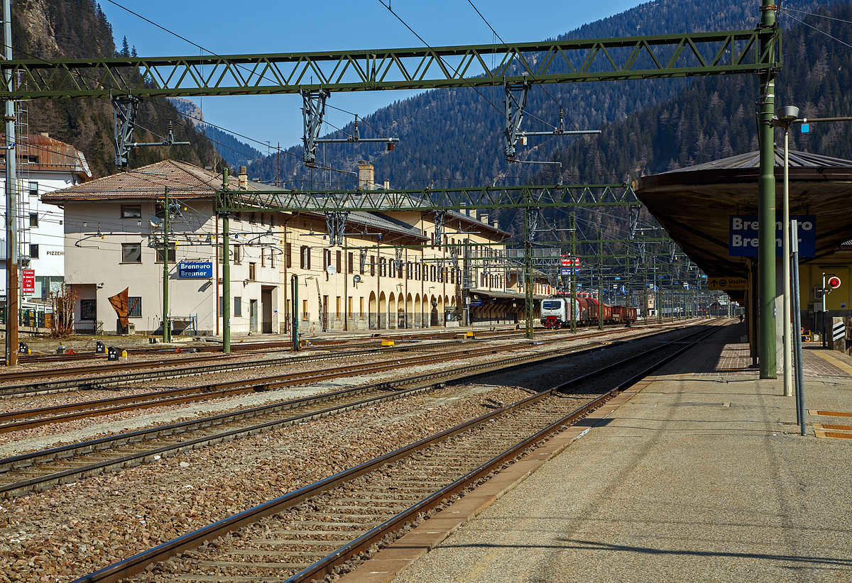 Der Bahnhof Brenner (Stazione di Brennero) am 26.03.2022, der Blick vom Bahnsteig 6 in n�rdlicher Richtung aufs Empfangsgeb�ude. Recht weit hinten liegt der �sterreichischen Teil.

Der Bahnhof Brenner (italienisch Stazione di Brennero) befindet sich an der Brennerbahn. Er ist der Grenzbahnhof zwischen Nord- und S�dtirol und so zwischen �sterreich und Italien. Der Bahnhof liegt auf der Passh�he des Brenners (1.370 m). Dieser enge, h�chstgelegene Abschnitt des Wipptals bietet zwischen steilen Bergh�ngen nur wenig Platz f�r das kleine Passdorf und wird zu gro�en Teilen von Verkehrsinfrastrukturen wie dem Bahnhof, der A22/A 13 und der SS 12/B 182 beansprucht. Der Bahnhof befindet sich fast zur G�nze auf dem Gebiet der S�dtiroler Gemeinde Brenner bzw. auf italienischem Staatsgebiet, das hier auch auf Fl�chen n�rdlich der Wasserscheide �bergreift. Lediglich kleinere Teile im n�rdlichen Bereich des Bahnhofs geh�ren zur Tiroler Gemeinde Gries bzw. zum �sterreichischen Staatsgebiet.

Der von Wilhelm von Flattich entworfene Bahnhof Brenner wurde 1867 zusammen mit dem gesamten Abschnitt der Brennerbahn zwischen Innsbruck und Bozen in Betrieb genommen, damals geh�rte ja noch alles zur Doppelmonarchie �sterreich-Ungarn. An den planenden Ingenieur des Projekts, Carl von Etzel, erinnert eine Bronzeb�ste am Bahnhofsgel�nde. Die urspr�nglich relativ unbedeutende Station erfuhr 1888 aufgrund der hohen Fahrgastzahlen der neuen Strecke eine erste Erweiterung.

Die Annexion S�dtirols durch Italien infolge des Ersten Weltkriegs ver�nderte die Situation grundlegend, da nun die neue Staatsgrenze �ber den Brenner verlief. Die Teilstrecken Innsbruck–Brenner und Verona–Brenner wurden von nun an von zwei verschiedenen Verwaltungen betreut, die sich zudem noch in feindseliger Haltung gegen�berstanden. 1930 wurde ein kompletter Neubau des Empfangsgeb�udes eingeweiht.