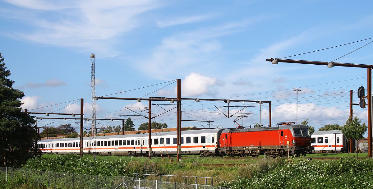 Der IC 1197 Kopenhagen Hbf - Hamburg Hbf mit DSB EB 3211 an der Spitze hat am 15.08.2023 in Pattburg/Padborg bereits über eine Stunde Verspätung und blockiert somit das Gleis 2 für den Gegenzug IC 1192, der bereits am Einfahrtsignal wartet, da auf Gleis 1 noch die Gumminase nach Aarhus steht.
Um 17.10 Uhr fährt IC 1197 vorsichtig Richtung Hamburg Hbf aus, kommt aber am Ausfahrtsignal wieder zum Stehen. Zwischenzeitlich hatte die Gumminase das Gleis 1 geräumt und man sieht im Hintergrund den letzten Wagen des IC 1192. Zwei ellokbespannte IC in unterschiedlichen Richtungen hatte ich bislang noch nicht gleichzeitig Pattburg gesehen