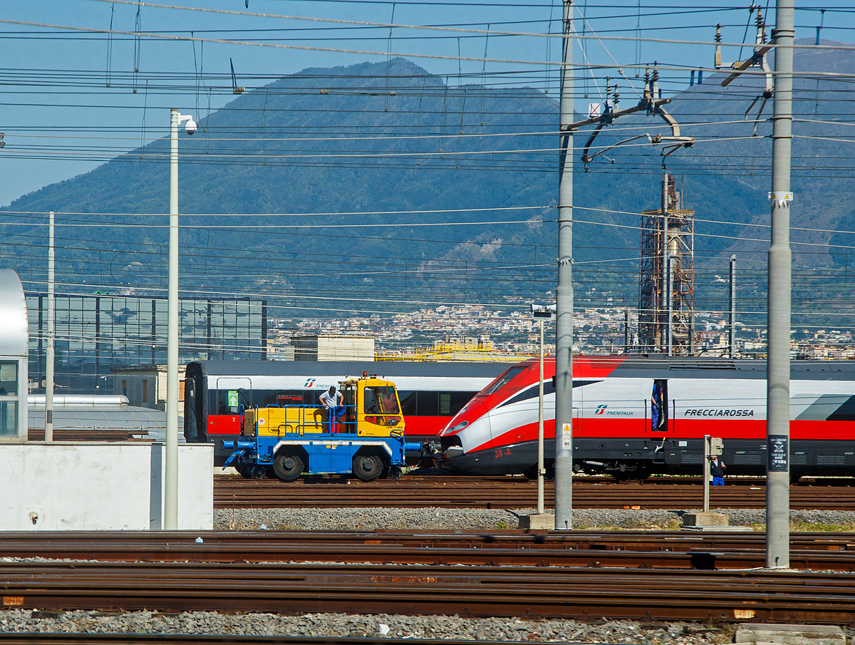 Der Trenitalia am 14.07.2022 aus dem Zug ins Depot in Neapel (Napoli) geschaut: Hier vor dem Trenitalia ETR 500 39 der Zephir Zweiwege-Rangierer (Elektro/Akku Rangierfahrzeug) vom Typ LOK 7.90E. 

Der italienische Hersteller ZEPHIR SpA in Modena ist seit über 50 Jahren der Marktführer in Europa für innovative Zweiwege Rangier Locotraktoren und industrielle Rangiertraktoren. Durch die Gummibereifung (Traktion am Gleis) hat ein solches Fahrzeug einen mehr als 2 x höheren Reibungskoeffizient als bei einer Lok.

TENISCHE DATEN von dem Rangierer:
Spurweite: 1.435 mm (normalspur)
Länge über Kupplung: 4.800 mm
Breite ca.: 2.500 mm
Höhe ca.: 3.400 mm  
Gewicht: 16.000 kg
Motorleistung: 30 kW 
Zugkraft: 70 kN 
Max. Anhängelast: 1.400 t 
Höchstgeschwindigkeit: 7 km/h