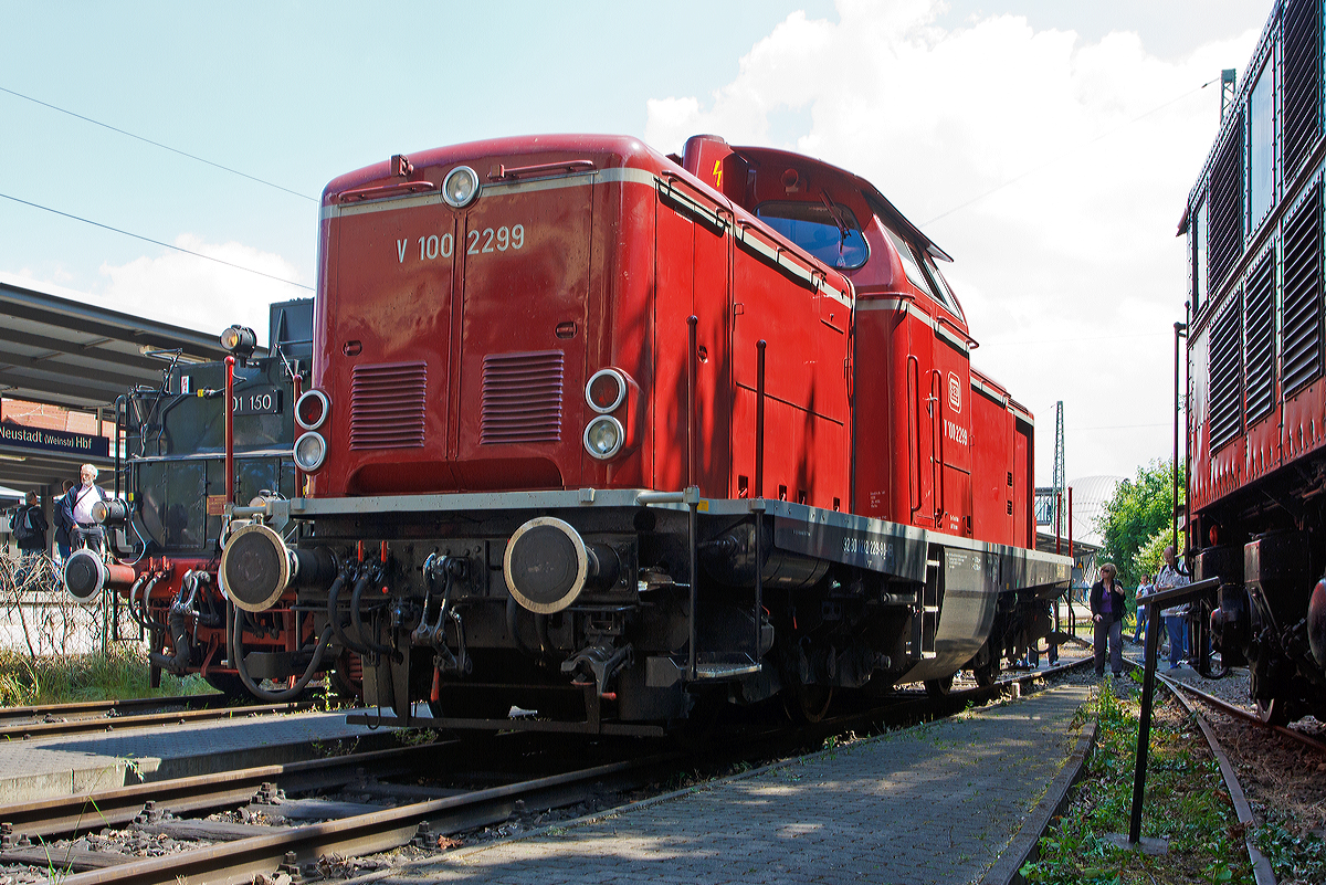 
Die Die V100 2299 (92 80 1212 229-9 D-VEB), ex DB 212 299-2, der VEB (Vulkan-Eifel-Bahn) ist am 31.05.2014 im DGEG Eisenbahnmuseum Neustadt/Weinstraße (Pfalzbahn - Museum), beim Dampfspektakel 2014, abgestellt. 
Die V 100.20 wurde 1965 bei MaK unter der Fabriknummer 1000346 als V 100 2299 für die DB gebaut. 1968 wurde sie 212 299-2 umbezeichnet, die Ausmusterung bei der DB erfolgte 2002., über ALS, Stendal ging sie dann an die VEB die sie wieder in V 100 2299 um bezeichnete, wobei sie die NVR-Nummer 92 80 1212 299-2 D-VEB trägt. Die Leistung der Lok beträgt 993 kW / 1.350 PS, die Höchstgeschwindigkeit 100 km/h.

Nachdem man eine der Vorserienloks der V100.10 probeweise mit einem 1350 PS starken Motor versehen hatte und diese sich im Betrieb bewährte, wurde zunächst eine Serie von 20 Lokomotiven bestellt, die bis auf den stärkeren Motor der Serie der V100.10 entsprachen.
Bei der ab 1963 gelieferten Serien wurde dann der Rahmen um 200 mm verlängert und der Lüfter wurde nun nach vorne von senkrecht stehenden Lamellen bedeckt.

Gebaut wurden die Loks zum überwiegenden Teil bei MaK, aber auch Deutz (70), Henschel (58) und Jung (37) kamen zum Zuge. Eng verwandt mit der V100.20 sind auch die Steilstreckenloks der späteren Baureihe 213.

Als Motor verwendete man ein 12-Zylinder-V-Dieselmotor vom Typ Daimler-Benz MB 835 Ab (MB 12 V 652 TA/TZ) mit einem Gesamthubraum  von 78,25 Liter der durch einen BBC VTR 250-Abgasturbolader aufgeladen wird, und so eine Leistung von 1350 PS (994 kW) abgibt. Der Dieselmotor incl. Regler wiegt ca. 4.500 kg.

Durch die hohe Motorleistung musste Voith ein neues Strömungsgetriebe für die V 100 entwickeln. Das Ergebnis war das L 216 rs, das in dreistufiger Bauart mit zwei Wandlern und einer hydraulischen Kupplung ausgeführt ist. Das L 216 rs-Getriebe war auf eine Getriebeeingangsleistung von 953 kW (1.300 PS) ausgelegt, was wegen der Verluste vor dem Getriebeeingang auch für einen 990 kW (1.350 PS)-Motor ausreichte. Durch Wirkungsgradverluste im Getriebe liegen die Getriebeausgangsleistungen bei der V 100.20 bei 790 kW (1.075 PS).

Das L 216 rs besteht aus einem Anfahrwandler als ersten, einem Marschwandler als zweiten und einer hydraulischen Kupplung als dritten Gang. Die hydraulische Kupplung setzte man wegen ihres um ca. 6 % besseren Wirkungsgrades ein. Sie dient nur für Beharrungsfahrten bei hohen Geschwindigkeiten; in der Beschleunigungsphase sind die beiden Wandler gefordert.
Die Umschaltung zwischen Langsam- und Schnellgang bzw. Rangier- und Streckengang (Stufenschaltung) erfolgt über zwei Zahnradpaare zwischen der Vorgelegewelle und der darauf folgenden Abtriebswelle. Je ein Zahnradpaar bilden die Übersetzung für Langsam- und Schnellgang. Die Umschaltung erfolgt über einen Handschalthebel und ein mechanisches Gestänge im Stand. Das Strömungsgetriebe wiegt incl. Ölfüllung ca. 4.665 kg.

Für die Stromversorgung im Stand hat die Lok einen Hilfsdieselmotor, mit einer sensationell niedrigen Leistung. Der Hilfsdieselmotor vom Typ AKD 412 Z der Motorenwerke Mannheim (MWM), sitzt im vorderen Vorbau zwischen Hauptdieselmotor und Kühler. Mit einem Hubraum von 2,08 l und einem Gewicht von ca. 580 kg leistet der luftgekühlte Zweizylinder-Viertakt-Reihenmotor satte 16,2 kW und hat eine Nenndrehzahl von 1.800 U/min. Er treibt einen Gleichstromgenerator GZ 164-24 der Fa. Still an, der bei einer Betriebsspannung von 120 V volle 11 kW leistet.

Technische Daten:
Spurweite: 1435 mm
Achsfolge:  B´B´
Länge über Puffer: 12.300 mm
Drehzapfenabstand: 6.000 mm
Drehgestellachsstand: 2.200 mm
größte Breite: 3.115 mm
größte Höhe über Schienenoberkante: 4.275 mm
Raddurchmesser: 950 mm (neu)
kleinster befahrbarer Gleisbogen: 100 m
Dienstgewicht: 63 t
Motor: Daimler-Benz MB 835 Ab, ein 12-Zylinder-V-Dieselmotor mit Abgasturbolader
Motorleistung: 1.350 PS (994 kW) mit max. 1.500 1/min
Getriebe: Voith L216rs
Höchstgeschwindigkeit: 100 km/h
Kraftstoffvorrat: 2.270 l
