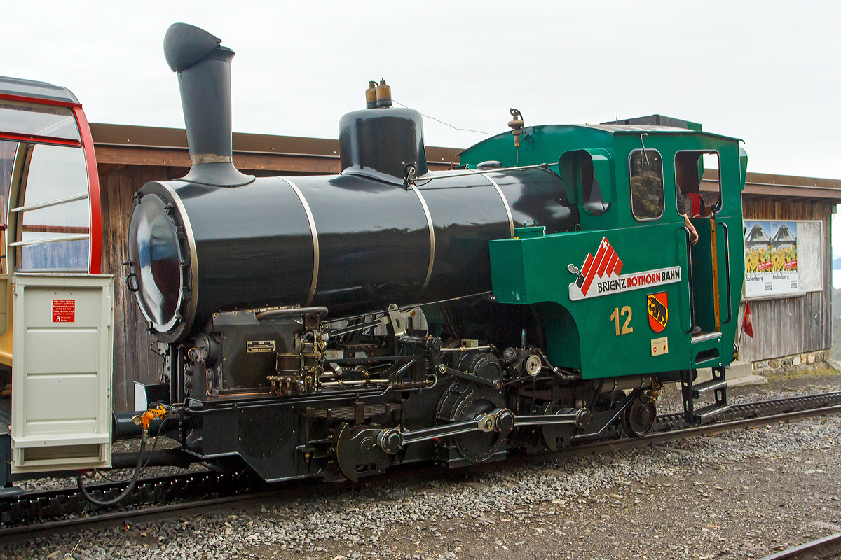 
Die Heizöl befeuerte BRB 12 (Kanton Bern) steht am 29.09.2012 mit ihrem Zug an der Bergstation Rothorn Kulm (2.244m ü. M.), zum letzten mal an diesem Tag, zur Talfahrt nach Brienz bereit, und leider muss ich gleich mit.

Die Lok der 3. Generation wurde 1992 bei der Schweizerische Lokomotiv- und Maschinenfabrik, Winterthur (SLM, heute DLM AG) unter der Fabrik-Nr. 5456 gebaut. 

Eine wirklich moderne Heissdampf-Zwillingsmaschine mit Heusinger-Steuerung, durch die Befeuerungsart entfällt der zweite Mann auf der Maschine, der Heizer.

Technische Daten:
Spurweite: 800 mm
Zahnstange System: Abt
Leistung: 300 kW (408  PS) 
Zugkraft: 70 kN 
Leergewicht: 13.200 kg
Dienstgewicht: 15.700kg 
Länge über Puffer: 6.260 mm
Breite: 2.200 mm
Höhe: 3.200 mm
Achsfolge: 2zz1' (d.h. 2 nicht angetriebene Tragachsen, 2 Triebzahnräder, 1 bewegliche Laufachse)
Tragraddurchmesser (neu): 653 mm
Laufraddurchmesser (neu): 440 mm
Zahnradübersetzung:  1 : 2.3 
Triebzahnraddurchmesser: 573 mm (688 mm Ø könnte Vmax auf 15 km/h erhöhen werden (Projekt DLM)
Heizölvorrat im Tank: 560 Liter
Wasser im Kessel: 1.200 l
Wasservorrat im Kasten: 1.400l
Wasserverbrauch pro Fahrt Brienz-Rothorn und retour: 2.000 l
Heizölverbrauch pro Fahrt Brienz-Rothorn und retour: 150 l
Höchstgeschwindigkeit bei 250 ‰ unter Volllast: 12 km/h
max. Vorstelllast  bei 250 ‰:  17.000 kg 
max. Kesselüberdruck: 16 bar
max. Überhitzung: 420° C
Zylinderhub: 400 mm
Zylinderdurchmesser: 280 mm

Keine Feuerung bei Talfahrt: ergeben gute Durchschnittswerte für Abgase. Bei Talfahrt wird die Dampfmaschine als Luftpumpe betrieben: sie bremst den gesamten Zug; zur Kühlung muss Wasser eingespritzt werden.

Gegendruckbremse: System Riggenbach
Druckluftbetätigte Federspeicherbremse
Handspindelbetätigte Bandbremse
Elektronische Sicherheits- und Notbremssteuerung
Rückrollsicherung

Mit zusätzlichem elektrischem Vorheizgerät, wird eine Lok unbeaufsichtigt auf einen Kesseldruck von 10 bar vorbereitet und dann in 10 Min. einsatzbereit
    
Beschaffungskosten (1992): 1.800.000,00 CHF
Die Maschine kann im 2-Stunden-Takt eingesetzt werden (alle zwei Stunden ab Brienz).
