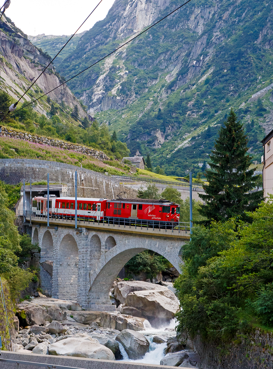Die MGB Deh 4/4 – 55 „Brig“ kommt am 01.08.2019 von Andermatt nach G�schenen hinab und �berquert hier die Reuss. 

Die Strecke G�schenen–Andermatt ist die Sch�llenenbahn, eine einspurige Zahnradbahn (Zahnstangensystem Abt) im Schweizer Kanton Uri. Sie durchquert die Sch�llenenschlucht der Reuss und weist eine Maximalsteigung von 179 Promille auf. Die Bahnstrecke wurde zwischen 1913 und 1917 durch die Sch�llenenbahn AG (SchB) gebaut. Die Sch�llenenbahn AG fusionierte 1961 mit der Furka-Oberalp-Bahn (FO), welche wiederum  zum 1. Januar 2003 mit der Zermatt-Bahn (BVZ), zur heutigen Matterhorn-Gotthard-Bahn (MG) fusionierte. 

Heute bef�rdert die Sch�llenenbahn im Jahr ca. 400.000 Reisende. Sie hatte in der Vergangenheit auch eine gro�e milit�rische Bedeutung. Sie versorgte die Festungsanlagen des R�duit im Gotthardmassiv. Die Bahnstrecke hat eine Gesamtl�nge von 3.770 Metern, davon sind 2.509 mit Zahnstange ausger�stet. 1.022 Meter der Strecke befinden sich in Tunneln und 1.110 Meter in Galerien. Die Bahn f�hrt durch f�nf Tunnel und f�nf sch�tzende Galerien. Vier Mal f�hrt die meterspurige Schmalspurbahn �ber eine Br�cke.

Auf der Sch�llenenbahn wurden urspr�nglich vier zweiachsige Elektrolokomotiven f�r kombinierten Adh�sions- und Zahnradbetrieb von SLM und BBC mit Bezeichnung SchB HGe 2/2 eingesetzt. Urspr�nglich liefen sie mit 1.200 Volt Gleichstrom. 1941 wurden sie auf 11.000 Volt Wechselstrom umgestellt. Die letzte dieser vier Lokomotiven wurde 1985 Sp�ter kamen kamen FO BCFhe 2/4 der Schweizerischen Lokomotiv- und Maschinenfabrik mit einem Antrieb der BBC zum Einsatz. ausrangiert. Heute (2019) befahren Deh 4/4 und Wagen der Matterhorn-Gotthard-Bahn die Strecke. Dabei befindet sich das Triebfahrzeug stets am talseitigen Ende, am Zugschluss l�uft ein Steuerwagen.
Die Sch�llenenbahn bietet einen st�ndlichen Pendelverkehr an und ist in den Fahrplan der SBB und der Matterhorn-Gotthard-Bahn vollst�ndig integriert.
