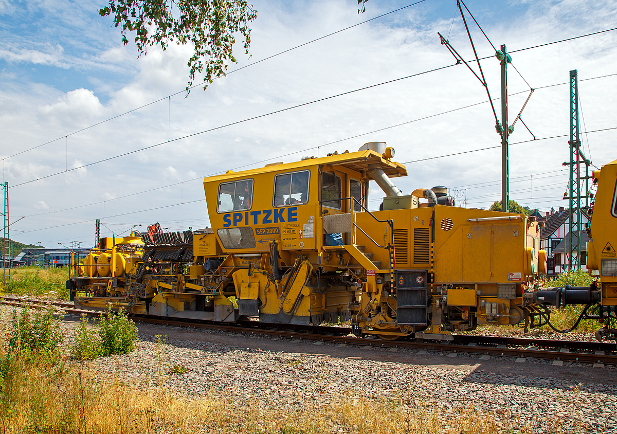 
Die Plasser & Theurer Schotterverteil- und Planiermaschine SSP 2000 der SPITZKE SE, Schweres Nebenfahrzeug Nr. D-SPAG 99 80 9125 007-1, abgestellt am 21.07.2018 in Wissen (Sieg).

Die Schnellschotterplaniermaschine SSP 2000 stellt den erforderlichen Regelbettungsquerschnitt in Gleisen und Weichen her. Die Maschine verfüllt, planiert und kehrt das Gleis. Sie verfügt über Besenwellen für alle Oberbauformen.

Funktionsmerkmale:
- Automatische Ausschwenkbegrenzungen der Flankenpflüge verhindern ein Überschreiten des Regellichtraumprofils
- Besenwellenschnellwechselvorrichtung
-  Zwei durchgehende Achsen als Triebachsen
- Durch Schraubenfedern und Stoßdämpfer wird eine ausreichende Absorption von Schwingungen und Stößen und eine große Laufruhe des Fahrzeuges erreicht
- Geschlossene schallisolierte Großraum-, Fahr- und Arbeitskabine am hinteren Teil der Maschine
-  Zwei waagerecht und senkrecht verstellbare Flankenpflüge im vorderen Teil der Maschine
- Mit Planierpflugeinrichtung für schwerste Schotterarbeiten – bestehend aus zwei voneinander unabhängig absenkbaren in Gleisrichtung laufenden Pflughälften
- Kehranlage inklusive einer Kehrbürste und einem Querförderband zur Verfüllung der Zwischenfächer bzw. Ableitung des überflüssigen Schotters auf das Querförderband
- Drehzahl des Bürstenantriebes kann bis max. 350 U/min stufenlos verstellt werden
- Schotterentfernung zwischen Schiene und Kleineisen durch zwei Kleineisenbürsten hinter der Vorderachse
- Ausgerüstet mit Sifa und Indusi


TECHNISCHE DATEN der SSP 2000:
Spurweite: 1.435 mm
Achsformel: A´A´
Länge über Puffer: 17.000 mm
Achsabstand: 10.000 mm
Eigengewicht: 40,3 t
Anhängelast: 60 t
Leistung: 400 kW
Höchstgeschwindigkeit: 100 km/h (Eigenfahrt und geschleppt)
Zugelassen zur Mitfahrt:  4 Personen
Kleinster befahrbarer Kurvenradius:  R 90 m (Arbeitsradius  120 m)     
Zugelassen für Streckenklasse: C2 oder  höher
Bremse: KE-GP mZ
Bremsgewichte: G = 26 t / P = 26 t
Tankvolumen: 2x 1.000l Diesel
Wasservorrat: 1.000 l (für Sprühnebel bei Staubanfall)

Besonderheiten: 5-fach verstellbarer Mittelpflug, Ausschwenkbegrenzung für Pflüge auf mehrgleisigen Strecken

Leistungsparameter
Arbeitsleistung bei Durcharbeitung des Gleises: max. 1.600 m/h
Arbeitsleistung bei Umbau des Gleises: max. 1.200 m/h
Arbeiten in Überhöhung: max. 180 m

Quelle: http://www.technikpark.com (SPITZKE SE), sowie Anschreibungen am Fahrzeug.
