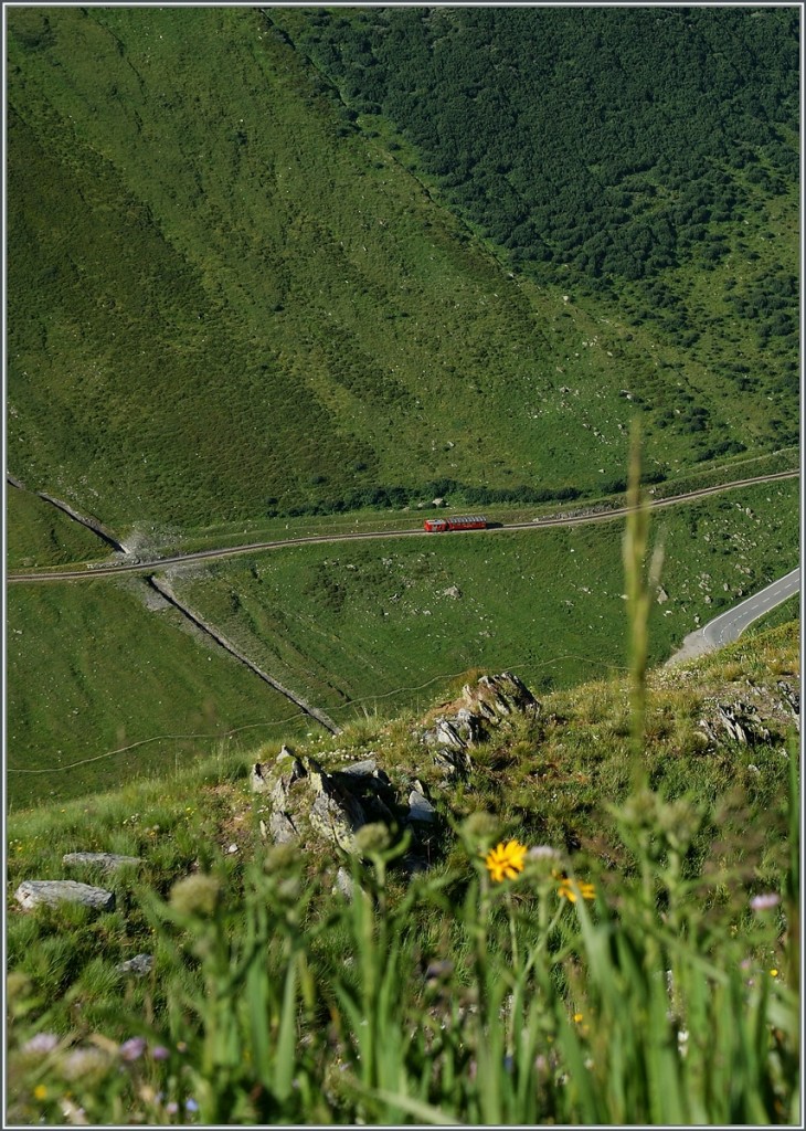 Eigentlich ein Bahnsuchbild, doch die paar Pixel DFB-Rot des Tm und B im Tal fallen sofort auf...
Ein Blick von der Furka Passs Strasse auf den Dienstzug auf dem Weg Richtung Realp. 
5. Aug. 2013