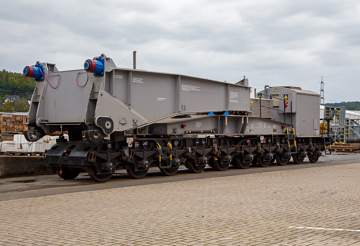 Eine Hälfte des 20-achsigern Tragschnabelwagen der Gattung Uaai 687.9 (84 80 9960 003-5 D-AMPR) der Amprion GmbH abgestellt am 03.10.2021 in Kreuztal auf dem Betriebsgelände der KAF (fotografiert vom Gehweg durch den Zaun). Der Trafo war bereits (oder war noch) auf einer Scherenhub-Kesselbrücken der Kahl Schwerlast GmbH verladen.

Die Amprion GmbH ist ein deutscher Übertragungsnetzbetreiber für den Strombereich. Das Unternehmen, welches als Teil des RWE-Konzerns entstand, beschäftigt etwa 1100 Mitarbeiter, sein Hauptsitz befindet sich in Dortmund.

Der Tragschnabelwagen wurde 1961 bei MAN unter der Fabriknummer 146523 gebaut. Es wurden 3 Stück der Bauart Uaai 687.9 hergestellt.

TECHNISCHE DATEN:
Spurweite: 1.435 mm (Normalspur)
Anzahl der Achsen: 20 in 4 Drehgestellen á 5 Achsen
Gattung/Bauart: Uaai 687.9
Länge über Puffer: 32.070 mm (Leerfahrt) / 41.140 mm (mit Trafo)
Drehzapfenabstand 1: 15.886 mm (Leerfahrt) / 24.956 mm (mit Trafo)
Drehzapfenabstand 2 (zw. den DG1+2 / DG 3+4): 7.500 mm
Achsabstand in den Drehgestellen: 4 x 1.500 mm = 6.000 mm
Laufraddurchmesser: 1.000 mm (neu)
Eigengewicht: 117 t
Maximale Ladegewicht: 250 t
Achsdruck: 5,85 t (Leerfahrt) / 18,35 t (mit Trafo)
Meterlast: 3,65 t/m (Leerfahrt) / 8,92 t/m (mit Trafo)
Höchstgeschwindigkeit: 90 km/h (Leerfahrt) / 40 km/h (Beladen)
Kleinster befahrbarer Gleisbogenhalbmesser: 75 m
Tragende Bauteile gefertigt aus: M St 52-3
Bremse: KE-G (LL)
Bremssohle: IP 116
Bauart der Handbremse: bodenbedienbare Handbremse 2 x 45 t