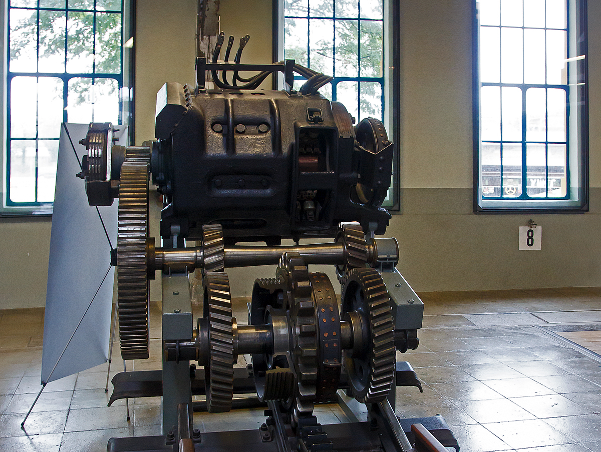 Elektrischer Zahnradantrieb der Bayerischen Zugspitzbahn (BZB) am 11.09.2022 in der Lokwelt Freilassing, vermutlich einer der drei Antriebe der Berglokomotive 11 der BZB, die seit 2008 als Denkmal beim Verkehrszentrum des Deutschen Museums in München steht.

Jeder der drei hintereinander geschalteten 500 V Gleichstrommotoren der Zugspitzbahnlok wirkt auf ein eigenes Triebzahnrad, dessen Drehzahl durch ein Getriebe (Zahnräder) auf 1:12,7 der Motordrehzahl herabgesetzt wird und dementsprechend wiederum die Kraft erhöht wird.

Die Bandbremsen beiderseits des Triebzahnrades dienen nur zum Anhalten des Zuges, die Bremsung bei der Talfahrt erfolgt ausschließlich durch die Elektromotoren. Die dabei erzeugte elektrische Energie wird aber nicht an den Fahrdraht abgegeben, sondern in Widerständen unter dem Dach der Lokomotive verheizt.

Auf einer Gesamtlänge von 18,7 km verbindet die Zugspitzbahn Garmisch-Partenkirchen mit der Zugspitze und überwindet dabei 1.945 Meter Höhenunterschied. Die Meterspurbahn wurde von Anfang an mit 1.500 Volt Gleichstrom elektrisch betrieben. Der Betrieb auf der 11,5 km langen Zahnradstrecke, die über 4,5 km durch den Fels der Zugspitz-Nordwand bis zum Schneefernerhaus führte, wurde am 8. Juli 1930 eröffnet. Mit einer Zahnstange des Systems Riggenbach muss die
Zahnradlokomotive eine Steigung von 25% überwinden, um auf Deutschlands höchsten Berg zu fahren.

TECHNISCHE DATEN:
Hersteller: Allgemeine Elektrizitätsgesellschaft, Berlin (AEG)
Baujahr: 1928
Gewicht: 4.600kg
Leistung: 510 kW (600 PS), bei 8 km/h
Dauerleistung: 360 kW (bei 9 km/h)
Geschwindigkeit: maximal 13 km/h
Spurweite: 1.000 mm
Zahnstangensystem: System Riggenbach
