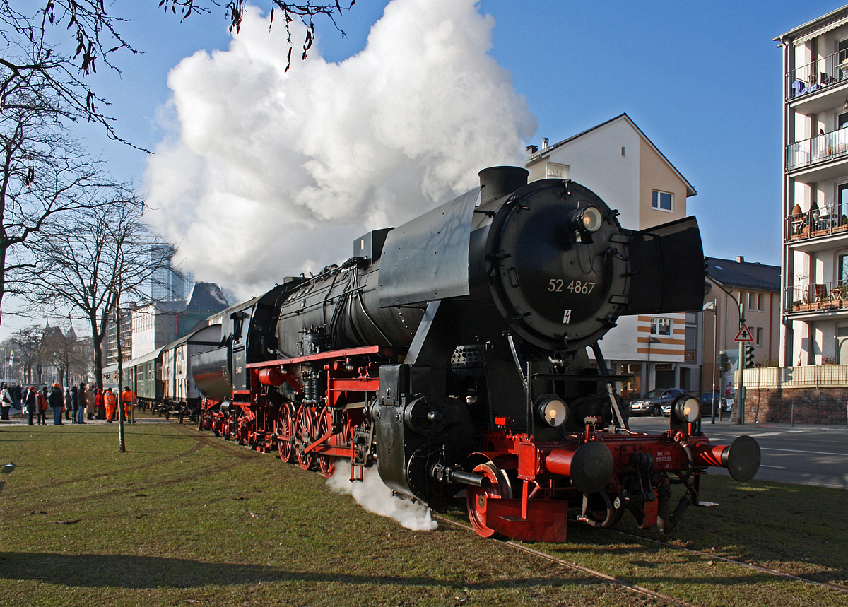 Fahrtag der Historische Eisenbahn Frankfurt e.V. auf der Frankfurter Hafenbahn am Mainufer am 30.01.2011 mit der HEF 52 4867 (90 80 0052 867-3 D-HEF), ex GKB 152.4867 (Graz-Köflacher Eisenbahn- und Bergbaugesellschaft), ex ÖBB 152.4867, ex DRB 52 4867.

Historische Dampflokomotiven im direkten Schatten von Hochhäusern. Das gibt es nur in Frankfurt am Main!  Die Historische Eisenbahn Frankfurt betreibt in Kooperation mit der städtischen Hafenbahngesellschaft (HFM) eine in Deutschland einmalige Museumseisenbahnstrecke am Frankfurter Mainufer. Abfahrt ist am Eisernen Steg, nur wenige hundert Meter vom Frankfurter Römer entfernt. Die Fahrt führt Sie von dort abwechselnd mitten durch die Parkanlagen am Mainkai zum Stellwerk Mainkur (Rundfahrt Osthafen) oder in die andere Richtung als  Straßenbahn  durch die Speicherstraße zum Übergabebahnhof Frankfurt Griesheim (Rundfahrt Westhafen). Hoffentlich sind auch diese Fahrten bald wieder machbar.

Die Güterzug-Dampflokomotive 52 4867 wurde 1943 bei Maschinenbau und Bahnbedarf AG in Potsdam-Babelsberg unter der Fabriknummer 13931 gebaut und an die Deutschen Reichsbahn geliefert. Nach dem Krieg blieb sie in Österreich  und wurde zur ÖBB 152.4867, 1970 kam sie zur GKB und 1980 kaufte die HEF die Lok.

So ist diese Lok noch eine Ur-52er (also keine Roko-Lok) mit Barrenrahmen.  Barrenrahmen, wie sonst allgemein bei der Deutschen Reichsbahn üblich, wurden von den Lokomotivfabriken bei den erste Lieferungen der Baureihe 52 noch eingebaut. Dies aber nur solange wie noch vorgefertigte Rahmen, für die zugunsten der BR 52 eingestellte Produktion, der in den Abmessungen identischen Baureihe 50, lagerte. Später wurden sie mit geschweißtem Blechrahmen gefertigt.

In Österreich befanden sich nach Kriegsende über 700 Lokomotiven, von denen nach Ausmusterungen, Rückgaben, Tauschen und Beschlagnahmen 1953 letztlich noch 313 für die Umzeichnung auf den neuen ÖBB-Nummernplan übrigblieben, die bei den Österreichischen Bundesbahnen unter Beibehaltung der Nummerierung als Reihe 52 eingereiht wurden, aber nach österreichischer Tradition mit einem Punkt zwischen Stamm- und Ordnungsnummer. Die 37 Maschinen der BR 52, die auf einem Barrenrahmen aufgebaut waren, erhielten die Reihenbezeichnung 152 (eine „1“ vor die 52).  Die GKB hatte zwischen 1968 und 1973 13 Barrenrahmenlokomotiven der Baureihe 152 gekauft. Zu ihnen zählte auch diese 52 4867, die nach ihrer Ausmusterung wieder nach Deutschland gelangte.

TECHNISCHE DATEN der Güterzug - Dampflokomotive 52 4867: 
Hersteller: Maschinenbau und Bahnbedarf A. G. Babelsberg
Fabriknummer: 13 931
Baujahr: 1943
Spurweite: 1.435 mm
Bauart: 1`E h2
Gattung: G 56.15
Länge über Puffer:  22.975 mm
Treibraddurchmesser: 1.400 mm
Laufraddurchmesser:  850 mm
Zylinderzahl: 2
Zylinderdurchmesser:  600 mm
Kolbenhub: 660 mm
Kesselüberdruck: 16 bar
Rostfläche: 3,89 m²
Verdampfungsheizfläche: 177,83 m²
Überhitzerheizfläche: 68,94 m²
Indizierte Leistung: 1.621 PS (1.192 kW)
Höchstgeschwindigkeit: 80 km/h (vorwärts / rückwärts)
Achslast max. : 15,3 t
Lokreibungslast:  75,5 t
Leergewichte: 75,9 t (Lok) / 18,7 t (Tender)
Dienstgewichte: 84,4 t (Lok) / 133,1 (Lok mit Tender)
Wasservorrat: 30 m³ ( 30.000 l)
Kohlevorrat: 10 t
Tender: Wannentender Typ  2'2' T 30 
Wannentender, sind  von Westwaggon, Köln, entwickelten Tender in Wannenform (daher die Bezeichnung), mit 2 zweiachsigen Drehgestellen und 30 m³ Wasserinhalt, sowie 10 Tonnen Kohleinhalt.
