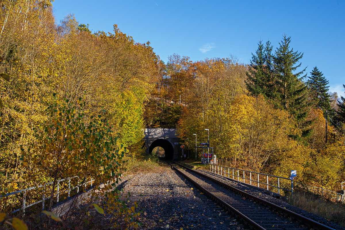 Herbstzeit im Hellertal.....
Der Bedarfs-Haltepunkt Herdorf-K�nigsstollen dahinter der Herdorfer Tunnel (137 m lang) bei km 88,6 der Hellertalbahn - KBS 462 (Bahnstrecke K�ln-Deutz – Betzdorf – Herdorf – Haiger – Gie�en). Vorm Tunnel das (Form) Vorsignal f�r das Einfahrtsignal vom Bahnhof. Es zeigt Vr 0 „Halt erwarten“ (Die runde Scheibe steht senkrecht, der Fl�gel zeigt er senkrecht nach unten). 

Die Hellertalbahn wurde als Teil der Deutz-Gie�ener Eisenbahn gebaut, die in den Jahren 1859 bis 1862 als Hauptbahn von K�ln-Deutz nach Gie�en in mehreren Etappen durch die C�ln-Mindener Eisenbahn errichtet wurde. Aufgrund der Verkehrsentwicklung und der milit�rischen Bedeutung 1870/71 wurde die Strecke 1871 zweigleisig ausgebaut. 

Damals war diese Strecke noch die Hauptstrecke. Der Niedergang der Hellertalstrecke begann im Jahre 1915, als die durch den Rudersdorfer Tunnel verlaufende Alternative er�ffnet wurde, erst ab da gab es eine direkte Verbindung zwischen Siegen und Haiger. Sowohl der hochwertige Reiseverkehr als auch der Gro�teil des G�terverkehrs nutzten nunmehr die direkte und g�nstiger trassierte Dillstrecke in Richtung Gie�en und weiter ins Rhein-Main-Gebiet. 

Im Hellertal wurde aber noch Eisenerz abgebaut und auf die Bahn verladen. Auch gab es in Herdorf eine Stahlh�tte. So war der Niedergang des Siegerl�nder Erzbergbaus Anfang der 1960er Jahre dann der gro�e Niedergang der Stecke. Zudem wurden die Ruhr-Sieg- , die Sieg- und die Dillstrecke elektrifiziert. So wurde die Strecke Mitte der 1960er Jahre als Nebenstrecke zur�ckgestuft, folgte im Jahre 1965 die Demontage des zweiten Gleises im Bereich Herdorf–Haiger. Im Jahr 1987 wurde das zweite Gleis auf dem Abschnitt Betzdorf–Herdorf stillgelegt. Hier im Bild kann man (links) noch das zweite Gleis erahnen.

Heute erinnern nur noch die durchgehende Kilometrierung von K�ln-Deutz und die gemeinsame Streckennummer an die alte Streckenf�hrung.
