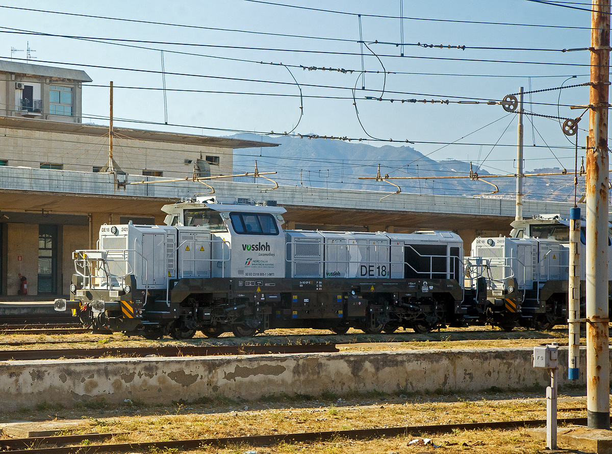 Neue Verschub-Lokomotiven fürs Trajekt-Manöver an den Ufern der Straße von Messina....
Die DE 18 2421  Barbara  alias 2318005-1 I-IMTI (92 83 2318 005-1 I-IMTI) der MIST - Mercitalia Shunting & Terminal S.r.l. íst am 20.07.2022 beim Bahnhof Messina Centrale abgestellt. 

Die vierachsige (Bo'Bo') dieselelektrische DE 18 wurde 2020 von Vossloh unter der Fabriknummer 550 2421 gebaut und im März 2021 von Kiel nach Italien überführt. Sie ist Eigentum der Vossloh Locomotives GmbH und an die MIST - Mercitalia Shunting & Terminal S.r.l. vermietet. Sie sind für Manöver von Zügen auf die Eisenbahnfähren, wobei im Einsatz konnte ich nur die RFI D.145.2000 sehen. Sie hat d. Z. nur die Zulassung für Italien. 

Die Vossloh DE 18 ist eine diesel-elektrisch angetriebene Lokomotive für den schweren Rangier- und Streckendienst mit der Achsfolge Bo'Bo'. Es handelt sich um die erste Lokomotive aus dem ehemaligen MaK-Werk Kiel seit der Einstellung der Produktion der DE 1002 im Jahr 1993. Etwa 60 % der Bauteile der DE 18 sind mit denjenigen der diesel-hydraulischen Variante G 18 deckungsgleich. Die Konstruktion des Fahrzeuges entspricht nach Herstellerangaben der Crash-Norm EN 15227. Einsatzbereit mit mehreren europäischen Länderzulassungen nach TSI hat sich die vierachsige Universallokomotive als hochmoderner Branchenstandard etabliert. Bei Geschwindigkeiten zwischen 17 und 120 km/h bietet die DE 18 kontinuierlich eine Leistung von 1.800 kW, was sie zur aktuell leistungsstärksten Mittelführerhauslokomotive auf dem europäischen Markt macht.

TECHNISCHE DATEN:
Spurweite:  1.435 mm 
Achsfolge:  B‘B‘
Länge über Puffer : 17.000 mm  
Drehzapfenabstand: 7.940 mm
Achsabstand im Drehgestell: 2.400 mm
Raddurchmesser:  1.000 mm (neu) / 920 mm (abgenutzt)
Größte Höhe:  4.310 mm  
Größte Breite:  3.080 mm
Höchstgeschwindigkeit: 120 km/h
Dieselmotor Typ:  MTU 12V 4000 R43L 
Dieselmotorleistung:  1.800 kW (2.447 PS) bei 1.800 U/min
Leistungsübertragung: elektrisch
Stromrichter : IGBT
Traktionsmotoren: 4 Stück Drehstrom-Asynchronmotoren vom Typ VEM DKLBZ 3510-4
Leistung am Rad: 1.440 kW
Anfahrzugkraft:  300 kN
Dauerzugkraft: 230 kN bei 24.2 km/h
Dienstgewicht:  90 t
Kraftstoffvorrat:  4.000 l
Elektrodynamische Bremsleistung: max. 1.450 kW  
Bremse: 2 x KE-GP-E mZ (D)
Kleinster befahrbarer Bogenradius:  55 m
Fährbootwinkel: 1° 30’ (bei dieser Lok wichtig)

Weitere Motordaten (MTU 12V 4000 R43L):
Dieselmotorart: 12 Zylinder -Viertakt-90°-V-Dieselmotor mit Abgasturboaufladung, Ladeluftkühlung und Common-Rail-Einspritzung
Motorhersteller: Motoren- und Turbinen-Union Friedrichshafen (MTU)
Motorhubraum: 57.2 l (Ø 170 mm Bohrung x 210 mm Hub)
Motorabmessungen: 2.386 x 1.562 x 2.015 mm
Motorgewicht: 6.613 kg (trocken)
Abgasvorschriften:  EU/2004/26 Stufe IIIA/prepared for stage IIIB  