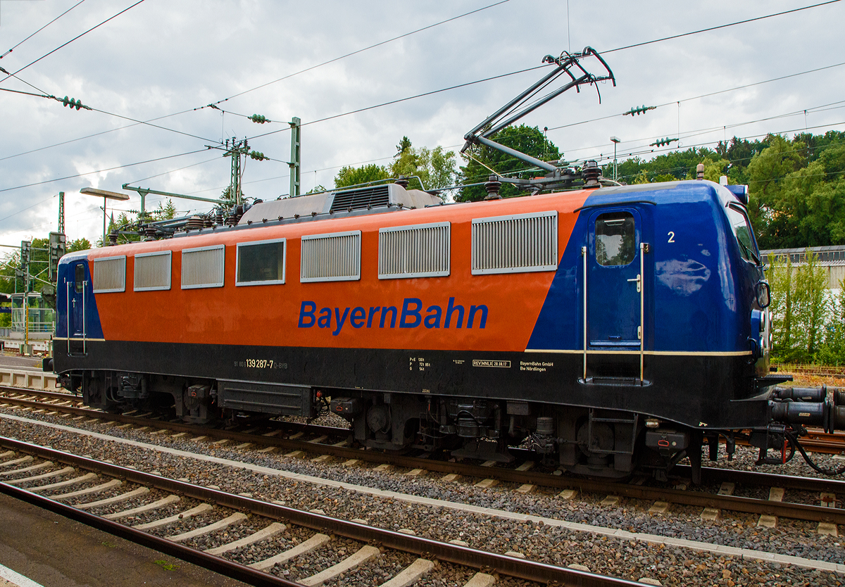 Noch ein Seitenblick.....
Die 139 287-7 (91 80 6139 287-7 D-BYB) der BayernBahn GmbH f�hrt am 09.06.2020, mit dem sogenannten  Henkelzug  (Langenfeld/Rhld. nach Gunzenhausen), durch Betzdorf (Sieg) in Richtung Siegen. 	

Die Lok wurde 1963 von Krauss-Maffei AG in M�nchen-Allach unter der Fabriknummer 18956 gebaut, der elektrische Teil ist von den Siemens-Schuckert-Werke (SSW) in Berlin. Als DB E10 287 wurde in Dienst gesetzt, mit der Einf�hrung des EDV-Nummernsystems wurde sie zum 01.01.1968 zur DB 110 287–0. Die Lok ist mit Einholmstromabnehmern ausger�stet, sie ist die letzte gebaute Kasten 110er. Zur 139er wurde sie erst 1994 nach einem Umbau, der Lokkasten wurde auf Drehgestelle der Baureihe 140 (E40) gesetzt und es folgte die Umzeichnung in DB 139 287-7. Zum Mai 2009 erfolgte die Z-Stellung bei der DB AG.

Zum 1.Oktober 2011 wurde die Lok durch die BayernBahn GmbH erworben und erhielt anschlie�end eine Untersuchung. Die Neulackierung in kobalt-blau/orange erhielt sie dann 2017.
