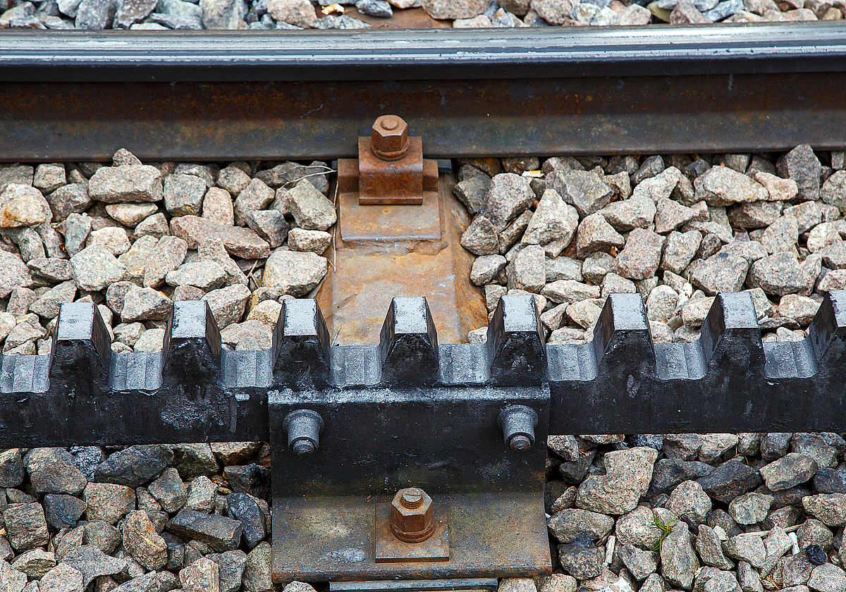 Nochmal im Detail, Gleis der Dolderbahn hier am 06.06.2015 an der Bergstation. 

Die Dolderbahn ist eine Privatbahn in der Stadt Zürich. Die Zahnradbahn erschließt (seit 1973, davor Standseilbahn) das Dolder-Gebiet im Quartier Hottingen ab der Haltestelle Römerhof am Römerhofplatz auf 444 Metern über Meer und endet in der Station Dolder auf dem Adlisberg auf 606 Metern über Meer. 

Die Bahn ist in der Spurweite1.000 mm (Meterspur) mit dem Zahnstangensystem von Roll ausgeführt. Die Zahnstangen sind hochliegend (über der Schienenoberkante). 
System Von Roll:
Die von der Firma Von Roll (heute Tensol) entwickelte Zahnstange ist nur dem Namen nach eine Lamellenzahnstange, nämlich eine einlamellige. Sie hat dieselbe Zahnteilung (100 mm) wie die Riggenbach'sche und die Strub'sche Zahnstange. Von letzterer unterscheidet sie sich in der Grundform: einfaches Breitflach-Profil anstatt einer Keilkopfschiene ähnliches Profil. Die Von Roll Zahnstange kommt in erster Linie bei Neubauten sowie als preisgünstiger Ersatz alter Zahnstangen nach den Systemen Riggenbach oder Strub zur Anwendung. Sie ist zwar dicker (30–80 mm, je nach Zahndruck) als eine der Lamellen nach Abt, doch ihre Biegsamkeit ist ausreichend, um flexibler als die Originale nach Riggenbach oder Strub anwendbar zu sein. Sie kann auch durchgehend verschweißt werden. Zur Befestigung auf den Schwellen dienen besondere Profilstahl-Sättel.

Die Systeme Von Roll, Riggenbach und Strub können miteinander kombiniert werden, d.h. in einer Zahnradbahn können Zahnstangen nach allen drei Systemen verbaut sein. Wobei man heute eigentlich aus Kostengründen nur noch Von Roll-Zahnstangen verbaut, da diese Lamellenzahnstangen auf einer automatischen Spezialmaschine präzis und wirtschaftlich hergestellt werden.