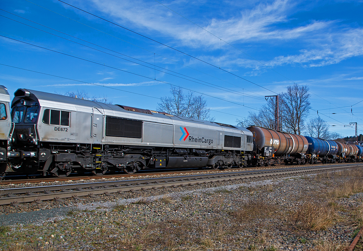 Nochmals im Detail...
Die RheinCargo DE 672 (92 80 1266 072-8 D-RHC), ex HGK DE 172, u.a. geschleppt von der RHC 2056 bzw. 185 588-1 (91 80 6185 588-1 D-RHC, die am 20.03.2021mit den beiden Class 66 (DE 670 und DE 672) und einem Kesselwagenzug, durch Rudersdorf (Kr. Siegen) über die Dillstrecke (KBS 445) in nördlicher Richtung fährt.

Die Lok wurde 2003 von EMD (Electro-Motive Division eine Tochter von General Motors) unter der Fabriknummer  20028453-5 gebaut, Eigentümer und Vermieter ist die Beacon Rail Leasing Ltd in London.

Die Lok ist eine EMD JT42CWR (auch bekannt als Class 66). Diese sind diesel-elektrische 6-achsige Schwerlastlokomotive. Sie besitzt einen 12 Zylinder 2-Takt-Turbodieselmotor vom Typ 12N-710G3B-EC, der einen Generator vom Typ EM AR8/CA6 antreibt der wiederum den Strom für die 6 Gleichstrommotoren vom Typ D43TR erzeugt welche die 6 Achsen angetrieben. Die Lokomotive wird von einem Board-Computer (EM 2000) überwacht und verfügt über verschiedene Mess- und Diagnosefunktionen. Die Lokomotive hat Zulassungen für Deutschland und Belgien.

Die JT42 CWR basiert auf der Entwicklung der 70er Jahre. Die Lokomotive erweist sich als eine grundsolide Baureihe, die dank dem einfachen Design und den Gleichstromantriebsmotoren einen zuverlässigen Posten in jeder Flotte darstellt. Die dreiachsigen HTCR-E Drehgestelle verfügen über gegenläufig radialgelenkte Endachsen, die Mittelachse ist seitenverschiebbar, diese ermöglichen den Betrieb dieser 6-achsigen-Lokomotive auf Strecken die in der Regel auf 4-achsige Lokomotiven eingeschränkt sind (Kleinster befahrbarer Radius 80 m). Die seitlichen Schiene-Kräfte sind dadurch auch gesenkt.
 
TECHNISCHE DATEN: 
Achsfolge: Co`Co`
Spurweite: 1.435 mm
Länge über Puffer: 21.349 mm
Drehzapfenabstand: 14.140 mm 
Breite: 2.692 mm
Höhe: 3.912 mm
Gewicht: 126 t
Dieselmotorleistung:  2.462 kW (ca. 3.200 PS)
Motorbauart:  V 12-Zylinder-2-Takt-Turbodieselmotor 
Motortyp:  12N-710G3B-EC
Drehzahl: 235 – 904 U/min
Tankinhalt: 6.400 l
Generator: AR8/CA6 
Fahrmotoren: 6 Stück D43TRC (DC / Gleichstom)
Leistung an den Rädern: 2.268 kW / 3.072 PS
Höchstgeschwindigkeit: 120 km/h
Anfahrzugskraft: 400 kN