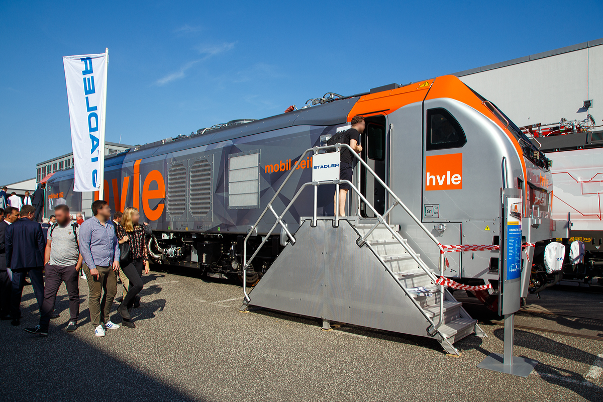 Stadler pr�sentierte auf der InnoTrans 2018 (hier 19.09.2018) in Berlin seine sechsachsige Eurodual eine Hybrid- bzw. Dual-Mode-Lokomotive. Hier in Form der f�r die Havell�ndische Eisenbahn AG (hvle) bestimmte 159 003-3 (90 80 2159 003-3 D-HVLE).
Leider war die ganze Messe so sehr �berlaufen, dass ein Foto ohne Menschen davor nicht m�glich war.

Die Lok wurde 2018 von Stadler Rail Valencia S.A.U. (Spanien) unter der Fabriknummer  3942 gebaut. Die Auslieferung an die hvle erfolgte 2019.

Bei den EURODUAL -Lokomotiven handelt es sich um kombinierte Diesel- und elektrische Lokomotiven f�r den Streckendienst im Personenverkehr und G�terverkehr, die von Stadler Rail bei Valencia in Spanien produziert werden. Zum 01. Januar 2016 hatte Stadler Rail das Werk bei Valencia von Vossloh �bernommen. Die Dual-Mode-Lokomotive l�sst sich dank einem elektrischen und einem dieselelektrischen Antrieb sowohl auf elektrifizierten als auch nicht elektrifizierten Eisenbahnlinien einsetzen. Die Lokomotiven z�hlen zu den gr��ten einteiligen Lokomotiven auf deutschen Gleisen. 

Die Konstruktion der Lokomotiven beruht auf Technik des ehemaligen Vossloh-Werks Valencia. Die Lokomotive setzt sich aus Komponenten der Vossloh Euro 4000 (Rahmen und Drehgestelle), der vierachsigen Diesellokomotive UKLIGHT (Class 68) (Tank, Dieselmotoranlage, L�fter, Abgasanlage) und der bimodalen, auf der UKLIGHT basierenden Class 88 (Haupttransformator, elektrische Ausr�stung) zusammen. Durch die Kombination dieser Elemente entstand die von der HVLE gew�nschte Konfiguration der Baureihe. Mit einer L�nge �ber Puffer von 23.020 mm sind die Lokomotiven eine der l�ngsten einteiligen Lokomotivbauarten eines deutschen Betreibers. Die EURODual-Lokomotive von Stadler ist eine Lokomotive mit einer beeindruckenden Leistung, sowohl im Diesel- als auch im Elektroantriebsmodus.

Die tragenden Elemente der Lok sind aus verschiedenen Stahlsorten hergestellt. Die Seitenw�nde des Maschinenraumes sind fest mit dem Rahmen verschwei�t. F�hrerh�user und Einstiegsr�ume sind separate Aufbauten. Das Dach besteht aus f�nf Segmenten, sie nehmen neben den Stromabnehmern auch andere Komponenten wie die K�hlerl�fter auf. Die F�hrerst�nde sind schallisoliert und klimatisiert. Der Lokf�hrer hat seinen Arbeitsplatz in der Mitte des F�hrerraumes.

Die Drehgestelle gelten trotz ihrer dreiachsigen Ausf�hrung als gleisschonend, da sie beim Bogenlauf noch geringere Querkr�fte als die zweiachsigen Drehgestellen der Bombardier TRAXX und Siemens Vectron aufweisen. Die Prim�rfederung erfolgt �ber Schraubenfedern, die Sekund�rfederung wird in Form von Gummi-Metall-Elementen und Schwingungsd�mpfern realisiert.

Der dieselelektrische Antrieb geschieht durch einen Caterpillar  V-16-Viertakt-Dieselmotor mit Abgasturbolader und Ladeluftk�hlung  vom Typ CAT C175-16 von mit einer Leistung von 2.800 kW, der elektrische Antrieb hat eine Leistung von 6.150 kW bei Speisespannungen von 25 kV / 50 Hz und 15 kV / 16,7 Hz.  Die Loks haben Wechselstrom-Antriebssystem mit IGBT. 1 Wechselrichter pro Achse und besitzen eine hohe Anfahr- und Dauerzugkraft.

Die Havell�ndische Eisenbahn AG (HVLE) ist der erste Kunde, an den die sechsachsigen Lokomotiven mit bimodalem Antrieb, die von Stadler f�r den europ�ischen Markt entwickelt und ausgeliefert wurden. Die Lokomotiven der Havell�ndische Eisenbahn sollen mit unterschiedlichen Fahrdrahtspannungen elektrifizierte und nichtelektrifizierte Strecken bedienen. Konkret betrifft es die mit 25 kV bei 50 Hz elektrifizierte R�belandbahn, das mit 15 kV bei 16,7 Hz versorgte deutsche Bahnnetz und die bislang nicht elektrifizierten Zulaufstrecken zur R�belandbahn. Bisher wurde dieser Verkehr elektrisch mit Lokomotiven der Reihe 185 und auf den nicht elektrifizierten Abschnitten mit Diesellokomotiven abgewickelt. Die Eurodual w�re die Universallokomotive f�r diese Dienste. Au�erdem ist sie bedeutend leistungsst�rker als die gegenw�rtig eingesetzten Maschinen und besitzt dazu noch die f�r die Steilstrecken notwendige Lokreibungslast. Nach der DR-Baureihe E 251 kommen damit wieder sechsachsige Elektro-Lokomotiven auf der R�belandbahn zum Einsatz. 

Die Zulassung der Lokomotiven f�r die HVLE erfolgte am 12. Februar 2020. Am 29. August 2020 wurde die (hier gezeigte)159 003 von DB Fernverkehr f�r Testfahrten auf der Schnellfahrstrecke K�ln/Rhein-Main angemietet. Der Testzug bestand aus zwei Triebwagen der Baureihe 407 sowie einer Lokomotive der BR 101. Diese sollte allerdings nur die Masse der Fahrg�ste simulieren.

TECHNISCHE DATEN, BR 159 der hlve:
Inbetriebsetzung: 2020
Spurweite: 1.435 mm (Normalspur)
Achsanordnung: Co’Co’ 
L�nge �ber Puffer: 23.020 mm
Breite: 2.900 mm
H�he: 4.290 mm
Treibdurchmesser: 1.067 mm (neu)
Eigengewicht: 123 t
Achslast: 21 t
H�chstgeschwindigkeit: 120 km/h
Elektrische Leistung am Rad bei 25 kV 50 Hz: 7.000 kW
Elektrische Leistung am Rad bei 15 kV 16.7 Hz: 6.150 kW
Leistung bei Dieselantrieb: 2.800 kW (3.807 PS)
Anfahrzugkraft: 500 kN
Elektrische Bremskraft	: 240 kN

Dieselmotor: 
Motorbauart: Caterpillar  V-16-Viertakt-Dieselmotor mit Abgasturbolader und Ladeluftk�hlung  vom Typ CAT C175-16
Motorleistung: 2.800 kW (3.807 PS)
Motornenndrehzahl: 1.800 U/min
Hubraum: 84,67 l (Bohrung � 175 mm / Hub 220 mm)
Motorgewicht (trocken): ca. 13.000 kg
Motorabmessung: 4.515 x 1.845 x 2.478 mm (l x b x h)
Abgasnorm: IIIB

Anzahl der Fahrmotoren: 6
Antrieb: elektrisch oder dieselelektrisch
Speisespannung: 25 kV 50 Hz und 15 kV 16.7 Hz
Tankinhalt Diesel: 3.500 l
Tankinhalt Urea: 400 l (f�r Abgasbehandlung selektive katalytische Reduktion („AdBlue“))
Bremse: KE-GP-E mZ (D)
Bremssystem Mechanisch: Pneumatisch 
Bremssystem Dynamisch: Regenerativ/Rheostatisch
Prim�r Federung: Schraubenfedern
Sekund�r Federung: Gummi-Metall Vertikal- und Horizontald�mpfer
Zugbeeinflussung: PZB, ETCS

Bei einer EuroDual die unter 1,5 kV DC Gleichstromoberleitung f�hrt liegt die 4100 kW, f�r eine Leistungssteigerung auf 6.000 kW ist dann auch der Dieselmotor i (im Gleichstrombetrieb) zuschaltbar.

Quelle: Stadler Rail, CAT und Wikipedia