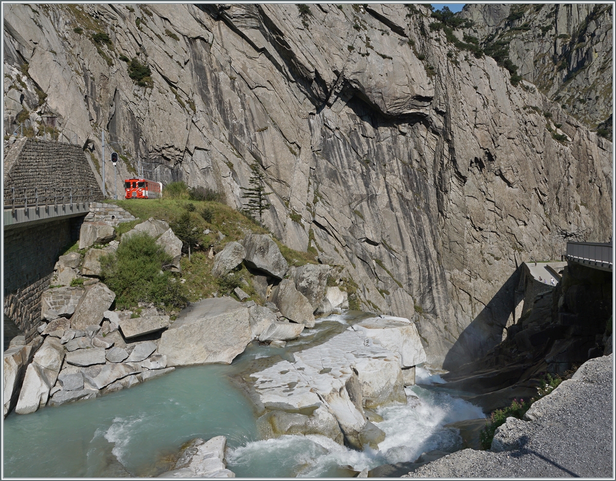 W�hrend die Strecke der MGB behutsam und schachte ins Talhinunter geht und hier im Tunnel verschwindet, tost das Wasser der Reuss den Abhang hinunter, zur Teufelsbr�cke, die am rechten Bildrand zu erkennen ist.

Dessen ungeachtet erreicht ein Zug von G�schenen her den Ausgang der Schlucht und erreicht in K�rze Andermatt. 

13. Sept. 2020