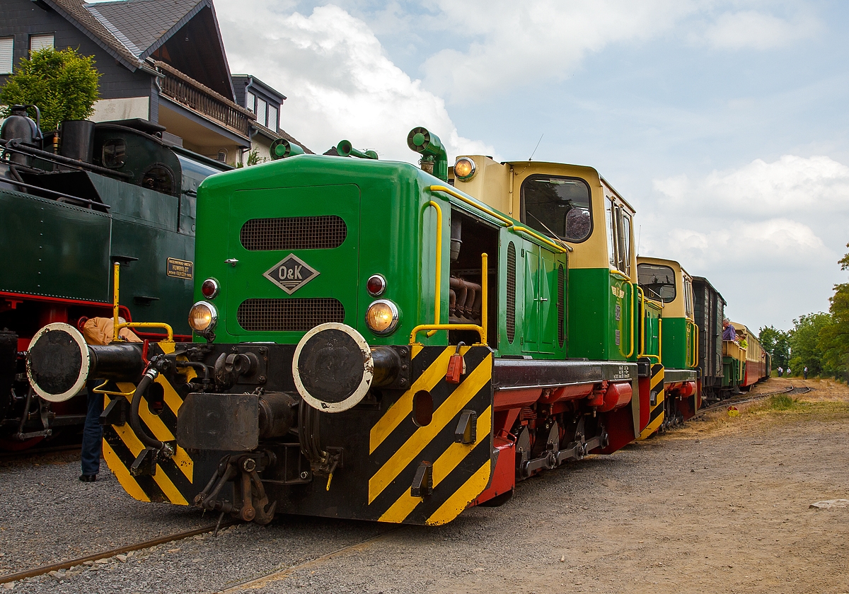 Wegen der folgenden 5,5 km langen 50 ‰ Steilstrecke ist für die Malletdampflok 11sm in Oberzissen Schluss, so wird hier nun umgespannt....

Nachdem die 11sm umgesetzt hat, fahren nun die Lok D2 und D1 der Brohltalbahn an den Zug heran, um diesen an den Haken zu nehmen und ihn weiter nach Engeln zu ziehen. 

Auffällig sind auch die, eigentlich für Schmalspurloks unüblichen Puffer. Die Brohltalbahn hat im Umladebahnhof Brohl ein Dreischienengleis Meterspur (1.000 mm) und Normalspur (1.435 mm), so können die Loks auch Normalspur-Wagons dort verschieben.
Die beiden baugleichen 1.000 mm Dieselloks wurden 1965 von O&K in Dortmund gebaut, die D1 unter Fabriknummer 26528 und die D 2 unter Fabriknummer 26529. 

Die Diesellokomotiven D1-D3:
Nachdem über 60 Jahre lang Dampflokomotiven auf der Schmalspurstrecke der Brohltalbahn ihren Dienst getan hatten, wurden 1965 zwei fabrikneue Dieselloks (D1 und D2) in Brohl angeliefert, die fortan die Dampfloks ablösten. Im Jahr 1967 folgte noch die dritte (D 3) Die beiden Loks mit den Betriebsnummern D1 und D2 sind bis heute betriebsfähig und ziehen jetzt vor allem Personenzüge auf der Strecke zwischen Brohl und Engeln. 

Das Dampflokzeitalter, das sehr lange den Alltag bei der Brohltalbahn bestimmt hatte, ging mit der Anschaffung der ersten beiden Dieselloks abrupt zu Ende. Die neuen Loks bewährten sich sehr schnell. Gegenüber den Dampfloks erforderte ihr Betrieb und Unterhalt viel weniger Aufwand, so mussten sie nicht vorgeheizt und ständig an zahlreichen Stellen geschmiert werden, sie waren innerhalb weniger Minuten betriebsbereit, ihr Führerstand war kein schmutziger und oft glühend heißer Arbeitsplatz mehr, sondern eine saubere, übersichtliche Kabine, von der aus der Lokführer sogar eine zweite, im Verbund fahrende Diesellok fernsteuern konnte.

Schon kurz nach der Anschaffung stellte sich heraus, dass die beiden dieselhydraulischen Loks D1 und D2 wegen ihrer Zuverlässigkeit und ihrem geringen Wartungsaufwand vier Dampflokomotiven ersetzen konnten. 1967 wurde deshalb im Dortmunder Werk des Maschinenbauers Orenstein & Koppel eine baugleiche dritte Lok bestellt. Nach vielen Jahren ist diese Lok mit der Betriebsnummer D3 inzwischen abgestellt. Die beiden älteren Loks D1 und D2, ursprünglich als Güterzug- und Rangierloks konzipiert, werden heute hauptsächlich für Personenzüge eingesetzt.

Typisch für die Brohltalbahn ist, dass die Loks wegen des besonders steilen Streckenabschnitts zwischen Oberzissen und Engeln mit drei verschiedenen Bremssystemen ausgestattet wurden und mit ihren drei Puffern auf jeder Seite sowohl Schmalspur- als auch Normalspur-Waggons auf den Gleisanlagen am Brohler Hafen rangieren können. Dort liegen Dreischienengleise, die sowohl von den Schmalspurfahrzeugen mit 1.000 Millimeter Spurweite, als auch von Loks und Waggons mit der Normalspurweite von 1.435 Millimetern befahren werden. Weil die Schmalspurloks dort im Verhältnis zu den Normalspurwaggons asymmetrisch stehen, sind auch die dafür vorgesehenen Pufferpaare an den Loks asymmetrisch. Die Mittelpuffer sind typisch für den Schmalspurbetrieb.

TECHNISCHE DATEN:
Typ: O&K MV 10 S
Achsformel:  C
Spurweite:  1.000 mm
Länge über Puffer:  7.140 mm 
Gesamtachsabstand: 1.900 mm (2 x 950 mm)
Breite: 2.500 mm
Höhe über Dachscheitel: 3.050 mm
Dienstgewicht: 32 t 
Höchstgeschwindigkeit: 28 km/h
Raddurchmesser: 750 mm
Motor: Luftgekühlter 90 Grad V12-Zylinder- Viertakt-Dieselmotor mit Abgasturbolader vom Typ Deutz BF 12L714
Dauerleistung: 300 PS (221 kW)
Motorhubraum: 19 l (Bohrung Ø 120 mm x Hub 140 mm)
Getriebe: Voith L203
Leistungsübertragung: dieselhydraulisch, vom Getriebe auf Blindwelle und von dieser über Kuppelstangen auf die Räder.
Bremse: KE-GPmZ , Kraftbremse und Vakumbremse
