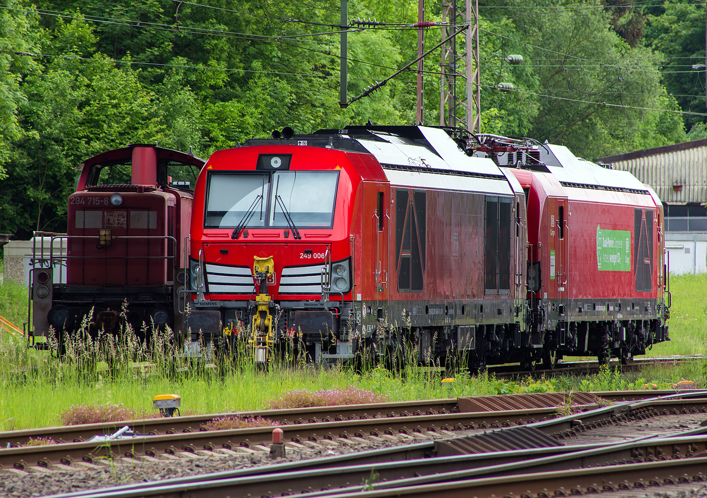 Abgestellt unter der Langenauer Brücke in Kreuztal (nahe dem Rbf) sind am 21 Mai 2024, von links nach rechts die Loks der DB Cargo AG:
Die remotorisierte V90 – 294 715-8, ex 294 215-9, ex 290 215-3. Die V90 wurde 1971 von MaK in Kiel unter der Fabriknummer 1000523 gebaut und als 290 215-3an die DB geliefert. Die Ausrüstung mit Funkfernsteuerung und die Umbezeichnung in DB 294 215-9 erfolgte 1996. Die Remotorisierung mit einem MTU-Motor 8V 4000 R41, Einbau einer neuen Lüfteranlage, einem neuem Luftpresser und Ausrüstung mit dem Umlaufgeländer erfolgten 2003 bei der DB Fahrzeuginstandhaltung GmbH im Werk Cottbus. Daraufhin erfolgte die Umzeichnung in die heutige 294 715-8.

Daneben die beiden neuen Zweikraftlokomotiven „Siemens Vectron Dual Mode light“ (BR 249), vorne die 249 006-8 (90 80 2249 006-8 D-DB) und dahinter die 249 003-5 (90 80 2249 003-5 D-DB). Beide Vectron DM light wurden 2022 von Siemens Mobility GmbH in München-Allach unter den Fabriknummern 23061 bzw. 23064 gebaut und waren erst durch Siemens Mobility GmbH als 90 80 2249 003-5 D-SDEHC bzw. 90 80 2249 006-8  D-SDEHC registriert/eingestellt. Erst nach der Abnahme durch die DB Cargo und den Verkauf an diese im März 2024 wurde sie durch die DB Cargo eingestellt. Die Loks der Baureihe 249 haben die Zulassung für Deutschland und eine Höchstgeschwindigkeit von 120 km/h.