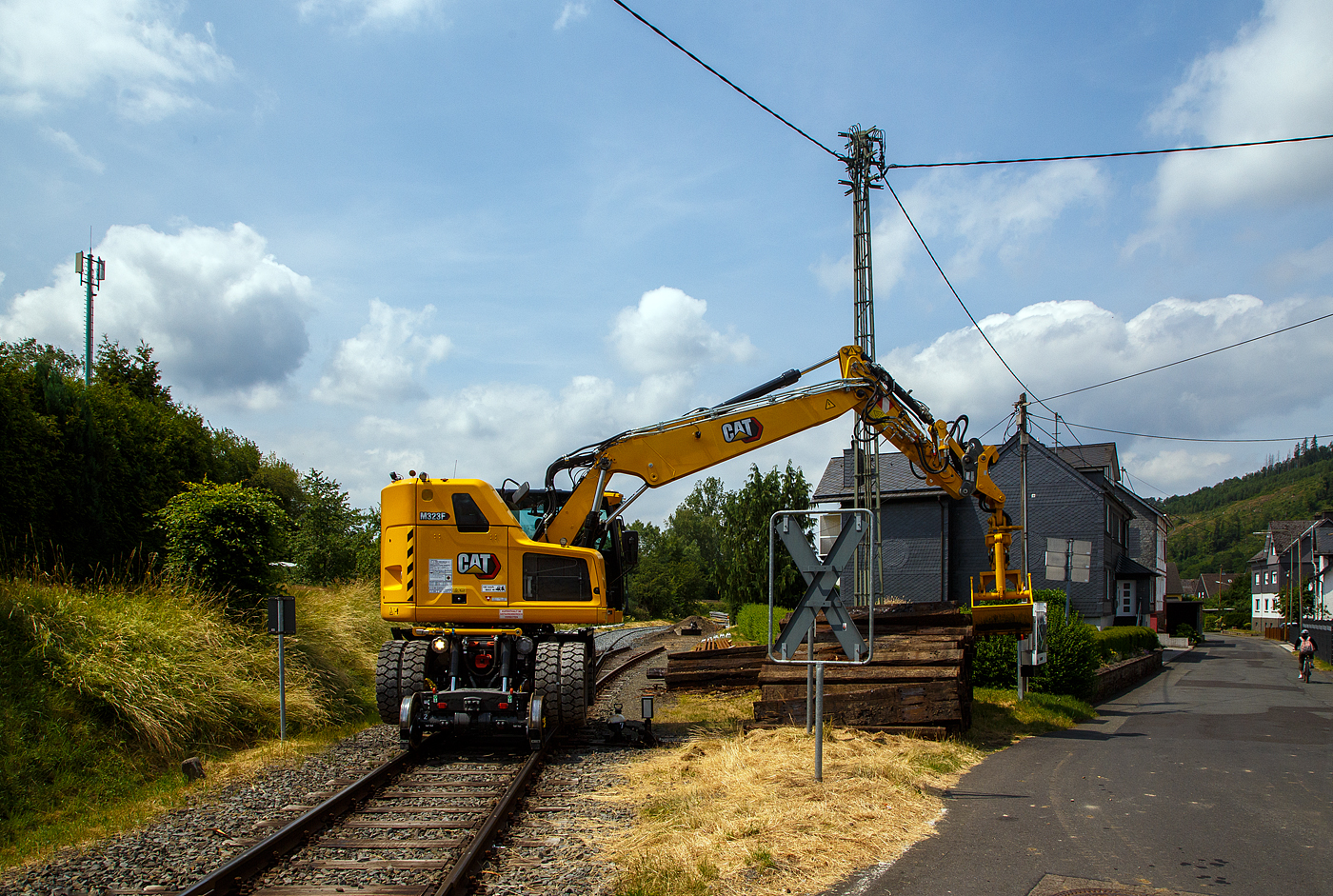 Bei dem Rangierbahnhof der KSW (Kreisbahn Siegen-Wittgenstein) in Herdorf der Betriebsst�tte FGE -Freien Grunder Eisenbahn (KSW NE447 / DB-Nr. 9275) wurden und wird der Unterbau der Gleise erneuert. Der Umbau erfolgt ohne gro�e Einschr�nkungen des Tagesablaufes. 

Hier stapelt der Caterpillar CAT M323F Zweiwegebagger mit hydrostatischem Schienenradantrieb (Serien-Nr. RH600 189), Kleinwagen Nr. D-ZBM 99 80 9902 521-0 der ZEPPELIN Baumaschinen GmbH (Garching), wohl ein Mietbagger, am 26.06.2023 bei der Talbahnstra�e Schellen.

Der Zweiwegebagger wurde 2022 unter der Fabrik-Nr. CAT M323FERH600189 gebaut.

Schienenradantrieb
Der CAT Zweiwegebagger mit hydrostatischem Schienenradantrieb (vom franz�sischen Spezialmaschinenbauer UNAC) ist konsequent f�r den Einsatz auf der Schiene entwickelt. Mit seinem kurzen Heck, dem innovativen Radantrieb und Bremssystem f�r alle Gleisr�der und dem ausgefeilten, aber einfach bedienbaren Kontrollsystem erschlie�t der Cat M323F den Anwendern entscheidende Vorteile.Anders als bei den bisher �blichen Zweiwegebaggern bewegt sich die Maschine auf der Schiene damit nicht abgesenkt auf den herk�mmlichen R�dern voran, sondern ohne Bodenkontakt auf den Schienenr�dern selbst. Die hohe Bodenfreiheit gew�hrleistet dabei, dass die Sicherheitseinrichtungen im Gleisbett beim Fahren nicht besch�digt werden. Mit dem Bremssystem im �lbad an beiden Achsen und den Scheibenbremsen f�r alle Gleisr�der gew�hrleistet der Cat M323F sicheren Vortrieb und kraftvolle Beschleunigung bis auf 20 km/h.

Klassische Zweiwegebagger sind vielfach noch mit Reibradantrieb ausgestattet. Die Reifen des Baggers werden dabei auf die Schienen oder Rolle gepresst und �bertragen so die Antriebs- und Bremskr�fte. Die Nachteile: hoher einseitiger Reifenverschlei� und oft Besch�digungen von Sicherheitseinrichtungen im Gleisbett.

Kurzheckbauweise
Durch den kompakten Aufbau und die geringe Heckausladung von nur
1.566 mm kann der Schienenverkehr auf dem Nachbargleis problemlos
weiterlaufen. Auch mit dem optional verf�gbaren Zusatzkontergewicht bleibt der kurze Heckschwenkradius unver�ndert. Trotz des kompakten Hecks bietet die Maschine mit dem robusten Verstellausleger auch auf dem Gleis viel Reichweite und hohes Hubverm�gen.

Die Konstruktionsweise sowie das bis zu 7,5 t schwere Kontergewicht stellen dabei sicher, dass die Maschine dennoch �ber eine hohe Standsicherheit, Reichweite und Hubverm�gen verf�gt.

Motor
Angetrieben wird der neue CAT Zweiwegebagger von einem Vierzylinder-Viertakt-Reihendieselmotor mit zwei Turboladern (Reihenturboaufladung) und Ladeluftk�hlung (TTA) vom Typ CAT C4.4 ACERT TTA, Emissionen EPA Tier 4 Final (USA) bzw. Stufe V (EU) und Dieselpartikelfilter.

Motordaten:
Leistung: 129,4 kW (173 PS)
Maximales Drehmoment: 750 Nm bei 1400 U/min
Nenndrehzahl 2.200 U/min
Bohrung x Hub: 105 x 127 mm
Motorhubraum: 4,4 l
Verdichtungsverh�ltnis: 16,5 :1
Ansaugsystem: Turboladern und Ladeluftk�hlung (TTA)
Verbrennungsverfahren: Direkteinspritzung
Abmessung: 845 x 742 x 868 mm
Gewicht (trocken) 420 kg

Der C4.4-Motor kann entweder mit extrem schwefelarmem Dieselkraftstoff oder mit B20-Biodiesel betrieben werden und erf�llt die Emissionsnormen der EU-Stufe IV. Die Leerlaufabschaltung, die automatische Motordrehzahlregelung und das bedarfsgesteuerte K�hlsystem verringern den Kraftstoffverbrauch.

TECHNISCHE DATEN:
Spurweite: 1.435 mm (Normalspur)
Eigengewicht: 23.400 kg
H�chstgeschwindigkeit: 19,9 km/h (20 km/h auf Stra�e)
Zul. Anh�ngelast: 220 t
Schienenbodenfreiheit: 195 mm
Stra�enbodenfreiheit: 360 mm
Zugkraft auf Stra�e: 104 kN
Zugkraft auf Schiene: 45 kN

Quellen: CAT, ZEPPELIN und Anschriften

