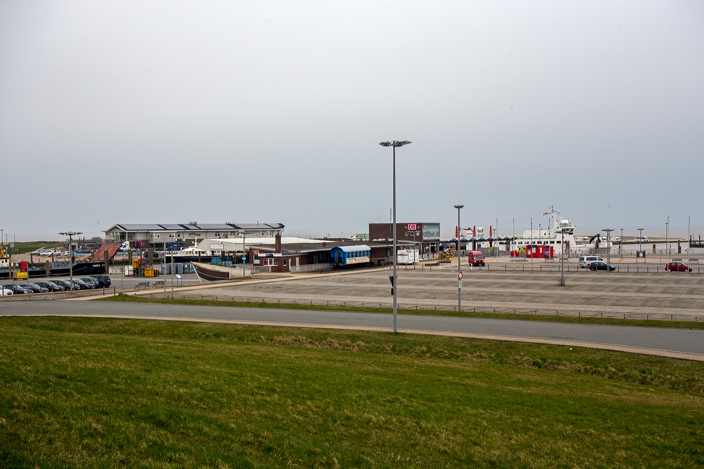 Blick am 11 März 2024 auf den ehemaligen Bahnhof Harle im Außenhafen Harlesiel, heute Fährterminal der SIW - Schifffahrt und Inselbahn Wangerooge (Teil der DB Fernverkehr AG). Hier war bis 1989 die Endstation der 20,1 km langen normalspurigen Bahnstrecke Jever–Harle, auch bekannt als „Tidebahn“ (ex KBS 10007). 

Übrigens ein Teil der KBS 10007 gibt es noch heute, dies ist die schmalspurige Wangerooger Inselbahn. Aber vor dem ehem. Bahnhof liegt auch noch ein Gleisstück der normalspurigen Bahnstrecke, mit einer 3. Schiene zur Aufnahme der beiden Wagen der Wangerooger Inselbahn. 

Die Bahnstrecke Jever–Harle war eine 20,1 Kilometer lange Nebenbahn im Nordwesten von Niedersachsen, die überwiegend dem Verkehr von und zu den Fährschiffen zur Insel Wangerooge diente. Im Januar 1990 wurde die Strecke stillgelegt und abgebaut. Da der Schiffsverkehr nach Wangerooge abhängig von den Gezeiten (der Tide) ist, hatten viele Zugpaare einen täglich wechselnden Fahrplan, weshalb diese Fahrten als Tidezug und die Strecke als Tidebahn bezeichnet wurden.

Die Strecke zweigte am Nordwest-Ende des Bahnhofes von Jever von der Ostfriesischen Küstenbahn ab und verlief weitgehend gradlinig und direkt neben der Landstraße nach Norden. Der wichtigste Zwischenbahnhof stand in Carolinensiel. Von dort führte sie bis in das Vordeichsgelände am Hafen Harle.

Der Bau der Bahn war vom Großherzogtum Oldenburg initiiert worden, um den Badebetrieb auf der einzigen oldenburgischen Nordseeinsel Wangerooge zu fördern. Gebaut wurde sie von der „Jever-Carolinensieler Eisenbahngesellschaft“, einer Aktiengesellschaft unter Führung des Bankhauses Erlanger & Söhne in Frankfurt am Main. Am 1. September 1888 wurde der Abschnitt Jever–Carolinensiel eröffnet; die Bahn endete jedoch nicht im damals preußischen Carolinensiel, sondern an der Friedrichsschleuse auf Oldenburger Gebiet. Der Anschluss zum Anleger Harle erfolgte am 1. Juli 1890. Der Betrieb wurde von Anfang an von den Großherzoglich Oldenburgischen Staatseisenbahnen (GOE) übernommen. Diese kaufte 1897 auch die verlustbringende Strecke. Gleichzeitig übernahm sie ein Seebäderschiff und errichtete die Inselbahn Wangerooge. 1956/1957 wurde der Hafen weiter in das Vordeichgelände verlegt und die Bahnstrecke verlängert.

Auf der Strecke überlagerte sich der nach festem Fahrplan verkehrende Zugverkehr Jever–Carolinensiel und der der Tidezüge Sande–Harle. 1944 verkehrten werktags sechs Zugpaare und ein Tidezugpaar, 1961 drei Zugpaare und ein bis zwei Tidezüge.

Der Betrieb war stets unrentabel. Im Jahr 1966 wurde der Verkehr im Winter eingestellt. Die Bedienung der Zwischenhalte endete 1968. Ab 1981 verkehrten Züge nur noch an verkehrsreichen Tagen, wobei sich der Fahrplan nach der Fähre richtete, der von Gezeiten abhing. Im Jahr 1987 musste das Umsetzgleis in Harle dem Parkplatzausbau weichen, so dass nur noch Schienenbusse verkehren konnten. Ein notwendiger Brückenneubau über das Tettenser Tief war Anlass, die Strecke stillzulegen. Zum Winterfahrplan 1987/1988 kündigte die Deutsche Bundesbahn die Einstellung des Personenverkehrs an. Am 27. September 1987 wurde der Reiseverkehr und am 25. September 1988 der Restverkehr eingestellt. Im Januar 1990 wurde die Strecke stillgelegt und abgebaut. Seitdem dienen große Teile der Trasse als Rad- bzw. Fußweg.

Das Bahnhofsgebäude und ein weiteres Bahngebäude in Carolinensiel werden privat genutzt, das Bahnhofsgebäude steht zudem heute unter Denkmalschutz. Das Bahnhofsgebäude in Harle dient als Verkaufsstelle für Fährtickets zur Insel Wangerooge. Vorhanden sind noch die ehemaligen Bahnhofsgebäude, heute privat genutzt, in Tettens und Garms.
