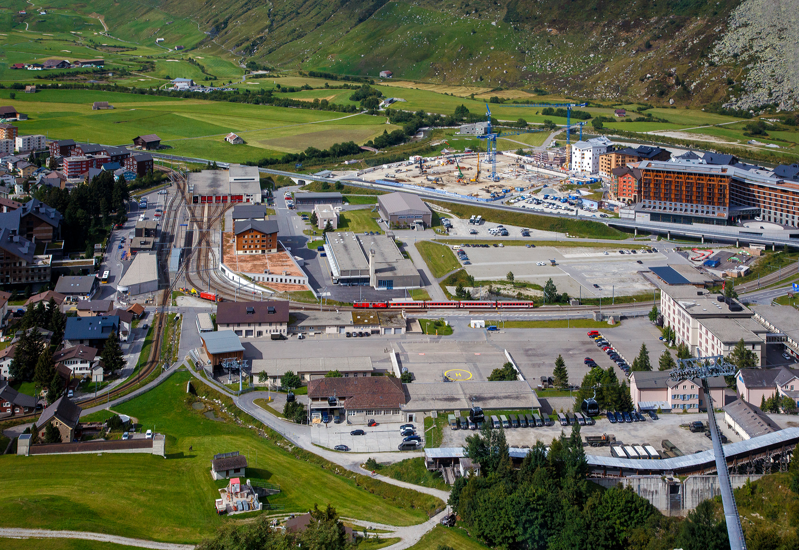 Blick aus einem vom Oberalppass kommenden  MGB Regionalzug auf den MGB Bahnhof Andermatt (auf 1436 m)  am 07 September 2021.

Nach rechts geht das Gleis der Schöllenenbahn nach Göschenen. Auf dem Nebengleis ist eine Deh 4/4 mit einem Zug abgestellt. Links unten ist das Gleis woraus wir gleich einfahren.

Auch links unten im Bild (rechts vom Gleis) die Talstation der im Dezember 2017 eröffneten 8er Gondelbahn (Ein-Seil-Umlaufbahn)   Gütsch-Express   (Andermatt – Nätschen - Gütsch). Sie fährt ab Bahnhof Andermatt über die neue Mittelstation am Nätschen zur Bergstation Gütsch. Die neue Anlage hat eine Förderleistung von 2.400 Personen pro Stunde, die Geschwindigkeit beträgt 5 Meter pro Sekunden und die Fahrzeit beträgt ca. 8 Minuten.