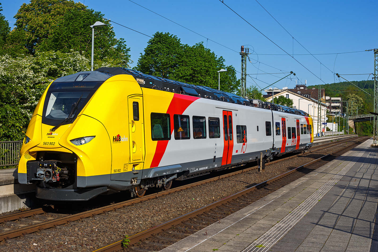 Das ist der neue Klimaschutz am Westerwald....
Einer der drei neuen zweiteiligen Hybridtriebz�ge (E/Akku) der BR 563 vom Typ SIEMENS Mireo Plus B der HLB (Hessische Landesbahn GmbH). Der HLB 563 802 / 563 902 (94 80 0563 802-8 D-HEB / 94 80 0563 902-6 D-HEB) f�hrt am 02 Mai 2025 auf Leerfahrt durch den Bahnhof Kirchen/Sieg in Richtung Betzdorf, hier hat er kurz Hp 0. Der Triebzug f�hrt hier sogar im Batteriemodus, denn es kein Stromabnehmer angehoben.  

Der zweiteilige SIEMENS Mireo Plus B wurden 2024/25 von SIEMENS in Krefeld gebaut und im April 2025 an die HLB ausgeliefert.

Auszug aus der Pressemitteilung der HLB:
Alternative Antriebe im Norden von Rheinland-Pfalz: Durchbruch beim Pilotprojekt mit Batteriez�gen im Westerwald / Zuschlag an Siemens Mobility f�r Mireo Plus B Fahrzeuge

Als Aufgabentr�ger f�r den Nahverkehr auf der Schiene im Norden von Rheinland-Pfalz setzt sich der SPNV-Nord gemeinsam mit seinen Projektpartnern von Bund, Land und Eisenbahnverkehrsunternehmen (EVU) f�r den Einsatz von alternativen Antrieben als Abkehr vom Dieselbetrieb ein.

Dabei konnte bereits im letzten Jahr f�r die Beschaffung der Fahrzeuge eine Unterst�tzung aus dem F�rderprogramm des Bundesministeriums f�r Digitales und Verkehr (BMDV) f�r alternative Antriebe gewonnen werden.

Als Besonderheit sollen im SPNV-Nord erstmalig die beiden Antriebstechnologien f�r die Dekarbonisierung des Schienenverkehrs, Wasserstoff und Batterieelektrik, nebeneinander im mehrj�hrigen Fahrgastbetrieb zum Einsatz kommen mit einer vollst�ndigen R�ckfallebene mit Dieselfahrzeugen.

Das betrifft auch den Pilotbetrieb mit drei batterie-elektrischen Fahrzeugen im Westerwald, der zum Fahrplanwechsel im Dezember 2025 geplant ist. Dieser sieht einen Fahrzeugeinsatz auf der RB 90 Limburg – Au – Siegen (Oberwesterwaldbahn und Siegstrecke) und auf der RB 29 Limburg – Siershahn (Unterwesterwaldbahn) durch die Hessische Landesbahn (HLB) vor. Bei diesem Pilotprojekt wurde j�ngst ein wichtiger Durchbruch erzielt:

Als Ergebnis der von der HLB daf�r durchgef�hrten Fahrzeugausschreibung hat Siemens Mobility jetzt den Zuschlag f�r drei zweiteilige Mireo Plus B Batteriez�ge erhalten. Das Fahrzeug mit seiner hohen Antriebsleistung ist f�r den anspruchsvollen Einsatz im Westerwald bestens geeignet. Der geplante Einsatz der drei Batteriez�ge auf den Linien RB 90 und RB 29 umfasst eine Jahresfahrleistung von fast 400.000 Zug-km und ersetzt drei Dieselfahrzeuge. Da die HLB emissionsfreien Bahnstrom bezieht, werden j�hrlich fast 1.150 Tonnen CO2 eingespart. Der Betrieb der Batteriefahrzeuge erfordert keine neue Infrastruktur, denn die Wendezeiten in Limburg von �ber 20 Minuten auf der RB 29 werden f�r die Aufladung der Fahrzeuge ausreichend sein. Bei den auf der RB 90 verkehrenden Batteriefahrzeugen erfolgt dies im elektrifizierten Abschnitt zwischen Au und Siegen. Die Oberwesterwaldbahn (Limburg – Au) ist mit der L�nge von rund 75 km und der zu �berwindende H�he von ca. 350 m derzeit in Deutschland die anspruchsvollste Strecke f�r den vorgesehenen Einsatz von Batteriez�gen.

Die Ausschreibung der Batteriefahrzeuge war so ausgestaltet, dass die Hersteller die M�glichkeit hatten, die Fahrzeuge in laufende Bestellungen zu integrieren, so dass eine schnelle Lieferzeit in Aussicht gestellt wurde.

Siemens Mobility baut f�r den Einsatz im Westerwald drei zweiteilige Mireo Plus B Batteriez�ge, die durch jeweils drei T�ren pro Seite einen schnellen Ein- und Ausstieg erm�glichen. Die Z�ge verf�gen f�r den Betrieb unter Oberleitung und zum Aufladen der Batterien �ber einen Stromabnehmer und verkehren auf den nicht-elektrifizierten Strecken im Batteriebetrieb. Die ger�umigen Fahrzeuge bieten den Fahrg�sten 126 Sitzpl�tze und 156 Stehpl�tze und sind mit einer speziellen Einstiegshilfe ausgestattet, die mobilit�tseingeschr�nkten Menschen das Bahnfahren erleichtert.

Die neuen Batteriez�ge werden auf der Oberwesterwaldbahn Limburg – Altenkirchen - Au - Siegen, und auf der Unterwesterwaldbahn zwischen Limburg – Montabaur – Siershahn unterwegs sein. Die Strecke der OWB betr�gt ca. 115 km, davon sind ca. 75 km ohne Fahrdraht. Es ist vorgesehen die Z�ge in Limburg und auf dem Teilabschnitt Au – Siegen nachzuladen. Auf der UWB betr�gt die nicht elektrifizierte Strecke ca. 35 km. Damit ist ein Zugbetrieb hin und zur�ck ohne Nachladen m�glich. Insgesamt werden die Z�ge �ber 50 Bahnh�fe anfahren.

Technik und Fahrzeugaufbau:
Die Triebz�ge werden nur mit elektrischem Antrieb angeboten. Die Fahrzeugplattform ist mit Jakobs-Drehgestellen und Einzeldrehgestellen, �hnlich wie bei den ICE 4 mit innengelagerten Rads�tzen lieferbar. Die Wagenk�sten werden in Aluminium-Integralbauweise hergestellt. Bei diesem zweiteiligen Triebzug ruht je ein Wagenkasten auf einen Triebdrehgestell SF 7500 als Enddrehgestell, sowie auf der H�lfte des mittigen Jakobs-Laufdrehgestell SF 7500. 

Die Triebz�ge werden im Siemens-Werk Krefeld gefertigt. Im M�rz 2020 erhielt Siemens Mobility den ersten Auftrag f�r eine zweiteilige Variante des Mireo Plus B die ihren Fahrstrom sowohl aus einer Batterie als auch aus der Fahrleitung erh�lt. Die Batterie kann im Stand und w�hrend der Fahrt aus der Fahrleitung geladen werden. Die Reichweite eines Mireo Plus B im Batteriebetrieb wird mit 80 bis 120 Kilometern angegeben.

Zum Einsatz kommen Lithiumtitanat-Akkumulatoren (LTO) von Toshiba, die unter den Wagenb�den verbaut sind. Diese haben eine hohe Zyklenfestigkeit auch bei hohen Ladestr�men, wie sie beim Bremsen und Anfahren auftreten – bei einer Laderate von 10C garantiert der Hersteller seit 2019 mindestens 15.000 Ladezyklen und seit 2022 mindestens 40.000 Ladezyklen.

Unterwesterwaldbahn/Oberwesterwaldbahn:
Am 7. Februar 2023 gab Siemens Mobility bekannt, dass die Hessische Landesbahn (HLB) f�r den Einsatz auf den Regionalbahn Linien RB 29 (Limburg (Lahn)–Montabaur–Siershahn) und RB 90 (Limburg/Lahn–Au/Sieg– Siegen) auf der Unterwesterwaldbahn bzw. Oberwesterwaldbahn drei Mireo Plus B bestellt habe. Der Einsatz ist ab Sommer 2025 geplant und soll im Rahmen eines Pilotbetriebes die Eignung von Triebz�gen mit alternativen Antrieben auf den topografisch anspruchsvollen Strecken demonstrieren. Der Betrieb soll nach Angaben der HLB j�hrlich fast 1.150 Tonnen Kohlenstoffdioxid einsparen.

TECHNISCHE DATEN:
Spurweite: 1.435 mm (Normalspur)
Achsfolge: Bo’-2’-Bo’
Fahrzeugl�nge �ber Kupplung: 46.560 mm
Drehzapfenanstand: 2 x 17.930 mm
Achsabstand im Triebdrehgestell (Enddrehgestell): 2.300 mm
Achsabstand im Jakobs-Laufdrehgestell: 2.600 mm
Drehgestellplattform: SF 7500 mit innengelagerten Rads�tzen
Raddurchmesser: 880 mm (neu) / 810 mm (abgenutzt)
Anzahl der T�ren je Seite: 3
Eigengewicht im betriebsbereiten Zustand: 92.891 kg
Installierte Leistung: 1.700 kW
Leistungs�bertragung: elektrisch
Motoren: 2 Drehstrom-Asynchronmotoren
H�chstgeschwindigkeit: 140 km/h 
Kupplung: Mittelpufferkupplung Schaku Typ 10
Sitzpl�tze: 126
Bremse: FT C-el-pn-R-A-E-Mg (D)
kleinster befahrbarer Gleisbogen: R 150 m (Normal) / R 100 m (Werkstatt)
Zulassungen: Deutschland (D)

Ein kleiner Nachteil gegen�ber den LINT-Dieseltriebz�gen ist mir aufgefallen, die Gesamt-Fensterfl�che ist geringer. Ich bin aber sehr gespannt auf den Betriebseinsatz und wie es l�uft.
