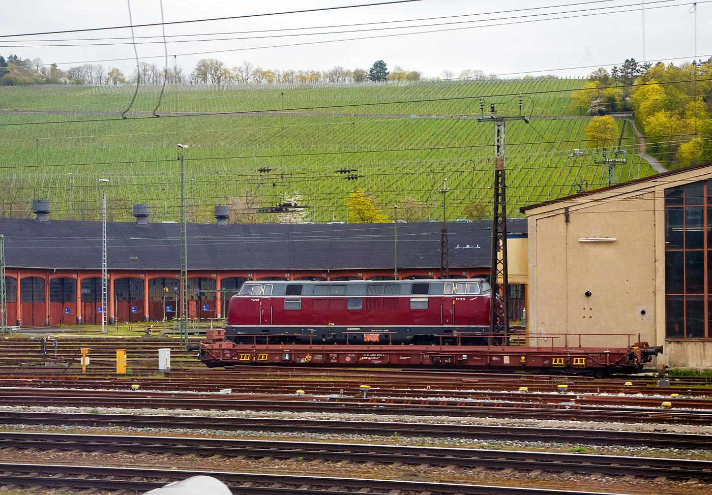 Der 8-achsiger Talbot-Niederflurwagen »Rollende Landstraße« (hier für den Bauzugdienst der DB), 81 80 4983 059-4 D-DBFWD der Gattung/Bauart Saadkms 690, der DB Fahrwegdienste GmbH, steht am 17.04.2023 in Würzburg vor dem Ringlokschuppen, aufgenommen aus einem Zug heraus. Dahinter steht die V 270.10 „Detlef T.“ alias 221 124-1 (92 80 1 221 124-1 D-SGL) der SGL - Schienen Güter Logistik GmbH (Dachau).

Der Wagen wurde 1981 von der Waggonfabrik Talbot in Aachen (den ältesten deutsche Hersteller von Schienenfahrzeugen) gebaut und an die Deutsche Bundesbahn geliefert. 

Nachdem Talbot 1979/80 vier Prototypen für den Huckepackverkehr gebaut hat, entsteht 1981 eine Serie von 200 Wagen. Die Deutsche Bundesbahn bezeichnet die Niederflurwagen erst als Saas-z 690. Die Wagen werden als  Rollende Landstraße  jeweils als Ganzzug in festen Relationen eingesetzt. Die wannenförmige Ladefläche liegt nur 450 mm über Schienenoberkante und kann von Lkw über den gesamten Zug hinweg befahren werden. Mittels Spezialkupplung werden die Wagen untereinander verbunden. Die Endwagen besitzen Kopfstücke, die mit  normalen  Zug- und Stoßeinrichtungen versehen sind und zum Be- und Entladen zur Seite geschwenkt werden. Dieser Wagen der DB Fahrwegdienste GmbH wird im Bauzugdienst eingesetzt (z.B. für den Tunnelspülzug 791 301, dann befindet sich ein Spül-LKW auf dem Wagen)

Die vierachsigen Drehgestelle der Bauart 690 besitzen Radsätze mit nur 360 mm Laufkreisdurchmesser. 

TECHNISCHE DATEN:
Spurweite: 1.435 mm
Länge über Puffer: 19.995 mm (mit Kopfstück) / 19.590 mm (ohne Kopfstück)
Drehzapfenabstand: 13.700 mm
Achsabstand in den Drehgestellen: 750 / 700 / 750 mm
Laufkreisdurchmesser: 360 (neu) / 335 mm (abgenutzt)
Ladelänge: 18.600 mm (mit Kopfstück) / 19.000 mm (ohne Kopfstück)
Eigengewicht: ca. 17.278 kg
Max. Zuladung: (S) 42,0 t ab Streckenklasse A
Zul. Geschwindigkeit: 100 km/h
Kleinster bef. Gleisbogenradius: R 150 m (R 80 m als Einzel Wagen)
Bauart der Bremse: KE-GP-A (D)
Drehgestell-Bauart: gummigefedert BA 690,  max. RSL 5,0 t, mit Scheibenbremsen