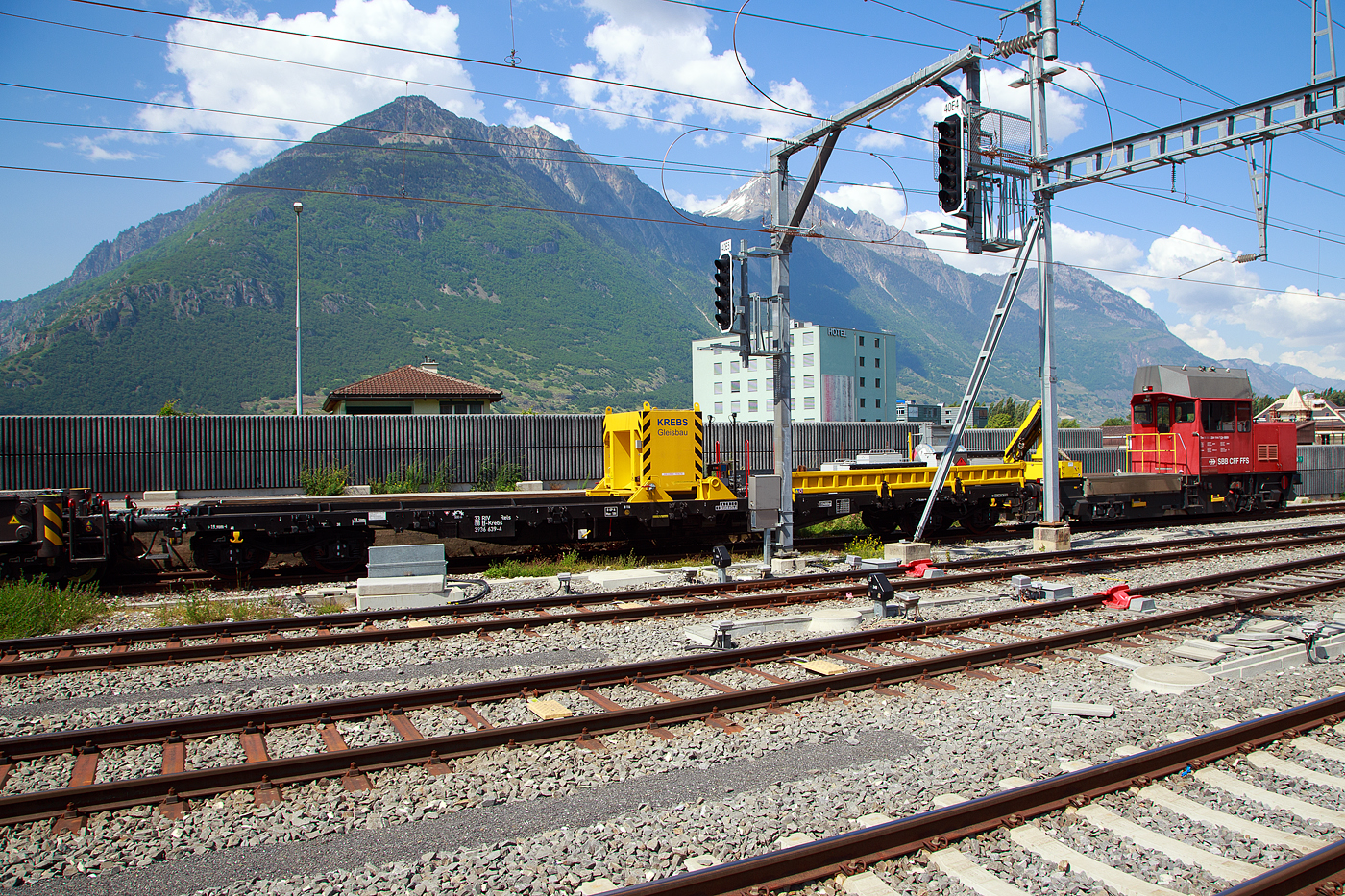 Der Gegenlastwagen 33 88 3936 639-4 B-Krebs ein vierachsiger Drehgestell-Flachwagen der Gattung Rels der Krebs GmbH & Co. KG, Bingen am Rhein (D) / Bern (CH) zum 130 t Eisenbahnkran vom Typ GOTTWALD GS 130.06 TT, D-KREBS 99 80 9419 008-4, ex 97 82 54 501 17-1, am 26.05. 2023 abgestellt beim Bahnhof Martigny. Auf dem Wagen liegt u.a. das Gegengewicht zum Kran. Links dahinter die „Ameise“ Tm 234 114-7 (Tm 98 85 5 234 114-7 CH-SBBI) der SBB Infrastruktur

TECHNISCHE DATEN von dem Gegenlastwagen:
Spurweite: 1.435 mm
Anzahl der Achsen: 4 (in 2 Drehgestellen)
L�nge �ber Puffer: 19.900 mm
Drehzapfenabstand: 14.860 mm
Achsabstand im Drehgestell: 1.800 mm
Laufraddurchmesser: 920 mm (neu)
Ladel�nge: 18.500 mm
Eigengewicht: 23.400 kg
Maximale Nutzlast: 56,6 t (ab Streckenklasse C)
H�chstgeschwindigkeit: 100 km/h
Bremse: O – GP-A (LL)
Bremssohle: IP 116
Intern. Verwendungsf�higkeit: RIV