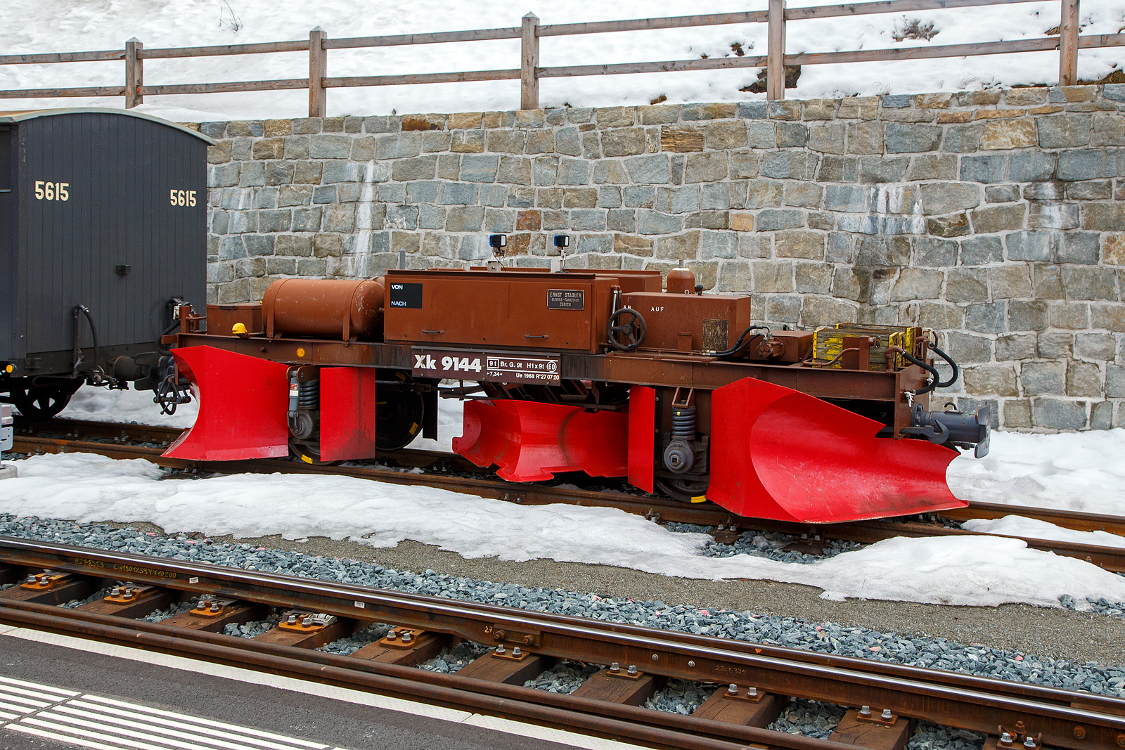 Der RhB Spurpflug Xk 9144 (Baujahr 1968 bei Ernst Stadler) abgestellt am 21.03.2023 im Bahnhof Pontresina.

Neben der Erneuerung des Bestandes an Schneeschleudern wurde ab Mitte der sechziger Jahre auch der Park der Schnee- und Spurpflüge modernisiert. Beschleunigt wurde die Entwicklung durch die Tatsache, dass mit den alten bemannten Pflügen immer wieder Unfälle passierten. Die alten Fahrzeuge, die nur geschoben werden konnten, besaßen einen manuell zu bedienenden heb- und senkbaren, unter Schienenoberkante reichenden Spurpflug. bei schlechter Sicht wurde der Spurpflug bei Wegübergängen und ähnlichen Hindernissen oft zu spät angehoben, und Entgleisungen mit Personenverletzungen und Materialschäden waren die Folge. Seitens des Bahndienstes rief man daher nach einem unbemannten, vom Führerstand der Schublokomotive aus fernsteuerbaren Spur- und Schneepflug.

1966 wurde dann der erste Prototyp-Pflug gemeinsam mit der Firma Ernst Stadler (heute Stadler Rail AG) speziell für die Bedüfrnisse der RhB entwickelt und gebaut, der X 9141. er war als Zweirichtungspflug konzipiert, kann also bei vorwiegender Räumung zwischen den Schienen auch gezogen werden. Neben kräftigen Stirn-Schneepflügen besitzt er einen hydraulisch senk- und hebbaren Spurpflug zwischen den Achsen. Der Öldruck für die Hydraulik wird in einem Pumpenaggregat auf dem Fahrzeug selbst mittels Achsantrieb erzeugt. Die Steuerung des Spurpfluges erfolgt über ein Steuerkabel mit Schaltkasten aus dem Führerstand der Schub- oder Zuglokomotive. Damit wird nicht nur Personal eingespart, es werden vor allem auch harte und gefährliche Arbeitsbedingungen eliminiert. Die eher konservativen Bahnmeister waren gegenüber dem neuen „Vehikel“ anfangs sehr skeptisch. Der Pflug X 9141 wurde dann aber immer beliebter, so dass 1968 drei weitere und bis 1989 nochmals drei Spurpflüge beschafft wurden, die sich vom Prototyp nur in Kleinigkeiten unterscheiden. Auch die FO stellte 1976 ein derartiges Fahrzeug in Dienst. Die alten Schneepflüge der RhB wurden daraufhin fast alle nach und nach verschrottet oder verkauft. Die modernen hydraulischen Pflüge sind über das ganze RhB-Netz verteilt. Besonders häufig müssen sie auf der Berninabahn eingesetzt werden, die stark mit Schneeverfrachtungen durch Wind zu kämpfen hat.

TECHNISCHE DATEN:
Hersteller: Ernst Stadler, Zürich
Baujahr: 1968
Spurweite: 1.000 mm
Gewicht: 9.40 t
Länge über Puffer: 7.340 mm
Achsabstand: 3.300 mm
Geschwindigkeit: 60 km/h
