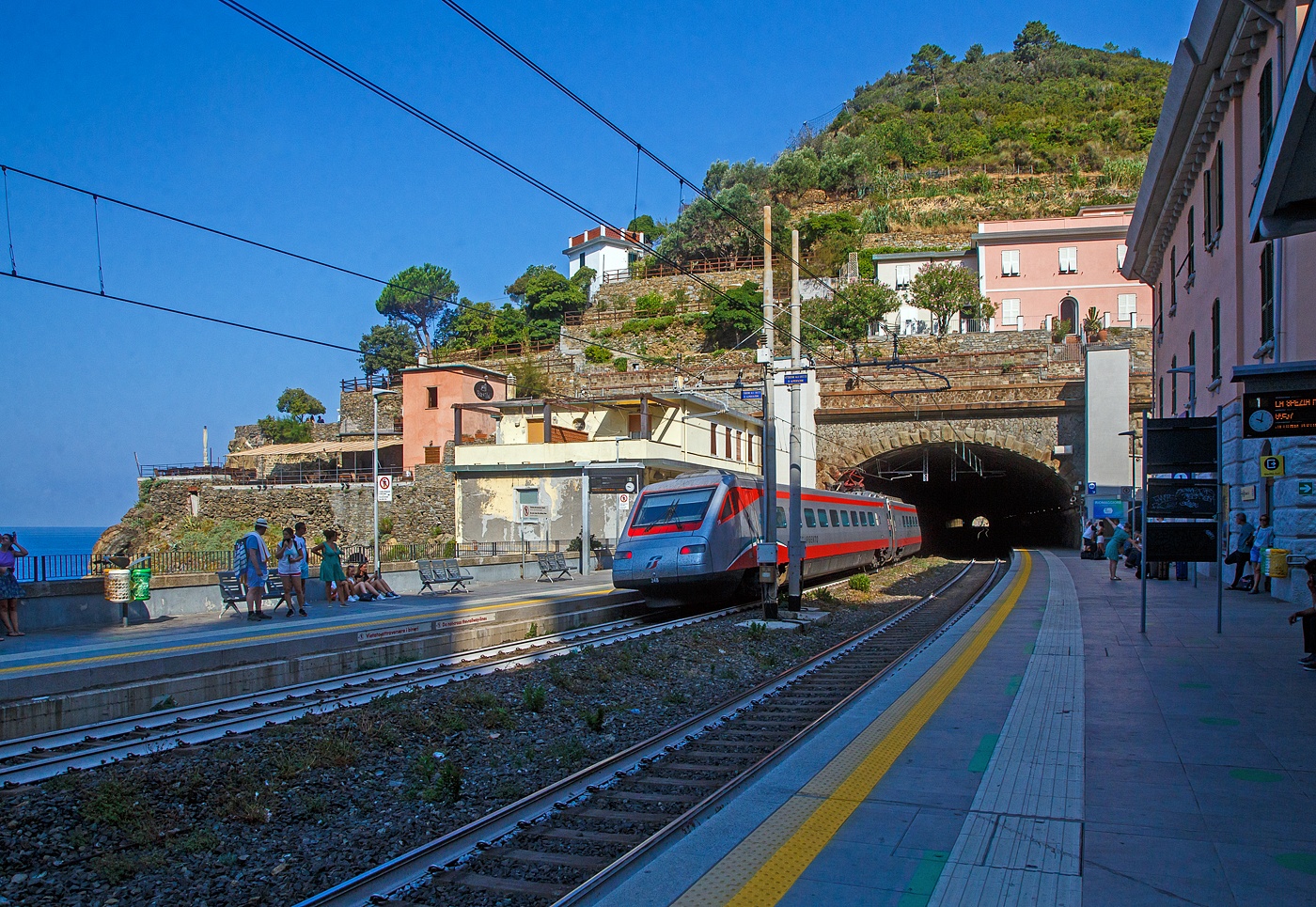 Der Trenitalia Frecciargento ETR 485 - 34 (Pendolino) fährt am 22.07.2022 durch den Bahnhof Riomaggiore in Richtung Genova.

Riomaggiore ist das südlichste der fünf Dörfer der Cinque Terre (Fünf Ortschaften) und verfügt, wie die anderen Dörfer, über einen Bahnhof an der Bahnstrecke Pisa–Genua (RFI Strecke-Nr. 77 / KBS 31 La Spezia–Genua), die den Ort mit den Nachbardörfern und mit La Spezia und Levanto verbindet. Der Bahnhof von Riomaggiore liegt am nordwestlichen Ortsrand, nur drei bis vier Wagenlängen befinden sich unter freiem Himmel, der Rest der Bahnsteige ist in den beiden Tunneln (davor und dahinter). Der Ortskern wird mittels eines in einem Eisenbahntunnel verlaufenden Fußpfades angebunden.

Hier mit Blick auf den nördlichen Tunnel (in Richtung Levanto). Rechts das Empfangsgebäude. Rechts und links vom Tunnelportal die Aufzüge (Lifte) vom einen zum anderen Bahnsteig für den barrierefreien Übergang. Es gibt auch eine Unterführung mit Treppen. 

Man kann auch mit dem Lift über den Tunnel fahren und geht dann nach links wo dann die Via dell'Amore beginnt. Dies ist ein in den Fels gehauener Fußweg zum nahe gelegenen Manarola, mit malerischen Aussichten (gegenwärtig aber gesperrt).