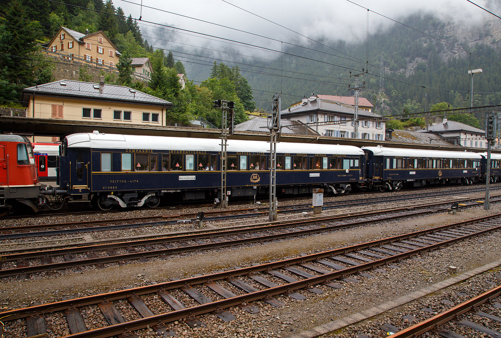 Der VSOE Schlafwagen Nr. 3553 – VSOE Voiture-Lits / Carrozza-Letti N° 3553 (F- VSOE 61 87 06-70 553-9 [P]) im Zugverbund vom Venice Simplon-Orient-Express am 02 August 2019 beim Halt im Bahnhof Göschenen (CH), leider bei Regen.

Der Schlafwagen, wurde 1929 von EIC - Entreprises industrielles des Charentes (EIC, heute zu Alstom gehörend) in Aytré (F), als CIWL Typ Lx 18 (Schlafwagen mit Schlafwagenschaffnerabteil), gebaut und als Schlafwagen Nr. 3553 an die CIWL - Compagnie Internationale des Wagons-Lits geliefert. 1943 wurde er zum in den Typ LX 20 (zehn Zweibettabteile) umgebaut. Im Jahr 1980 wurde er an die VSOE (Venice Simplon-Orient-Express Ltd.) verkauft. Hier wurde der Wagen überholt und technisch modernisiert, unter anderem mit Klimaanlagen. Bei den VSOE-Wagen wurde ein Schlafwagenabteil zum Abteil für den Schlafwagenschaffner hergerichtet, die Wagen werden seitdem (wieder) als Typ Lx 18 bezeichnet. 

Zwischen 2003 und 2006 wurde die Wagen der VSOE wieder modernisiert und erhielten unter anderem moderne Drehgestelle von Bombardier sowie neue Klimaanlagen. Durch die neuen Drehgestelle sind die Wagen seitdem für 160 km/h zugelassen. 

TECHNIK
Mit der Einführung von Ganzstahlwagen ging die CIWL dazu über, von Ausnahmen abgesehen alle Fahrzeuge auf einem einheitlichen Rahmen mit 23.452 mm Länge über Puffer und einem Drehzapfenabstand von 16.000 mm aufzubauen. Die Fahrzeugbreite beträgt 2.850 mm, die Höhe über Schienenoberkante 4.000 mm. Auf dieser Basis entstanden neben dem Typ Lx auch die Schlafwagen der Typen S, Y und Z. Die gleichen Rahmen wurden auch für Speisewagen und Pullmanwagen verwendet, sie bestehen aus drei Längsträgern mit Querverbindungen und zwei Gussstahlblöcken an den Enden zur Aufnahme der Zug- und Stoßvorrichtungen. Auf dem Rahmen sind die Seitenwände und Fußböden sowie die beiden Zustiegsplattformen aufgebaut. Das Gewicht des Typs Lx beläuft sich auf 53 Tonnen (heute 57 t). Als Drehgestelle erhielten die Wagen ursprünglich Schwanenhals-Drehgestelle mit Rollenlagern, auch als Pennsylvania-Drehgestelle bezeichnet. Im Laufe der Jahre wurden diese teilweise durch neuere Drehgestelle oder andere Bauarten ersetzt. Ursprünglich waren die Wagen lediglich für 130 km/h zugelassen, nach dem Krieg wurde die Geschwindigkeit auf 140 km/h angehoben. Die mit neuen Drehgestellen modernisierten Wagen des VSOE sind für 160 km/h zugelassen.

Die CIWL rüstete alle Wagen neben einer über die Heizdampfleitung des Zuges versorgten Dampfheizung mit einer unabhängig zu betreibenden Kohleheizung aus, die durch den Schlafwagenschaffner bedient wurde und bei längerem Stillstand eines Zuges zum Einsatz kam. In den Nachkriegsjahren erhielten viele Fahrzeuge außerdem elektrische Heizleitungen. In jedem Abteil befand sich zur Belüftung ein Ventilator, die Wagen der VSOE wurden mit Klimaanlagen ausgerüstet.

Es gab kein gesondertes Abteil für den Schlafwagenschaffner, dieser nächtigte auf einer an einem Ende des Wagens aufgeklappten Liege im Gang. Vorräte für die Versorgung der Fahrgäste befanden sich in Schränken an den Wagenenden. An einem Ende war ein WC untergebracht. Jeweils zwei der Abteile (mit Ausnahme der beiden äußersten Abteile) ließen sich mittels einer verschließbaren Tür zu einer größeren Suite verbinden. Die in den historischen Luxuszügen eingesetzten, noch erhaltenen Wagen des Typs sind teils umfassend modernisiert und umgebaut worden. Bei den im VSOE eingesetzten Wagen wird eines der Abteile für den Schaffner genutzt. Die Wagen besitzen zudem moderne Klimaanlagen.

TECHNISCE DATEN:
Spurweite: 1.435 mm (Normalspur)
Anzahl der Achsen: 4 in zwei Drehgestellen
Länge über Puffer: 23.452 mm
Drehzapfenabstand: 16.000 mm
Achsabstand im Drehgestell: 2.500 mm
Eigengewicht: 57 t
Höchstgeschwindigkeit: 160 km/h (ursprünglich 140 km/h)
Betten- und Sitzplätze: 18 (in 9 Zweibettabteilen) plus Schaffnerabteil 

DER HEUTIGE WAGEN 3553 - L'Observatoire
Im Jahr 2023 entwarf französische Künstler JR das Innere des neuen Privatwagens 3553 - L'Observatoire (Privatwagen) des Venedig Simplon-Orient-Express, der so 2023/24 umgebaut wurde und nun die UIC-Nummer F- VSOE 61 87 76-70 000-6 [P] trägt. Jetzt ist es ein Privatwagen mit einem Schlafzimmer für zwei Personen, einem Wohnzimmer, einer Bibliothek, einer Teekammer und einem Badezimmer mit freistehender Badewanne. Das Fahrzeug wurde im April 2024 auf der Biennale in Venedig ausgestellt, um erste Eindrücke zu liefern, und es läuft seit 2025 im Zug des Venice Simplon-Orient-Express. Ich würde ich gerne mal selbst von innen sehen. 

L’Observatoire, das sich über einen ganzen Wagen an Bord des Venedig Simplon-Orient-Expresss entfaltet, ist ein einzigartiger Raum, um Neugier, Abenteuer und Kreativität zu genießen. Inspiriert von astronomischen Observatorien hat der Künstler JR eine wagengroße Suite entworfen, er soll ermutigen, zu blicken, hinaus und darüber hinaus - und zwar mit Handwerkskunst sowohl von alten Meistern als auch von aufstrebenden Wegbereitern harmonieren. Wenn man das nötige Kleingeld hat😉.

In einem 23 Meter langen Raum entfalten sich die Innenräume des Wagens in mehreren Umgebungen, von einem Schlafzimmer mit einer freistehenden Badewanne bis zu einer Bibliothek voller Gallimard-Bücher. Wenn man den Korridor entlang schlendert, kann man die ausgestellte JR-Fotografie bewundern. Ein Plattenspieler mit einer kuratierten Vinyl-Sammlung ist als Soundtrack zum außergewöhnlichen Abenteuer auch dabei.

Zudem heißt es: Enthüllen Sie handgefertigte Intarsien, Glasmalereien und sogar einen Miniatur-Zugwagen, der von einem Modellbaumeister aus der Schweiz geschaffen wurde. Schauen Sie näher, um eine Welt von Feiernden zu entdecken, die auf winzigen Bildschirmen im Inneren des Modells laufen. Entdecken Sie die versteckte Teestube, ein kreisförmiges Refugium, in dem Sie Momente stiller Kontemplation genießen können. Dieser exklusive Raum ist nur für Ihre Augen reserviert. Schließlich schauen Sie auf, um einen Oculus zu enthüllen und den Himmel zu bestaunen.
