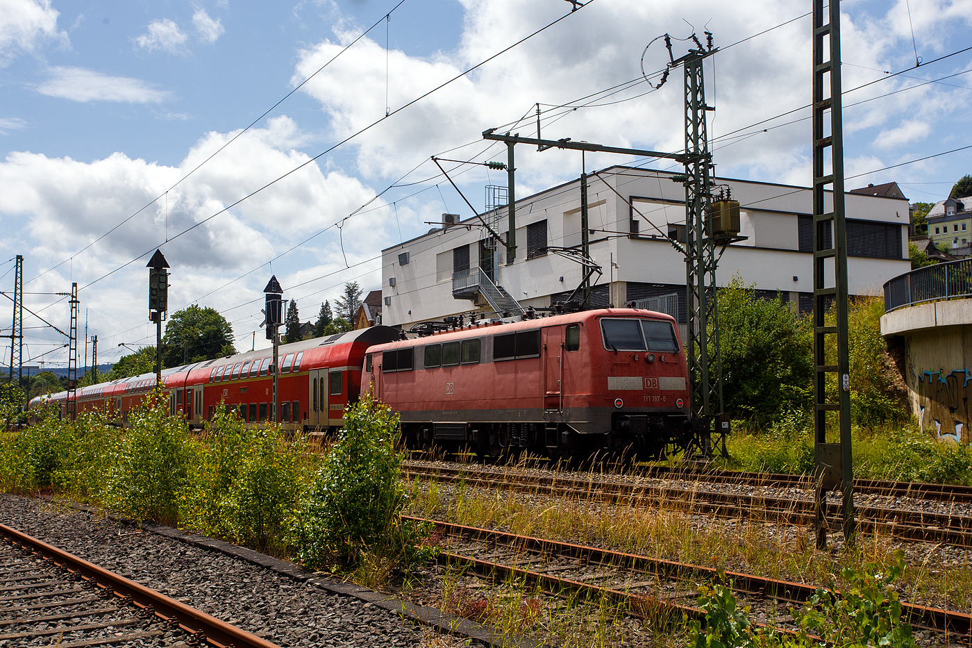Die 111 197-0 (91 80 6111 197-0 D-DB) der DB Regio NRW bzw. DB Gebrauchtzug schiebt den RE 9 rsx - Rhein-Sieg-Express (Siegen – Köln – Aachen) am 21 Juni 2024 in schneller Fahrt Steuerwagen voraus durch Niederschelden in Richtung Köln.

Die Lok wurde 1982 von Friedrich Krupp in Essen unter der Fabriknummer 5508 gebaut, der elektrische Teil wurde von AEG unter der Fabriknummer 9023 geliefert.
