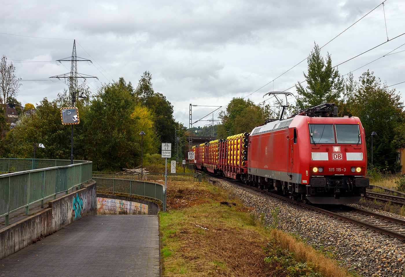 Die 185 115-3 (91 80 6185 115-3 D-DB) der DB Cargo Deutschland AG fährt am 26 September 2024 mit einem Röhrenzug auf der Siegstrecke durch Siegen-Eiserfeld in Richtung Köln. Der Zug bestand aus Drehgestellflachwagen mit Niederbindeeinrichtungen der Gattungen Snps 719 / Sns 727, beladen mit gelb beschichteten Gasrohren bzw. HFI-längsnahtgeschweißte Stahlrohre Ø 323.9 x 12,7 (DN/NW 300 mm bzw. 12 ¾ Inch) mit gelber MAPEC® Polyethylen (HDPE)-Umhüllung), der Salzgitter Mannesmann Line Pipe GmbH in Siegen (ex RW Fuchs), in Herstellungslänge von 12 m. 

Nochmals einen lieben Gruß an den netten grüßenden Lokführer zurück.

Die TRAXX F140 AC1 wurde 2003 von der Bombardier Transportation GmbH in Kassel unter der Fabriknummer 33554 gebaut. Man kann es auch an den vier Stromabnehmern erkennen, die Lok hat die Zulassung für Deutschland und die Schweiz (D/CH).
