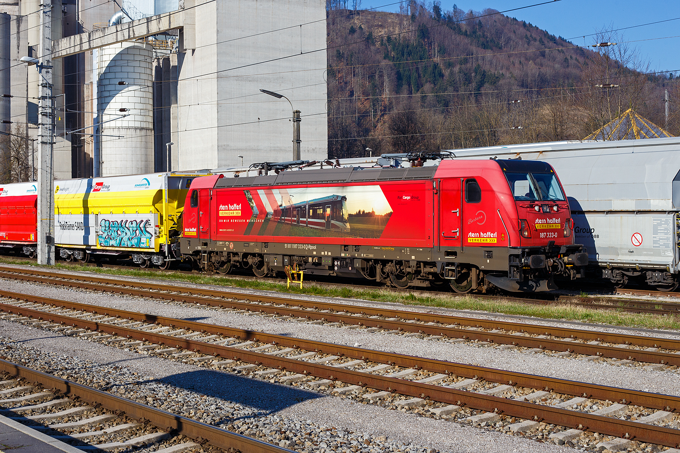 Die an die Stern & Hafferl Verkehrsgesellschaft m.b.H. (StH) vermiete 187 333-0 „Barbara“ (91 80 6187 333-0 D-Rpool, ex 91 81 1187 333-0 A-STH) der Railpool GmbH (M�nchen) kommt am 03 April 2025 im Dieselbetrieb, mit einem Kalkstein beladenen RockTainer SAND-Zug, vom Kalksteinbruch in Ebensee kommend beim Bahnhof Gmunden bzw. beim Zementwerk Hatschek der Rohrdorfer Zement GmbH in Gmunden an.

Die Bombardier TRAXX F140 AC3 LM wurde 2018 von der Bombardier Transportation GmbH in Kassel unter der Fabriknummer 35513 gebaut und an die Stern & Hafferl Verkehrsgesellschaft m.b.H. (Gmunden) geliefert. Die Lok wurde 2023 an Railpool verkauft und STH hat sie seitdem nur noch gemietet. Sie hat die Zulassungen f�r Deutschland (D) und �sterreich (A), f�r H/RO sind durchgestrichen. Fragw�rdig ist die angeschriebene UIC-Nummer …D-Rpool, da es nicht mit den Nummern �bereinstimmt.  

Der Zug bestand aus 2 x 4-achsigen Flachwagen in Sonderbauart (Doppelwagen) bzw. 8-achsig Containertragwagen, der Gattung Sggrrs 80 ft, der �sterreichischen INNOFREIGHT bzw, Rail Cargo Austria. Die achtachsigen Wageneinheiten (80ft Sggrrs IW) sind f�r den Transport von Ladegut mit Ladegestellen geeignet, hier in der Variante J - RockTainer SAND mit einer ISO-L�nge von 40‘. Mit einer maximalen Zuladung von 134,4 Tonnen pro Doppelwagen k�nnen gro�e Mengen problemlos transportiert werden. Das ist mit herk�mmlichen Containern oder auf LKWs unvorstellbar. Die Entladung erfolgt in einen Tiefbunker.

Die Rohrdorfer Unternehmensgruppe nutzt f�r die Lieferung von Kalkstein vom Steinbruch Ebensee in das Zementwerk Gmunden die neuen RockTainer SAND-Tragwagen der �sterreichischen �BB Rail Cargo Group (RCG), dem f�hrenden Bahnlogistiker in Europa. Die Spezialtransportwaggons wurden von der RCG in Zusammenarbeit mit der Rohrdorfer Unternehmensgruppe und Innofreight, ein �sterreichisches G�tertransport- und Logistikunternehmen, entwickelt, um mehr Ladung mit weniger Fahrten transportieren zu k�nnen. Seit Mai 2023 werden die 20 neuen, sogenannten InnoWaggons mit 40 RockTainer SAND-Containern auf der ca. 15 km langen Strecke Ebensee–Gmunden (Teilst�ck der „Salzkammergutbahn“ (�BB 170) Bahnstrecke Stainach-Irdning �ber Attnang-Puchheim nach Sch�rding). eingesetzt. Insgesamt werden in diesem Verkehr je Transportperiode rund 450.000 Tonnen Kalkstein bef�rdert. Das sind 36.000 Lkw-Fahrten, die jedes Jahr dank der umweltfreundlichen Schiene und des innovativen Equipments eingespart werden k�nnen.
