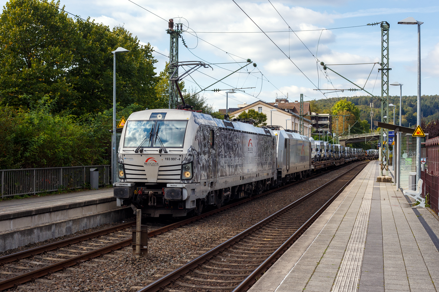 Die an die TX Logistik AG, Troisdorf  (zur Mercitalia Group geh�rend) vermietete SIEMENS Vectron AC 193 997-4 „Wir bringen die Kraft von 8.500 Pferden auf die Schiene“ (91 80 6193 997-4 D-Rpool) f�hrt am 15 September 2024, mit der kalten TXL 185 417-5 (91 81 0185 417-5 A-TXLA) der TX Logistik Austria GmbH und einem langen mit FIAT-Nutzfahrzeuge beladenen Flachwagenzug (2 x 2 achsige Flachwageneinheiten), durch den Bahnhof Kirchen (Sieg) in Richtung K�ln. 

Die Wechselstromlok (AC 15 kV 16,7 Hz und AC 25 kV 50 Hz) SIEMENS Vectron AC 193 997-4 wurde 2019 von Siemens Mobilitiy in M�nchen-Allach unter der Fabriknummer 22696. Sie ist als Vectron AC B16-2b ausgef�hrt und hat so die Zulassung f�r Deutschland, �sterreich, Ungarn und Rum�nien (D / A / H + RO). Da sie eine Leistung von 6.400 kW besitzt, was 8.700 PS entspricht, so m�sste es eigentlich hei�en „8.700 Pferde“. 

Die „kalte“ Bombardier TRAXX F140 AC2 wurde 2013 von Bombardier in Kassel unter der Fabriknummer 34993 gebaut und an die TXL - TX Logistik Austria GmbH geliefert. Sie hat die Zulassung f�r Deutschland, �sterreich, D�nemark und Schweden (D / A / DK und S).
