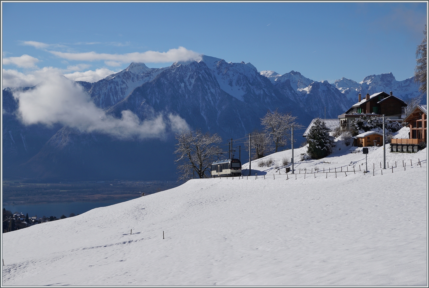 Die beiden MOB ABe 4/4 9304 und Be 4/4 9204 mit dem Regionalzug PE 2215 von Zweisimmen nach Montreux verlassen das Blickfeld bei Les Avants, zugleich gleitet der Blick auf die Savoyer Alpen und  links im Bild den Genfer See und die Rhone Ebene. 

3. Jan. 2025