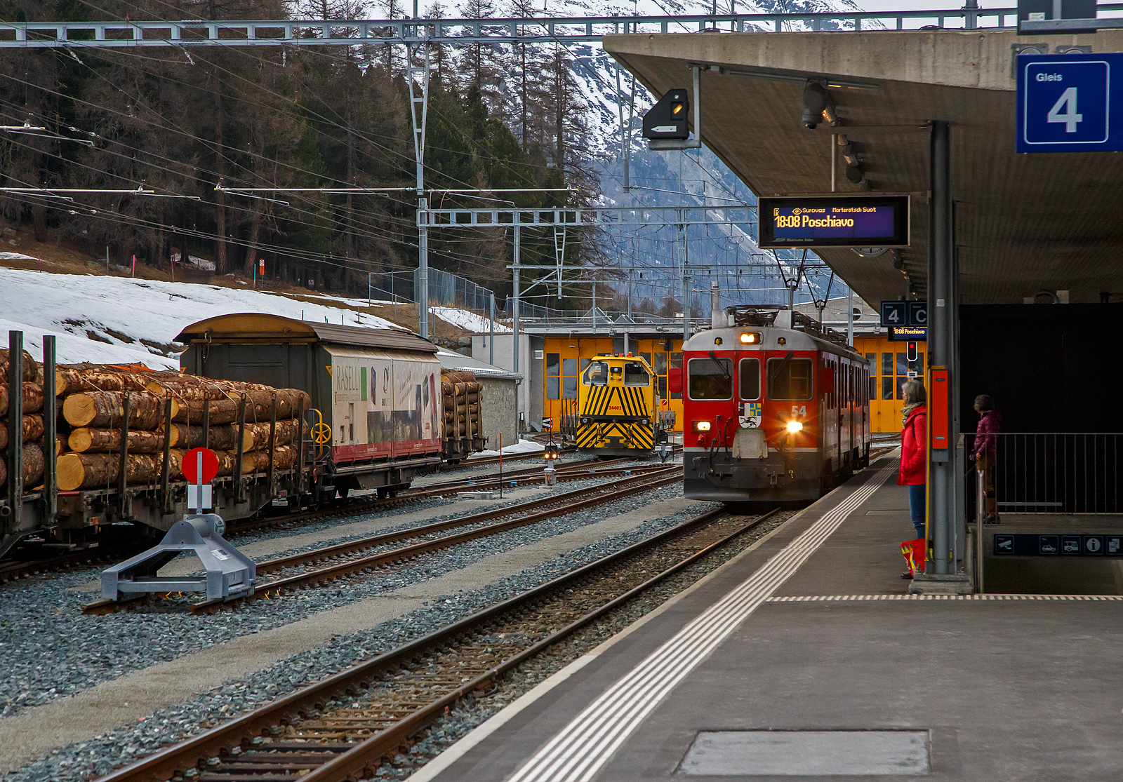 Die beiden RhB ABe 4/4 III Triebwagen 54  Hakone  und  51  Poschiavo  erreichen am 21.03.2023, als RhB-Regionalzug von St. Moritz nach Poschiavo, den Bahnhof Pontresina. Noch ist es ein reiner Personenzug, hier im Bahnhof wird er zum PmG (Personenzug mit G�terbef�rderung), denn er bekommt hier 3 mit Holz beladene vierachsige Flachwagen vom Typ “Sp-w“ angehangen. Bei der Fahrt hinauf nach Ospizio Bernina merkten wir wie die Triebwagen arbeiten mussten. 

Als ABe 4/4 III werden bei der Rh�tischen Bahn (RhB) die 1988 und 1990 beschafften Gleichstrom-Elektrotriebwagen mit den Betriebsnummern 51 bis 56 bezeichnet. Die Schlepptriebwagen werden nur auf der Berninabahn eingesetzt, wo sie die Verkehrszunahme bew�ltigen helfen. 

Die von SWA (Schindler Waggon AG in Altenrhein) und BBC (Brown, Boveri & Cie. in Baden) in zwei Serien (1988 und 1990)zu je drei St�ck gebauten und gelieferten Triebwagen waren seinerzeit die ersten RhB-Triebfahrzeuge in Umrichtertechnik mit Drehstrom-Asynchronmotoren. Zudem geh�rten sie weltweit zu den ersten Gleichstromtriebfahrzeugen mit GTO-Thyristoren. Sie sind 65 km/h schnell, 47 Tonnen schwer und waren mit einer Stundenleistung von 1.016 kW bei Ablieferung die st�rksten Gleichstromtriebwagen der RhB. Ihre Anh�ngelast bei 70 Promille Steigung betr�gt 90 beziehungsweise 95 Tonnen, sofern nur Vierachser im Zug sind. Sie weisen zw�lf Sitzpl�tze in der ersten und 16 in der zweiten Klasse auf. Dank Vielfachsteuerung k�nnen sie untereinander und auch mit den �lteren ABe 4/4 II 41–49 sowie Gem 4/4 801–802 in Doppeltraktion fahren, wovon im t�glichen Betrieb reger Gebrauch gemacht wird. Eine Doppeltraktion von zwei ABe 4/4 III hat theoretisch eine Leistungsreserve f�r die Bef�rderung von weiteren 50 Tonnen, da die maximale Zughakenlast von 140 Tonnen auf der Berninabahn nicht �berschritten werden darf.

TECHNISCHE DATEN:
Gebaute Anzahl: 6 (Nummerierung 51 – 56)
Hersteller: SWA / BBC
Baujahre: 1988 und 1990
Achsformel: Bo′Bo′
Spurweite: 1.000 mm
L�nge �ber Puffer: 16.886 mm
Radstand : 13.010 mm
Breite: 2.650 mm
Dienstgewicht: 47 t 
H�chstgeschwindigkeit: 65 km/h
Dauerleistung: 1.016  kW
Anfahrzugkraft: 178 kN
Stundenzugkraft: 108 kN bei 34 km/h
Stromsystem: 1 kV DC (Gleichstrom)
Strom�bertragung: 2 Einholmstromabnehmer
Steuerung:  GTO-Thyristor
Sitzpl�tze: 1. Klasse: 12 / 2. Klasse: 16

