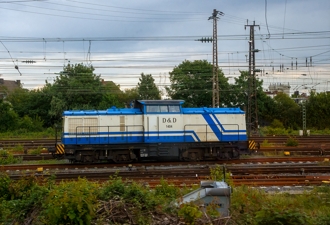 Die D&D 1404 bzw. 203 221-7 (92 80 1203 221-7 D-DUD) der D&D Eisenbahngesellschaft mbH (Hagenow), ex DB 202 735-7, ex DR 112 735-6, ex DR 110 736-8, steht am 31.05.2022 beim Bahnhof Hamm (Westf.). Aufnahme aus dem Zug heraus.

Die Diesellok eine DR V 100.1 wurde 1973 von LEW (VEB Lokomotivbau Elektrotechnische Werke „Hans Beimler“, Hennigsdorf) unter der Fabriknummer 14436 gebaut und als DR 110 735-8 an die Deutsche Reichsbahn ausgeliefert. 1986 erfolgte bereits eine Remotorisierung/Umbau im Bw Dresden und die Umzeichnung in DR 112 735-6. Zum 01.01.1992 erfolgte die Umzeichnung in DR 202 735-8 und zum 01.01.1994 dann DB AG. Die Ausmusterung bei der DB erfolgte 2001und sie ging sie die SFZ - Schienenfahrzeugzentrum (später ALS) Stendal. Von der ALS - ALSTOM Lokomotiven Service GmbH in Stendal erfolgte dann der Umbau (teilmodernisiert) in die heutige 203 221-7. Im Jahr  2006 wurde sie an die D&D Eisenbahngesellschaft mbH (Hagenow) verkauft und hat seit 2007 die UIC-Nummer 92 80 1203 221-7 D-DUD. 

TECHNISCHE DATEN:
Spurweite: 1.435 mm (Normalspur)
Achsanordnung: B'B'
Länge über Puffer: 14.240mm
Radsatzabstand im Drehgestell: 2.300mm
Drehzapfenabstand: 7.000mm
Höhe über SO: 4.255mm
Dienstgewicht: 68 t

Motor: 12-Zylinder CATERPILLAR-Dieselmotor mit Direkteinspritzung, Abgasturbolader und Ladeluftkühlung, vom Typ CAT 3512 DI-TA
Motorleistung: 1.082 kW (1.472 PS)
Nenndrehzahl: 1.800 U/min
Hubraum: 51,8 Liter (Bohrung-Ø 170 x Hub 190 mm)
Motorgewicht: 6.537 kg

Getriebe: Voith Strömungsgetriebe GSR 30/5,7
Leistungsübertragung: dieselhydraulisch
Anfahrzugkraft: 207 kN
Höchstgeschwindigkeit: 100 km/h
Kleinste Dauerfahrgeschwindigkeit: 11,1 km/h
Kleinster befahrbarer Gleisbogenradius: 80m