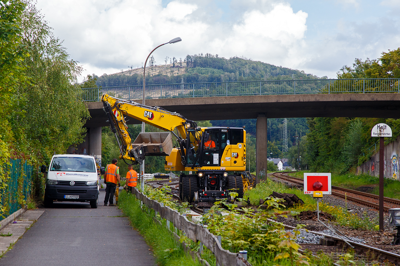 Die KSW (Kreisbahn Siegen-Wittgenstein) erneuert die ersten Gleismeter vom Anschlussgleis, zum Rangierbahnhof in Herdorf der Betriebsstätte FGE -Freien Grunder Eisenbahn (KSW NE447 / DB-Nr. 9275).

Hier am 16.08.2023 im Einsatz der Caterpillar CAT M323F Zweiwegebagger mit hydrostatischem Schienenradantrieb (Serien-Nr. RH600 189), Kleinwagen Nr. D-ZBM 99 80 9902 521-0 der ZEPPELIN Baumaschinen GmbH (Garching), ein Mietbagger vermietet an die Firma  W. Hundhausen Bauunternehmung GmbH (Siegen). Es werden die ersten Gleismeter vom Anschlussgleis erneuert, der Bagger ist bei der Einschotterung.
