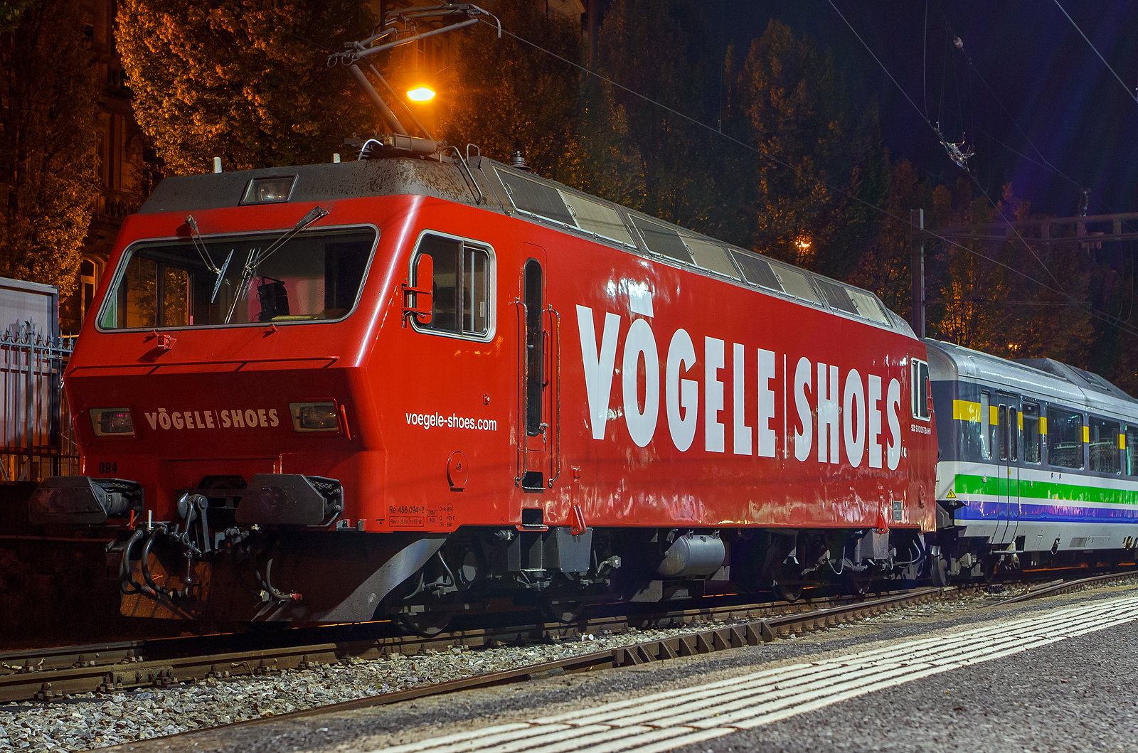 Die SOB (S�dostbahn) Re 456 094-2  Herisau    (91 85 4456 094-2 CH- SOB) im V�gele Shoes Design ist am 29.09.2012 (3:30 Uhr) mit dem Voralpen Express in Luzern abgestellt.

Diese vierachsige normalspurige Lokomotive in Umrichtertechnik wurde 1987/88 von der SLM - Schweizerische Lokomotiv- und Maschinenfabrik in Winterthur unter der Fabriknummer 5306 gebaut, der elektrische Teil ist von der BBC Baden. Die Bo'Bo'-Lok (Re 4/4) wurde an die die Bodensee-Toggenburg-Bahn (BT) geliefert, die BT fusionierte 2001 mit der SOB (S�dostbahn). Im Januar 2021 wurde sie an den Verein Depot und Schienenfahrzeuge Koblenz (DSF) verkauft.

Die SLM Re 456 ist eine vierachsige Lokomotive in Umrichtertechnik, die in den sp�ten Achtzigerjahren von SLM und BBC (sp�ter ABB) entwickelt und f�r Schweizer Privatbahnen konstruiert wurde. Die Lok wird daher gelegentlich als KTU-Lok bezeichnet, kurz f�r „Konzessionierte Transport-Unternehmungen“ (KTU), welcher Begriff damals die Privatbahnen einschloss, nicht aber die SBB.

Entstehung
Anfang der 1980er-Jahre hat das Bundesamt f�r Verkehr (BAV) bei mehreren Schweizer Bahnunternehmungen das Bed�rfnis f�r eine Streckenlokomotive mittlerer Leistungsklasse abkl�ren lassen. Zu diesem Zeitpunkt hatte nur die Bodensee-Toggenburg-Bahn (BT) ein Bed�rfnis an einer Lokomotive mit einer Leistung von 3 MW und einer H�chstgeschwindigkeit von 130 km/h, um unter anderem die BT Be 4/4 von 1931 abzul�sen. Aufgrund der Erfahrungen mit der Umrichtertechnik, die bei der SBB Ee 6/6 II, der DB E 120 und der NSB El 17 gemacht wurden, gab das BAV die Zustimmung f�r die Finanzierung (mit Schwerpunkt Entwicklung) eines Lokomotivtyps mit Umrichtern in GTO-Technik. Das BAV kn�pfte an die Finanzierung die Bedingung, dass der Lokomotivtyp auch f�r andere Privatbahnen geeignet sein m�sse, was sich schlie�lich in der Zusammenarbeit zwischen der Schweizer Industrie, den Schweizerischen Bundesbahnen (SBB) und diversen Privatbahnen niederschlug.

Entwicklung
Die Entwicklung begann mit der Bestellung von 6 Maschinen durch die BT, an die sich die Sihltal-Z�rich-Uetliberg-Bahn (SZU) bald darauf mit einem Bedarf von 2 Maschinen anschloss. Der Auftrag f�r die Produktion dieser ersten Serie �ber 8 Lokomotiven wurde an die Schweizerische Lokomotiv- und Maschinenfabrik (SLM) und Brown, Boveri & Cie (BBC) vergeben. Im Verlauf des Jahres 1987 wurden die Maschinen an ihre jeweiligen Besteller ausgeliefert, wo sie unter der Typenbezeichnung Re 4/4 in Betrieb genommen wurden.

Nachbestellung
Die SZU hatte durch die Fahrgastzunahme infolge der Inbetriebnahme der S-Bahn Z�rich im Jahr 1990 einen Mehrbedarf an Triebfahrzeugen, worauf es zu einer Nachbestellung von 4 Maschinen kam, an welche sich die Vereinigten Huttwil-Bahnen (VHB) mit 2 Maschinen anschlossen. Die Nachbestellung wurde 1993 ausgeliefert. Aufgrund eines hohen Auftragsbestands bei der SLM wurde der Bau der Lokomotivk�sten aus Kapazit�tsgr�nden an die SGP Verkehrstechnik in Graz untervergeben. Die Maschinen wurden in Graz einschlie�lich der elektrischen Ausr�stung von ABB fertig montiert und anschlie�end (bis Mai 1993) auf Hilfsdrehgestellen zur SLM �berstellt, wo die Endmontage und der Einbau der Drehgestelle erfolgte.

Weiterentwicklung
Da sich die Lokomotiven im t�glichen Einsatz bew�hrten und die SBB, f�r die im Aufbau befindliche S-Bahn Z�rich, Bedarf an Lokomotiven dieser Leistungsklasse hatten, wurde basierend auf diesem Lokomotivtyp die Re 4/4 V (Re 450) entwickelt. Dieser Lokomotivtyp unterscheidet sich von der Re 456 vor allem �u�erlich durch seinen asymmetrischen Lokomotivkasten mit einseitigem F�hrerstand.

Pflichtenheft
Die Lokomotive wurde von Anfang an als Universallokomotive ausgelegt, unter anderem um die BT Be 4/4 von 1931 abzul�sen. Als Haupteinsatzgebiet wurden die Schnellz�ge Romanshorn – St. Gallen – Wattwil – Rapperswil – Arth Goldau – Luzern bestimmt, die heute als Voralpen-Express vermarktet werden. Daneben sollten auch verpendelte Regionalz�ge Romanshorn – Rapperswil und Wil – Nesslau, sowie G�terz�ge bis 670 Tonnen (Romanshorn – Herisau) respektive bis 1500 Tonnen (St. Gallen – St. Gallen Haggen) gef�hrt werden k�nnen. Das daraus entstandene Leistungsdiagramm deckte auch die Bed�rfnisse der SZU ab.

Das definierte Einsatzgebiet beinhaltet Strecken mit einer Steigung von bis zu 50‰, die Leistung reicht um die H�lfte der maximal zul�ssigen Zughakenlast auf den Steigungen zu bef�rdern, so dass in Doppeltraktion die maximal zul�ssige Zughakenlast bef�rdert werden kann.

Die Zugkraft sollte in den unteren Geschwindigkeitsbereichen konstant bei 240 kN liegen, die Gesamtleistung von 3 MW sollte im gesamten Geschwindigkeitsbereich bis 130 km/h zur Verf�gung stehen. Die elektrische Rekuperationsbremse war auf Grund des maximalen Pufferdrucks auf 140 kN zu begrenzen.

TECHNISCHE DATEN:
Spurweite: 1.435 mm (Normalspur)
Achsfolge: Bo' Bo'
L�nge �ber Puffer: 16.600 mm
Drehzapfenabstand: 9.000 mm
Achsabstand im Drehgestell: 2.700 mm
Treibraddurchmesser: 1.100 mm (neu)
Dauerleistung: 3.200 kW
H�chstgeschwindigkeit: 130 km/h
Gewicht: 68.0 t
Anfahrzugkraft: 240 kN
Kleinster befahrb. Gleisbogen: R 150 m
Fahrleitungsspannung: 15000 V, 16.7 Hz ~

