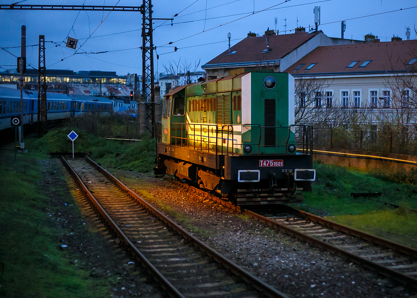 Die T 475.1501, alias 744 501-8 (CZ- RLK 92 54 2 744 501-8) der Retrolok s.r.o. (Prag) ist am 22.11.2022 beim Bahnhof Praha-Smíchov (tschechisch: Stanice Praha-Smíchov) abgestellt (aufgenommen aus einem alex-Zug). Der  Schmetterling  ist eine dieselelektrische Lokomotive, und wurde 1970 von ČKD in Prag (Českomoravská-Kolben-Daněk) als Prototyp gebaut. 

Die Lokomotive der Baureihe 744.5 (bis 1987 die Baureihen T 475.15 und T 476.0) ist eine vierachsige dieselelektrische Lokomotive, die 1970 in zwei Prototypen von der Lokomotivfabrik ČKD in Prag hergestellt wurde. Sie ist ein Entwicklungsvorläufer der späteren Serienlokomotiven der Baureihen 740 und 742 (bzw. 743). Zwei Jahre später entstand ein dritter Prototyp jedoch mit einem Achtzylindermotor K 8 S 230 DR.

Im Rahmen der Modernisierung des ČKD-Produktionsprogramms Ende der 1960er Jahre wurde die Entwicklung eines völlig neuen Typs von Reihensechszylindern mit einer Bohrung von 230 mm, im Zweigwerk Smíchov der ČKD Naftové motory (sog. Werk Wilhelm Pieck), begonnen. Dieser wurde als K 6 S 230 DR bezeichnet. Der geplante Einsatz dieses Motors sollte sowohl in Gleis- als auch in Rangierlokomotiven erfolgen. Um den neuen Motor in der Praxis testen zu können und gegebenenfalls konstruktive Mängel auszubessern, wurden 1970 zwei Prototypen gefertigt, die als Baureihe T 475.15 (heute 744.5) bezeichnet wurden. Bei jedem von ihnen wurde der Motor zum Testen auf eine andere Leistung (zwischen 600 bis 883 kW) eingestellt. Gleichzeitig wurde dieser Typ erstmals verwendet, um den Rahmen mit Gummi-Metall-Verbindungen am Fahrgestell zu befestigen, was später zum Standard wurde. Beide Prototypen wurden zunächst im ŽZO in Cerhenice getestet und dann an die ČSD zur Erprobung in den Schnellzügen von Prag nach Babín vermietet. Neben diesen beiden Prototypen mit dem Motor K 6 S 230 DR wurde 1972 ein dritter produziert, der als Baureihe T 476.0 bezeichnet und mit einem stärkeren Achtzylinder K 8 S 230 DR ähnlichen Konzepts ausgestattet und verglichen wurde zu schwächeren Maschinen.

Die Erprobung war 1973 abgeschlossen, und da die Produktionsvorbereitung der neuen Baureihe T 448.0 (740) bereits im Endstadium war, wurden beide Sechszylinder-Maschinen zum Verkauf angeboten. Das erste davon wurde von AZNP in Mladá Boleslav (heute Škoda Auto) gekauft und war hier bis 2017 in Betrieb, bevor sie von RETROLOK s.r.o. (Prag) ersteigert wurde. Am zweiten zeigte das Zementwerk in Hranice in Mähren Interesse. Später ging es in den Besitz des Dienstleistungsunternehmens Lokotrans über und wird heute von BF Logistics betrieben. Die Achtzylindermaschine hatte nicht so viel Glück - zwischen 1974 und 1978 wurde sie abwechselnd an die ČSD vermietet und in eigener Regie getestet, in den achtziger Jahren wurde sie in den Hütten in Kladno eingesetzt und 1988 wurde sie aufgrund ihrer endgültig eingestellt und verschrottet. 

TECHNISCHE DATEN der T 475.1501:
ČKD-Bezeichnung: 1435 Bo´Bo´ 1200
Spurweite: 1.435 mm
Achsfolge: Bo'Bo'
Länge über Puffer 13 540 mm
Dieselmotor: 6-Zylinder-Viertakt-Reihen- Dieselmotor mit Direkt-Einspritzung und Turbolader vom Typ ČKD  K 6 S 230 DR
Motorhubraum: 64,75 Liter (Zylinder-Ø 230 mm / Kolbenhub 260 mm)
Kompressionsverhältnis: 12,5 : 1
Nenndrehzahl: 400 – 1.250 U/min
Motorgewicht (ohne Generator): 7.700 kg
Leistung: 846 kW (1.150 PS)
Leistungsübertragung: dieselelektrisch
Höchstgeschwindigkeit: 140 km/h
Dienstgewicht: 60 t
Kleinster bef. Halbmesser: R 80 m
Anfahrzugkraft: 180 kN

Quellen: RETROLOK s.r.o., Wikipedia (CZ), zos-vrutky.sk