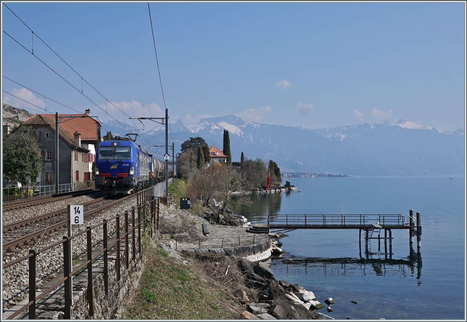 Die WRS Re 475 902 fährt mit einem Kesselwagenzug Richtung Lausanne bei St-Saphorin am Genfer See entlang. Das Bild entstand auf dem Bahnsteig von St-Saphorin.

25. März 2022 