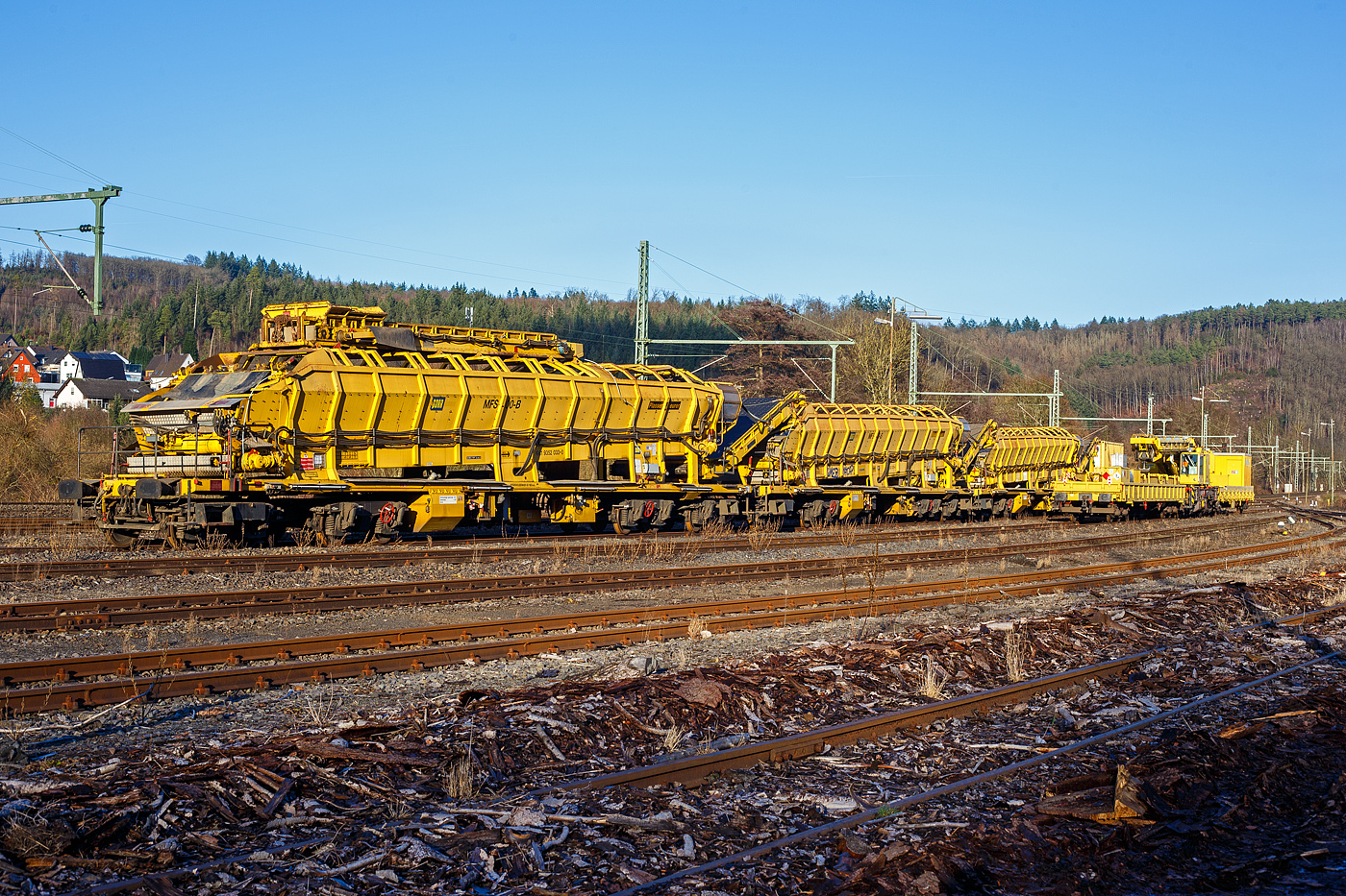 Drei Plasser & Theurer Materialf�rder- und Siloeinheiten (MFS 100) der �sterreichischen Gleisbaufirme PORR AG (Wien) sind, mit einem Schutzwagen, am 26 Dezember 2024, in Scheuerfeld/Sieg abgestellt. Davor auf dem Gleis steht der GOTTWALD Gleisbauschienenkran GS 80.08 T, Schweres Nebenfahrzeug Nr. 99 80 9419 007-6 D-Krebs der Krebs Gleisbau GmbH & Co. KG, Bingen am Rhein (Tochterunternehmen der schweizerischen KREBS Gleisbau AG, Bern), in Transportstellung mit dem Gegenlastwagen 37 80 3940 046-0 D-KREBS der Gattung Res und dem Schutzwagen auslegerseitig 99 80 9383 002-9 D-Krebs..

Hier im Vordergrund (links) die P&T Materialf�rder- und Siloeinheit MFS 100 B mit integrierter Beladestation (in Transportstellungen oben auf dem MSF) 99 81 9352 033-0 A-PTU.

TECHNISCHE DATEN:
Hersteller: Plasser & Theurer, Linz an der Donau (�sterreich)
Spurweite: 1.435 mm
L�nge �ber Puffer: 22.900 mm
Achsanzahl: 8 (in 2 Doppel-Drehgestellen)
Drehzapfenabstand der Doppeldrehgestelle: 15.100 mm
Drehzapfenabstand der Einzeldrehgestelle: 3.900 mm Achsabstand der Einzeldrehgestelle: 1.500 mm
Motorleistung: 165 kW (wassergek�hlter Deutz BF6M 1013 C Motor f�r Bandantrieb)
Eigengewicht: 67 t
Nutzlast: 77 t ab D4
Fahrgeschwindigkeit in Schleppfahrt leer, max.: 120 km/h
Fahrgeschwindigkeit in Schleppfahrt beladen, max.:100 km/h
Fassungsverm�gen: 68 m�
F�rderleistung (materialabh�ngig), max.: 700 – 800 m�/h
Entladezeit: ca. 5 min
Besonderheit: mit integrierter Beladestation
