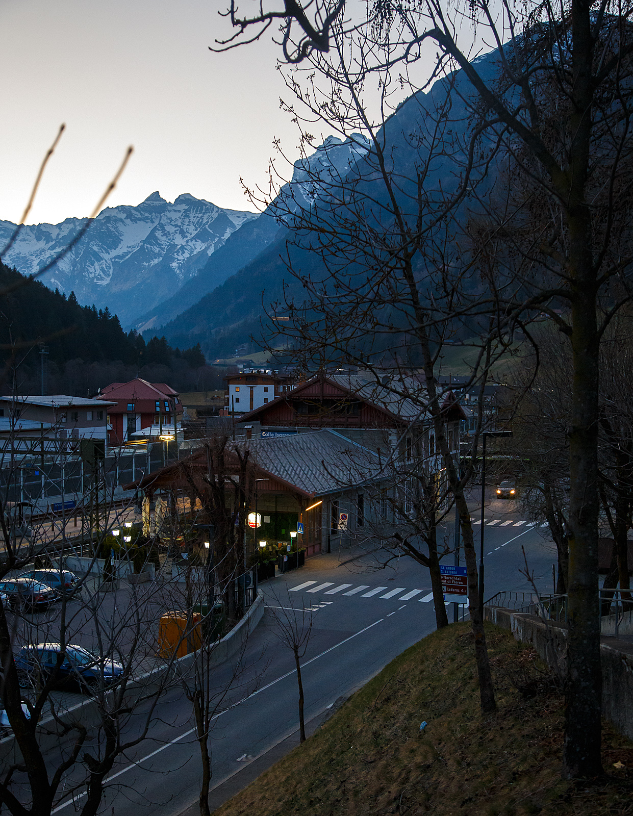Ein abendlicher Blick auf den Bahnhof Gossensaß/Colle Isarco am 26.03.2022.
Der Bahnhof Gossensaß (auch Gossensass; italienisch Stazione di Colle Isarco) befindet sich an der Brennerbahn in Südtirol (italienisch Alto Adige), amtlich Autonome Provinz Bozen – Südtirol.

Der Bahnhof Gossensaß ist der erste Haltepunkt im Wipptal südlich des Brennerpasses, zu dem die Bahnstrecke von hier aus über den Pflerschtunnel ansteigt. Er liegt auf 1.066,9 m Höhe nahe dem Zentrum von Gossensaß, dem Hauptort der Gemeinde Brenner, und der durch das Dorf führenden SS 12 (der alten Brennerpass-Straße). 

Der Bahnhof wurde 1867 zusammen mit dem gesamten Abschnitt der Brennerbahn zwischen Innsbruck und Bozen in Betrieb genommen. Durch ihn erlebte Gossensaß bis zum Ersten Weltkrieg seine Blütezeit als bekannter Touristenort. Er konkurrierte mit Orten wie St. Moritz oder Chamonix. 

Das Aufnahmegebäude war zunächst noch relativ kompakt gehalten, wurde wegen der vielen Touristen jedoch noch im 19. Jahrhundert durch einen südlichen Anbau erweitert. Das ursprüngliche Gebäude weist eine Verkleidung aus Grauwacke auf, während dekorative Details wie die Fensterfassungen in weißem Kalkstein gehalten sind. Straßenseitig ist es durch einen in sorgfältigen Details gearbeiteten Dachgiebel aus Holz gestaltet. Der Anbau ist in Brixner Granit gemauert und sticht durch eine hölzerne Veranda hervor. In dem sich heute das Buffet befindet und man auch den Espresso genießen kann. Das Gebäude steht seit dem Jahr 2000 unter Denkmalschutz.

Der Bahnhof Gossensaß wird durch Regionalzüge der Trenitalia sowie der SAD bedient, die auch Busverbindungen zum Bahnhof betreibt. Die Regionalzüge fahren in beide Richtung (Brenner bzw. Bozen) im Stundentakt und werden zu Hauptverkehrszeiten durch Regionalexpresszüge verdichtet.

Uns hat es in Gossensaß sehr gut gefallen, es war einfach zu kurz, so dass wir gerne wiedermal dort hinfahren wollen. Für die drei Tage haben wir uns ein Südtirol/Alto Adige Ticket (eine Mobilcard für 3 Tage) am Automat für 23,00 Euro geholt. So konnten wir mit diesem Ticket Südtirol mit der Bahn erkunden. 