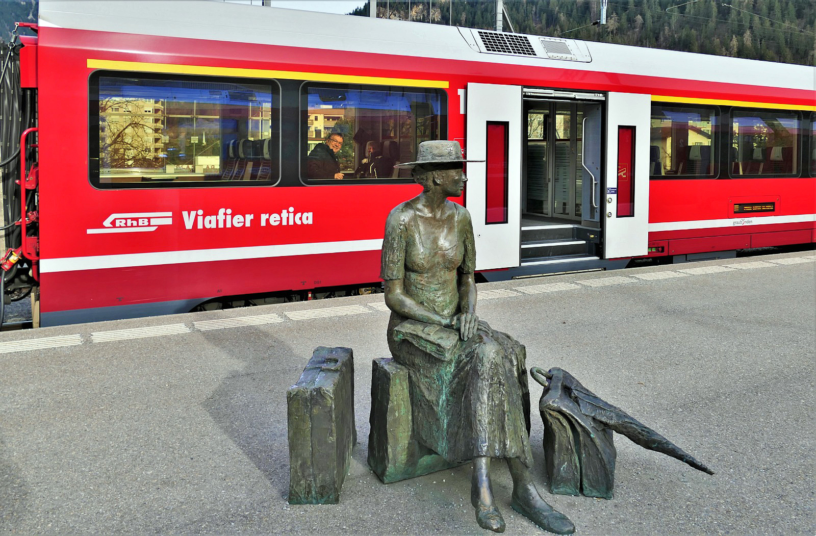 Hier aus der Sicht von Herbert (Foto Herbert Graf), die „wartende Reisende von Thusis“ vom Bildhauer Robert Indermaur und dahinter zwei auf die Abfahrt wartende Reisende in einem Alvra-Gliederzug, am 21.03.2023 im Bahnhof Thusis, wo die Albulabahn beginnt.