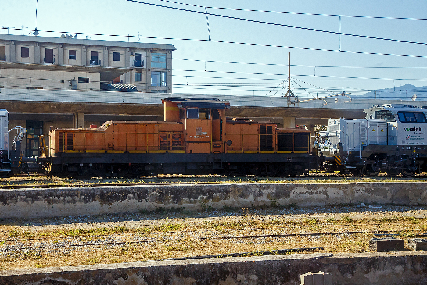 Im Juli 2022 erledigten den Verschub fürs Trajekt-Manöver an den Ufern der Straße von Messina, noch die älteren RFI D.145 Loks der Serie 2000, aber die modernen Vossloh DE 18 der MIST - Mercitalia Shunting & Terminal S.r.l. standen schon in den Startlöchern.

Die D.145.2021 (98 83 21-45 221-7 I-RFI) der RFI (Rete Ferroviaria Italiana), am 20.07.2022 abgestellt beim Bahnhof Messina Centrale. Aufnahme aus einem IC Notte.

