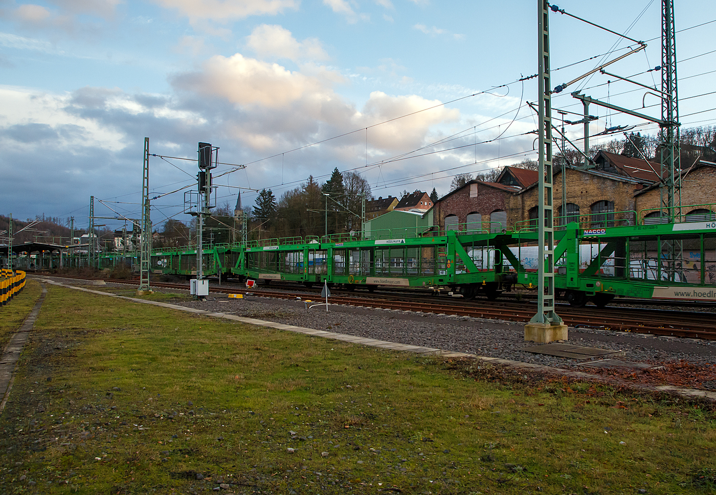 Leerer offener vierachsiger Doppelstock- Autotransportwaggon 27 80 4371 608-5 D-NACCO, der Gattung Laaers 560.1 (BA 5.854), noch registriert unter NACCO AG (geh�ren nun der TWA- TRANSWAGGON) am 11.01.2022 im Zugverband bei einer Zugdurchfahrt in Betzdorf (Sieg).

Diese Waggons haben zwei Ladeebenen und sind f�r den europaweiten Transport geeignet. Sie werden f�r den internationalen Transport von PKWs, Gel�ndewagen, und Vans eingesetzt und bieten maximale Flexibilit�t durch eine stufenlos verstellbare obere Ladeebene. Aufgrund der hohen Lastgrenze (34t) ist der Transport von besonders schweren Fahrzeugen der genannten Typen m�glich. Damit sowohl ein typenreiner Transport als auch eine Mischverladung in den unterschiedlichen Ladema�en m�glich ist, kann die obere Ladeebene hinsichtlich der Transportstellungen stufenlos eingestellt werden.

Die oberen Ladeebenen sind �ber jeweils vier dreig�ngige Spindeln und Trags�ulen mit dem Untergestell verbunden. Die S�ulenpaare lassen sich getrennt bedienen, damit die oberen Ladeebenen an den Fahrzeugenden - notwendig zur Be- und Entladung - rampenartig gestellt werden k�nnen. 

TECHNISCHE DATEN:
Gattung: Laaers 560.1 (BA 5.854),
Hersteller: ELH Waggonbau Niesky GmbH, Baujahr 2017
Spurweite: 1.435 mm
Anzahl der Achsen: 4
L�nge �ber Puffer : 31.000 mm
Achsabst�nde: 10.000 mm / 5.160 mm / 10.000 mm
Laufraddurchmesser (neu): 840 mm (au�en) / 730 mm (mittleren)
Ladel�nge : 30.070 mm (unten) / 30.550 mm (oben)
H�chstgeschwindigkeit: 100 km/h (120 km/h leer)
Eigengewicht: 30.000 kg
Nutzlast: 32 t bei Streckenklasse  A, 34,0 t ab B (max. 18 t pro Ebene)
Kleinster befahrb. Gleisbogenhalbmesser: 75 m
Bremse: KE-GP-A
Verwendungsf�higkeit: TEN-GE